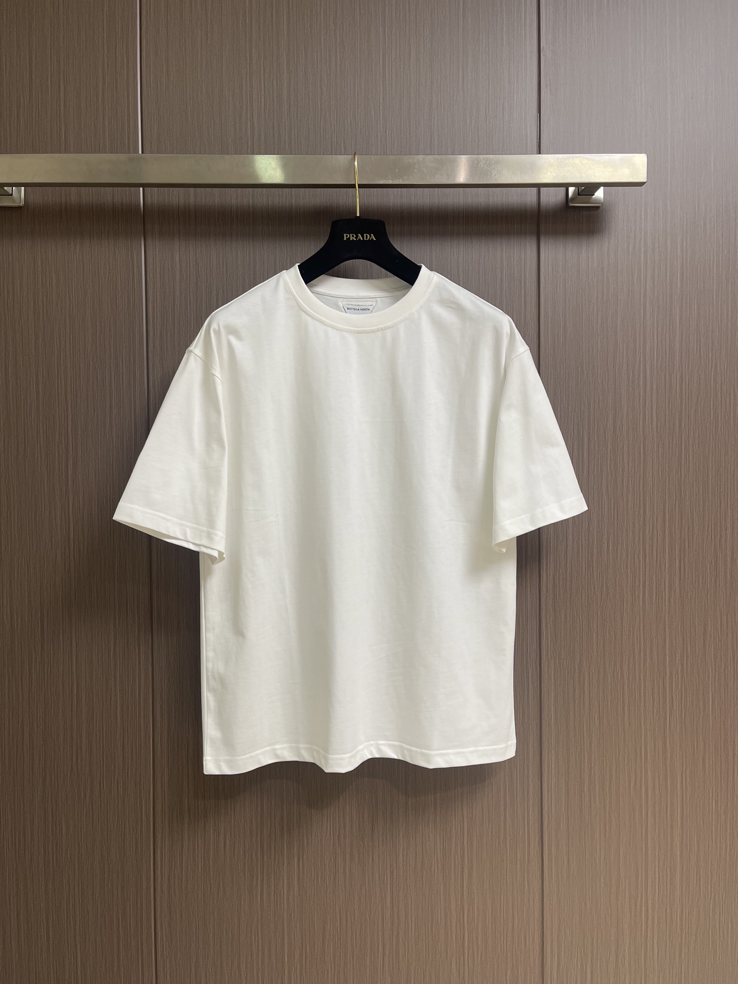 NO:842737,BV Woven triangular round neck short-sleeved T-shirt, pure cotton plain fabric. The fabric is made of 15-count special-spun compact cotton, 230gm, with 32-count 1×1 rib, 340gm. The 15-count special-spun compact cotton is a medium-low yarn count, and the yarn is thicker. The special-spun compact spinning process significantly reduces yarn hairiness, so that thick-count yarns can also present a delicate and slightly matte cloth texture. At the same time, it is large The anti-pilling level is greatly improved. The medium and high weight gives the fabric an excellent bone texture, and the cloth woven from roving has a more obvious yarn texture and micro-graininess. The 32-count high-density rib locking collar is stable, high-strength binding, and can firmly lock the neck arc. Sheep wool woven triangle patch patch, wool fiber has natural curl elasticity and matte luster. Woven into a triangle shape Finally, the chapter shows a fluffy, soft touch and rich texture levels that are different from cotton fabrics. The natural tone of wool contrasts with the pure cotton T-shirt. The crisp and dryness of cotton and the softness and warmth of wool create a visual and tactile collision. Fine cotton threads of the same color are used for high-density sewing and fixation along the edges of the chapter, which not only ensures firmness, but also makes the stitching itself a decorative element. .It adopts a conventional round neck and loose version, with precise tailoring and smooth lines. The shoulder line is processed naturally, which can highlight the wearer's shoulder line without restricting the freedom of movement, so that the clothing remains comfortable when worn. The neckline is uniquely designed and combined with the strong binding of high-density ribs. The sleeves are wide and short-sleeved. The cuffs and hem are finely closed and the structure is simple. Size XS-L XS size, bust 110, shoulder width 54.5, length 69, size S, chest size 114, shoulder width 56, length 71, size M, chest size 118, shoulder width 57.5, length 73, size L, chest size 122, shoulder width 59, length 75,,bottega veneta,T-shirt,tees,t-shirt,19860909BV 编织三角圆领短袖t恤,纯棉质平纹面料,面料采用15支特纺紧密棉,230gm,搭配32支1×1罗纹,340gm.15支特纺紧密棉属于中低纱支,纱线较粗.特纺紧密纺工艺显著减少了纱线毛羽,使粗支纱线也能呈现出细腻且微雾面的布面质感,同时大幅提升抗起毛球等级.中高克重赋予了面料极佳的骨感,粗纱织出的布面具有更明显的纱线肌理和微颗粒感.32支高密度罗纹锁定领口稳定,高强度收束,能牢牢锁定颈部弧线,绵羊毛编织三角贴饰章仔,羊毛纤维具有天然的卷曲弹性、哑光光泽.编织成三角形状后,章仔呈现出不同于棉织物的蓬松柔软触感和丰富的纹理层次.羊毛的天然色调与纯棉T恤形成材质对比,棉的挺括干爽与羊毛的柔软温暖,视觉和触觉上都有碰撞感.用同色系的细棉线沿章仔边缘进行高密度缝制固定,既确保牢固度,又让缝线本身成为装饰元素.采用常规圆领宽松版型,剪裁精准、线条流畅.肩线处理自然,既能够凸显穿着者的肩部线条,又不会限制活动自由度,使衣物在穿着时保持舒适.领口设计独特,配合高密度罗纹的强力收束,袖型为宽大短袖,袖口与下摆均采用精细收口,结构简洁.尺码XS-L XS码胸围110肩宽54.5 衣长69 S码 胸围114肩宽56 衣长71 M码胸围118 肩宽57.5 衣长73 L码 胸围122 肩宽59 衣长75,,bottega veneta,T-shirt,tees，t-shirt,,Men's clothing