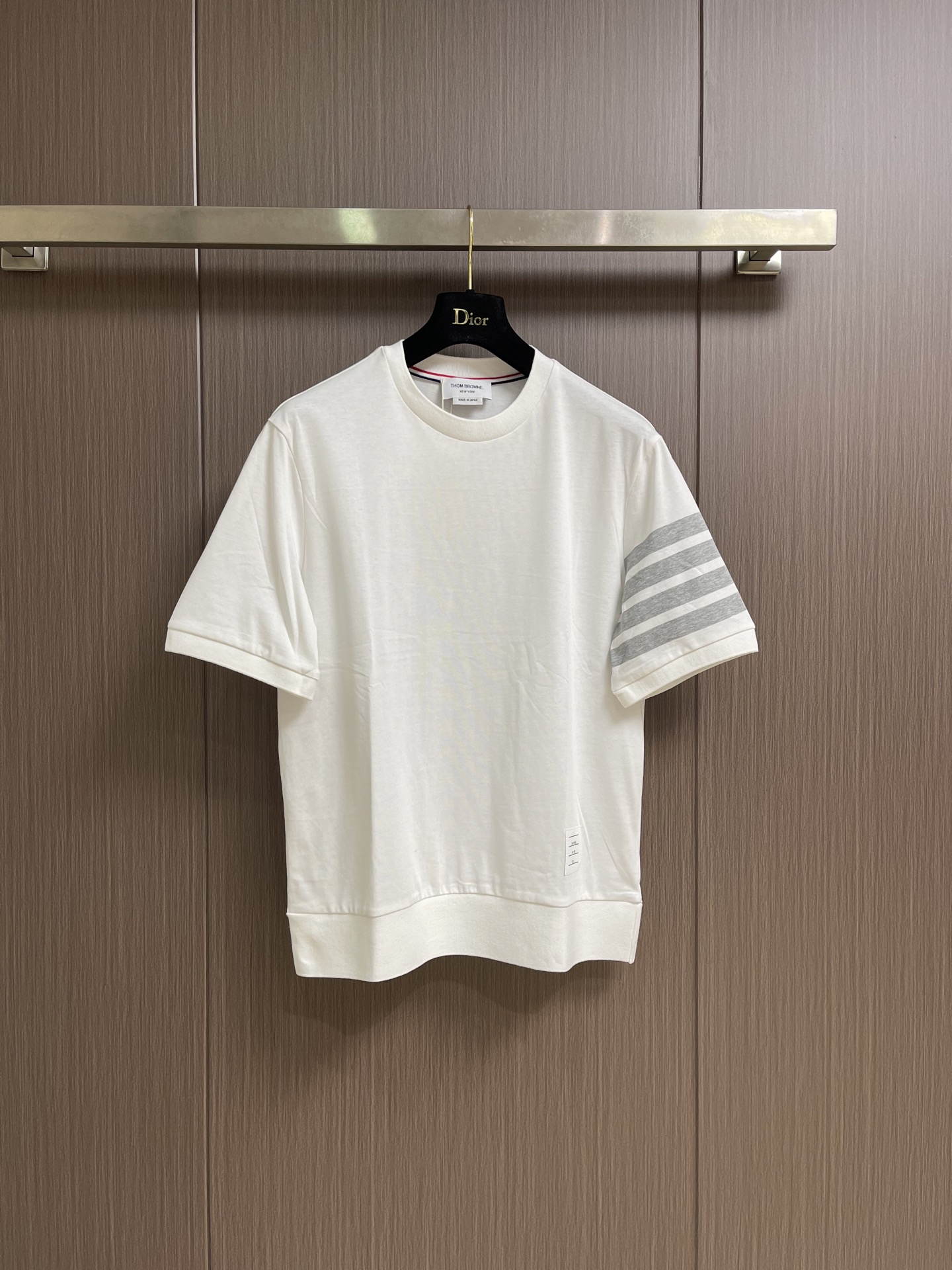 NO:845221,THOM BROWNE  Short-sleeved T-shirt with four stripes on the sleeves and arms. This T-shirt is made of 230g high-weight combed cotton knitted fabric. The surface of the fabric presents a delicate and full honeycomb texture. It feels soft and skin-friendly and has excellent breathability. It will not loosen and deform easily after being worn for a long time. The body is thin  The stitching is extremely elegant. The classic four-stripe logo on the left arm is made of high-end jacquard technology. The contrasting lines are sharp and clear, and the transition is natural and without overflowing colors. The neckline is made of warm and lustrous mother-of-pearl shell buttons, and the inner lining of the neckline is supplemented by red, white and blue three-color webbing for reinforcement.  , it is both iconic and effectively prevents neckline deformation. The placket and shoulder seams are made of double-needle hemming technology, and the stitches are fine, even and neat without losing threads; the hem adopts a classic arc design with short front and long back, and the slits on both sides are decorated with two metal buttons on each side.  It is equipped with the iconic red, white and blue webbing backing, and the brand's exclusive small logo is sewn on the inside of the hem. Every craftsmanship detail demonstrates the exquisite craftsmanship and high-end texture of high-quality garments. The overall routing is straight and delicate, the fabric is comfortable and soft, and the color is consistent with no color difference.  It can be matched with the same style to create a fashionable look, and can be used in various occasions. Customized accessories, complete with three standards, same style for men and women!  Size 1-2-3-4 1 size bust 104 shoulder width 45 length 69 size 2 bust 108 shoulder width 46 length 70 3 size bust 112 shoulder width 47 length 71 4 size bust 116 shoulder width 48 length 72,, T-shirt, tees, t-shirt,19860909THOM BROWNE 袖臂四条杠短袖T恤,这款T恤甄选230g高克重精梳棉针织面料,面料表面呈现细腻饱满的蜂巢肌理,触感软糯亲肤且具备优异的透气性,久穿不易松垮变形.衣身细节极尽考究,左臂经典的四道杠标识采用高端提花工艺,撞色线条利落分明,过渡自然无溢色；领口甄选温润光泽的珍珠母贝壳扣,领口内里辅以红白蓝三色织带包边加固,既具标志性又有效防止领口变形,门襟与肩缝处均采用双针锁边工艺,线迹细密均匀工整不脱线；下摆采用前短后长的经典弧形设计,两侧开衩处各缀两粒金属纽扣,搭配标志性红白蓝织带衬底,下摆内侧缝制品牌专属小标,每一处工艺细节都彰显出高品质成衣的精湛匠心与高级质感.整体走线平直细腻,面料舒适柔软,颜色一致无色差 能与同款搭配营造时尚造型,驾驭各种场合,定制辅料,三标齐全,男女同款！尺码1-2-3-4 1码 胸围104肩宽45 衣长69 2码 胸围108肩宽46 衣长70 3码 胸围112 肩宽47 衣长71 4码 胸围116 肩宽48 衣长72,,T-shirt,tees，t-shirt,,Men's clothing