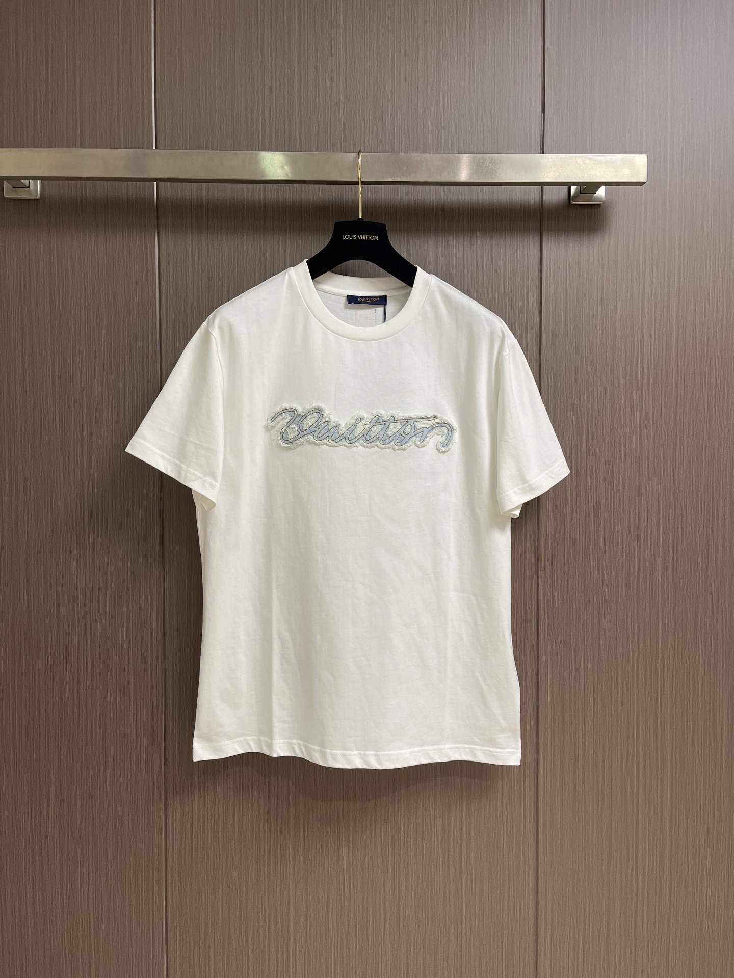 NO:847396,LV Denim appliqué embroidered round neck short-sleeved T-shirt, made of 15-count special-spun compact cotton with a weight of 230g㎡; paired with 32-count 1×1 rib; a weight of 340g㎡. The fabric is a medium-thick knitted fabric, the 15-count yarn is thicker, the fabric has a strong texture and a crisp texture. The cotton fiber cross-section of the fabric is round, Significantly enhances the gloss and smoothness. Mercerizing can improve the adsorption uniformity of dyes and make the fabric background color fuller and more uniform. It is then stretched and set by a high-temperature setting machine, and the warp and weft yarns are restored to straightness through tension control, eliminating wrinkles and internal stress. The 32-count rib neckline retracts to its optimal elastic state, and the ribbing The tight structure is fully stabilized during this process, forming a snug fit without being stretched. The patch itself is a piece of denim fabric. The pattern is precisely laser cut according to the outline of the handwriting to form a letter-shaped patch. It undergoes independent washing and distressing before sewing. Pumice and low-concentration bleach are added. Through mechanical friction and chemical action, the surface of the denim will produce irregular color fading, whitening and slight yarn breakage. This treatment simulates the natural fading and wear effects of denim after years of wearing, giving the patch a texture. The overall wiring is straight and delicate, the fabric is comfortable and soft, and the color is consistent without color difference. It can be matched with the same style to create a fashionable look, and can be used in various occasions. Customized accessories, complete with three standards, same style for men and women! Sizes XS-L19860909LV 牛仔贴布绣圆领短袖T恤,采用15支特纺紧密棉,克重为230g㎡；搭配32支1×1罗纹；克重为340g㎡.面料属于中厚型针织面料,15支纱线较粗,织物肌理感强,质地挺括.面料棉纤维截面圆润,显著增强光泽度与平滑感,丝光能提升染料的吸附均匀性,使面料底色更加饱满匀净.后经高温定型机拉幅定形,通过张力控制使经纬纱恢复平直,消除褶皱与内应力.32支罗纹的领口回缩至最佳弹性状态,罗纹的紧实结构在此过程中充分稳定,形成贴合而不勒的贴饰本身是一块牛仔布料,对版按照手写体轮廓进行精密的激光切割裁切,形成字母形态的贴饰.缝制前先经历了独立的洗水做旧处理.加入浮石和低浓度漂白剂,通过机械摩擦和化学作用,使牛仔布表面产生不规则的色落、磨白和轻微的纱线断裂.这种处理模拟了牛仔布经年穿着后的自然褪色和磨损效果,赋予贴饰纹理感.整体走线平直细腻,面料舒适柔软,颜色一致无色差 能与同款搭配营造时尚造型,驾驭各种场合,定制辅料,三标齐全,男女同款！尺码XS-L XS码胸围110肩宽49 衣长70 S码 胸围114肩宽50.5衣长72 M码胸围118肩宽52衣长74 L码 胸围122肩宽53.5衣长76,,louis vuitton,T-shirt,tees，t-shirt,,Men's clothing