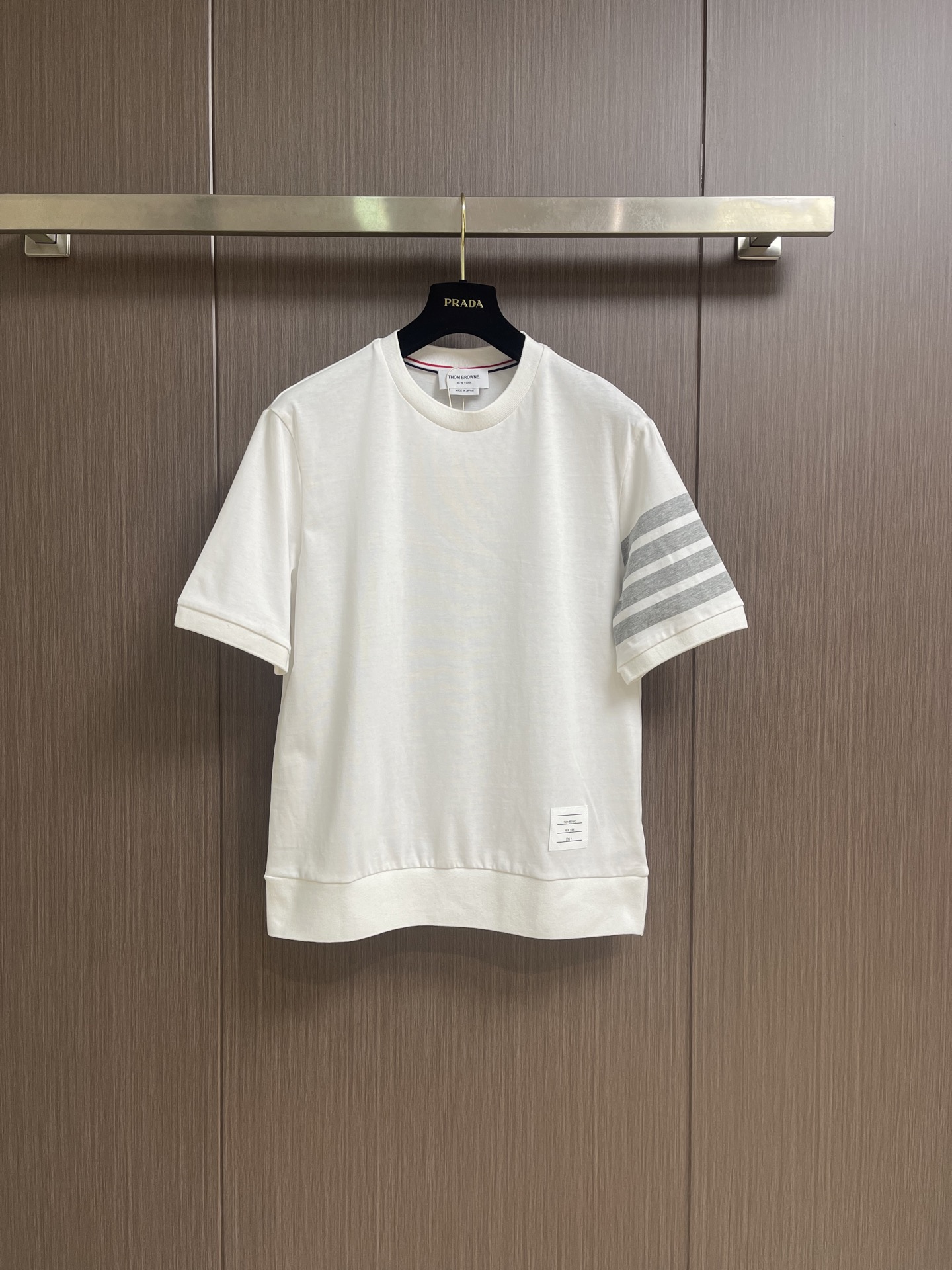 NO:847399,THOM BROWNE  Short-sleeved T-shirt with four stripes on the sleeves and arms. This T-shirt is made of 230g high-weight combed cotton knitted fabric. The surface of the fabric presents a delicate and full honeycomb texture. It feels soft and skin-friendly and has excellent breathability. It will not loosen and deform easily after being worn for a long time. The body is thin  The stitching is extremely elegant. The classic four-stripe logo on the left arm is made of high-end jacquard technology. The contrasting lines are sharp and clear, and the transition is natural and without overflowing colors. The neckline is made of warm and lustrous mother-of-pearl shell buttons, and the inner lining of the neckline is supplemented by red, white and blue three-color webbing for reinforcement.  , it is both iconic and effectively prevents neckline deformation. The placket and shoulder seams are made of double-needle hemming technology, and the stitches are fine, even and neat without losing threads; the hem adopts a classic arc design with short front and long back, and the slits on both sides are decorated with two metal buttons on each side.  It is equipped with the iconic red, white and blue webbing backing, and the brand's exclusive small logo is sewn on the inside of the hem. Every craftsmanship detail demonstrates the exquisite craftsmanship and high-end texture of high-quality garments. The overall routing is straight and delicate, the fabric is comfortable and soft, and the color is consistent with no color difference.  It can be matched with the same style to create a fashionable look, and can be used in various occasions. Customized accessories, complete with three standards, same style for men and women!  Size 1-2-3-4 1 size bust 104 shoulder width 45 length 69 size 2 bust 108 shoulder width 46 length 70 3 size bust 112 shoulder width 47 length 71 4 size bust 116 shoulder width 48 length 72,, T-shirt, tees, t-shirt,19860909THOM BROWNE 袖臂四条杠短袖T恤,这款T恤甄选230g高克重精梳棉针织面料,面料表面呈现细腻饱满的蜂巢肌理,触感软糯亲肤且具备优异的透气性,久穿不易松垮变形.衣身细节极尽考究,左臂经典的四道杠标识采用高端提花工艺,撞色线条利落分明,过渡自然无溢色；领口甄选温润光泽的珍珠母贝壳扣,领口内里辅以红白蓝三色织带包边加固,既具标志性又有效防止领口变形,门襟与肩缝处均采用双针锁边工艺,线迹细密均匀工整不脱线；下摆采用前短后长的经典弧形设计,两侧开衩处各缀两粒金属纽扣,搭配标志性红白蓝织带衬底,下摆内侧缝制品牌专属小标,每一处工艺细节都彰显出高品质成衣的精湛匠心与高级质感.整体走线平直细腻,面料舒适柔软,颜色一致无色差 能与同款搭配营造时尚造型,驾驭各种场合,定制辅料,三标齐全,男女同款！尺码1-2-3-4 1码 胸围104肩宽45 衣长69 2码 胸围108肩宽46 衣长70 3码 胸围112 肩宽47 衣长71 4码 胸围116 肩宽48 衣长72,,T-shirt,tees，t-shirt,,Men's clothing