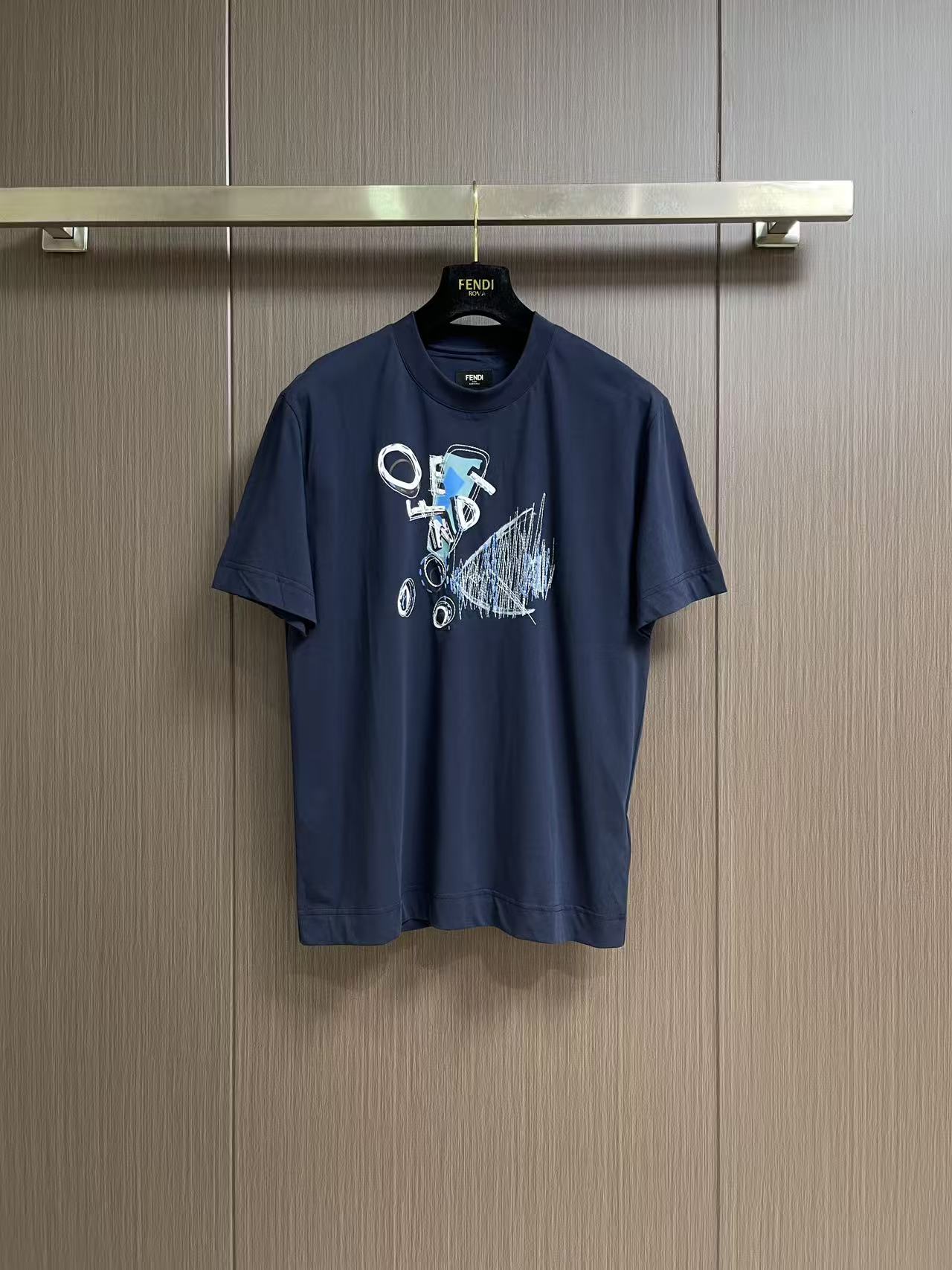 NO:856312,Fendi  The goldfish print embroidery round neck short-sleeved T-shirt is made of 24-count double-sided knitting, 250gm pure cotton fabric, with 24-count 1×1 rib, 200gm. The 24-count double-sided knitting is a medium-to-high fine yarn count, the yarn is thin, and the cloth surface is delicate and smooth. The double-sided knitting structure consists of two front loops nested in each other.  , with a front-facing appearance on both sides. The weight of the fabric is in the medium-thick range, which gives the fabric a soft and crisp feel. It has the unique fluffy feel of double-sided knitting without losing the drape support, and the upper body is not soft. High color fastness reactive dye dyeing ensures that the dark blue color remains full after multiple washings.  The goldfish pattern on the front achieves the coexistence of two-dimensional colors and three-dimensional textures through environmentally friendly elastic glue + dot printing and the precise cooperation of printed multi-color rice grain embroidery. The water-based polyurethane-based printing slurry forms a film with a very high elongation at break after curing, and can be stretched synchronously with the expansion of double-sided knitting.  It will not crack after repeated washing. Dot printing transfers the slurry to the fabric in the form of micron-level dots through a high-mesh screen plate, which can achieve photo-level grayscale gradient and half-tone effects, avoiding the common color block faults of glue printing. The overall wiring is straight and delicate, the fabric is comfortable and soft, and the color is consistent without color difference.  Can be matched with the same style to create a fashionable look, to suit various occasions, customized accessories, complete with three standards!  Size XS-L19860909Fendi 金鱼印绣圆领短袖t恤,选用了24支双面针织,250gm的纯棉面料,搭配24支1×1罗纹,200gm.24支双面针织属于中高细纱支,纱线较细,布面细腻光滑.双面针织结构由两个正面线圈相互嵌套,具有两面皆为正面的外观.面料克重属于中厚范围,赋予了面料柔软的挺括感；既有双面针织特有的蓬松手感,又不失垂坠支撑力,上身不软塌.高色牢度的反应性染料染色,确保深蓝色在多次洗涤后依然饱满.正面的金鱼图案通过环保弹力胶浆+网点印花与对印花多色米粒绣的精密配合,实现了平面色彩与立体肌理的共.水性聚氨酯基印花浆料,其固化后形成的薄膜断裂延伸率极高,能跟随双面针织的延展而同步拉伸,反复洗涤后不龟裂.网点印花通过高目数网版将浆料以微米级点阵形式转移到面料上,能够实现照片级的灰度渐变和半色调效果,避免了胶浆印花常见的色块断层.整体走线平直细腻,面料舒适柔软,颜色一致无色差 能与同款搭配营造时尚造型,驾驭各种场合,定制辅料,三标齐全！尺码XS-L XS码肩宽47 胸围104衣长69.5  S码肩宽48.5 胸围108衣长71.5  M码 肩宽50 胸围112衣长73.5 L码 肩宽51.5胸围116衣长75.5,,fendi,T-shirt,tees，t-shirt,,Men's clothing