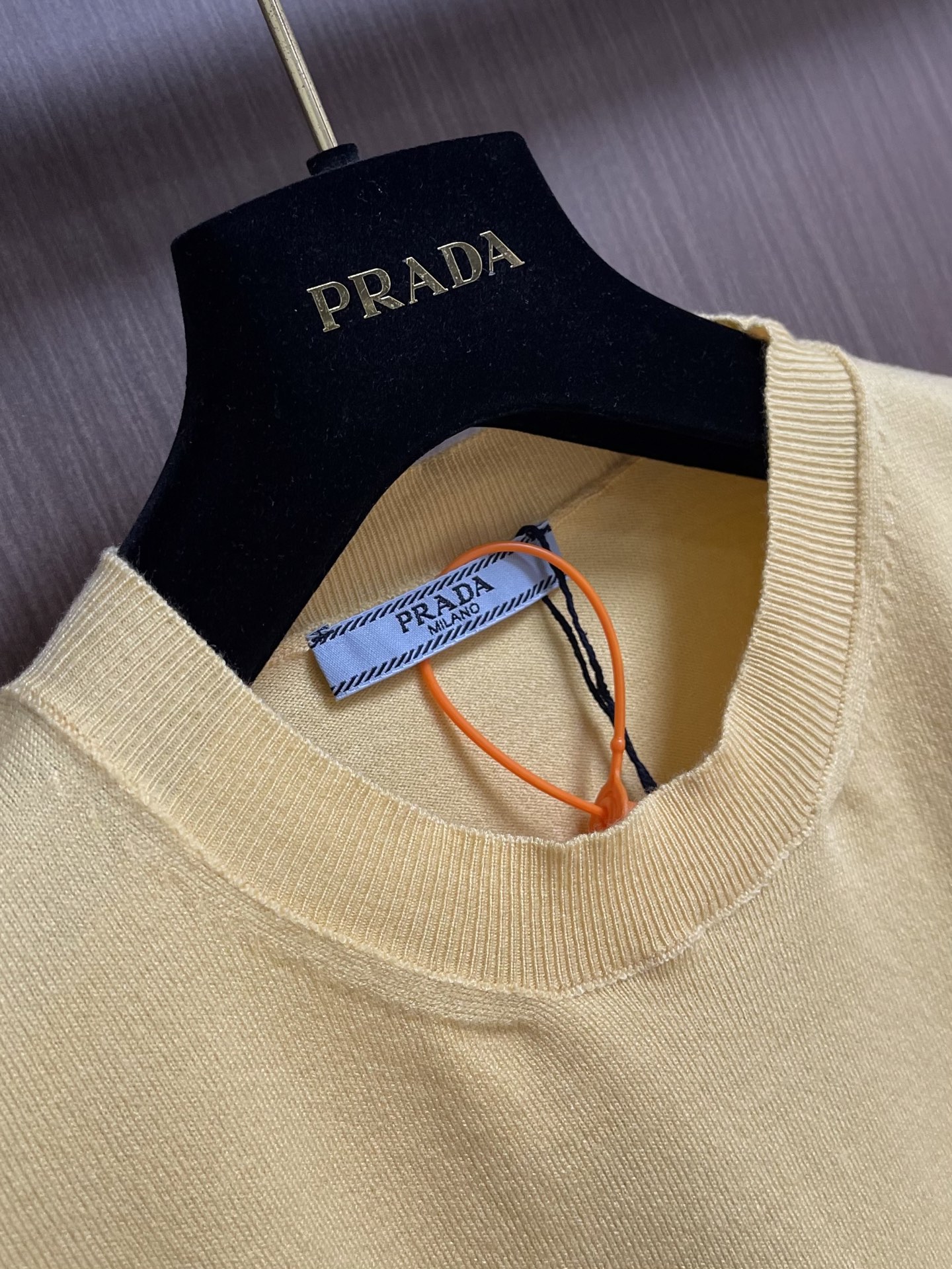 Prada 徽标嵌花圆领短袖针织毛衣，定织柔滑双股高密棉毛纱，柔软蓬松，舒适贴肤。以低饱和苋菜黄为基调，