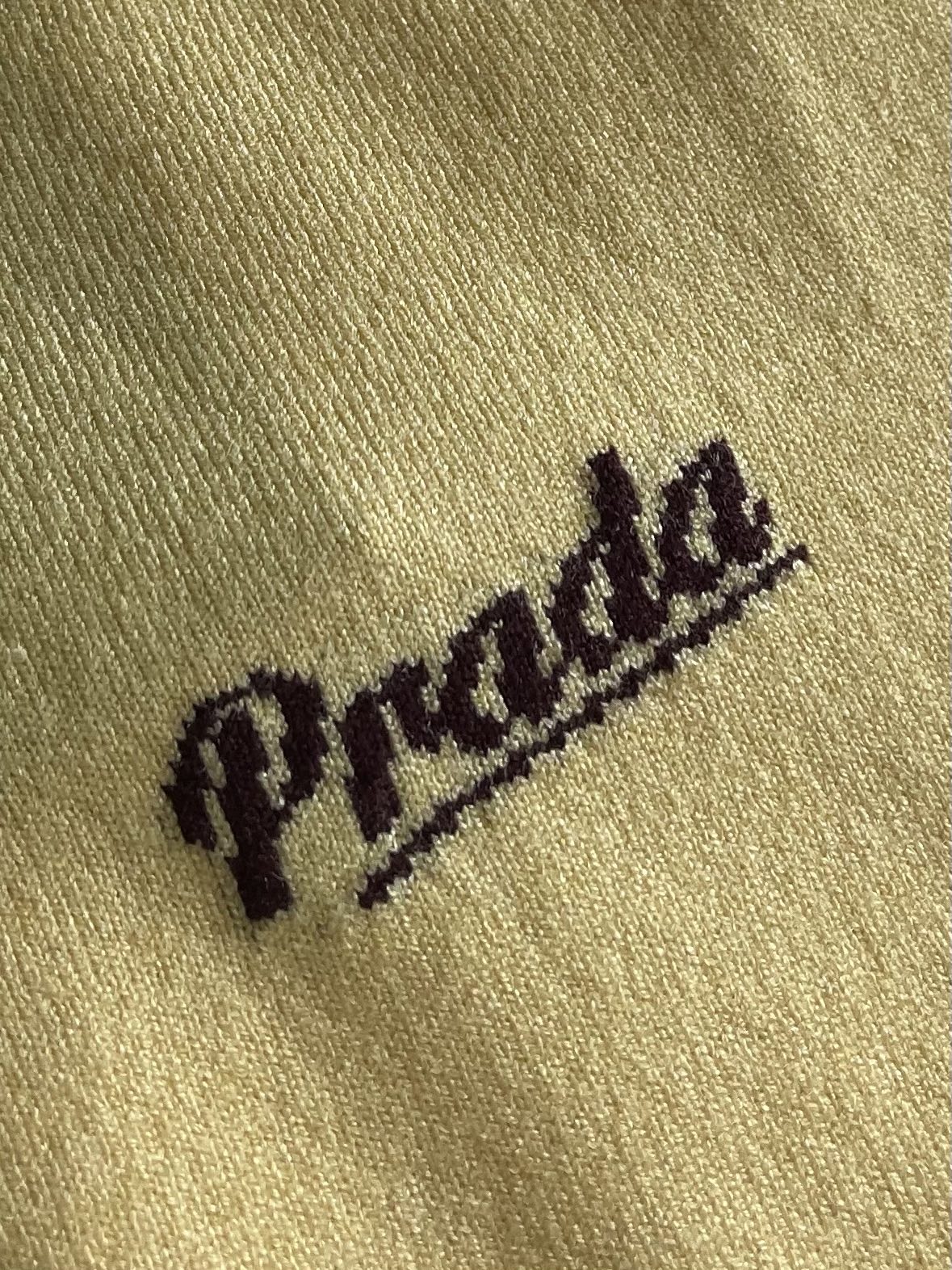Prada 徽标嵌花圆领短袖针织毛衣，定织柔滑双股高密棉毛纱，柔软蓬松，舒适贴肤。以低饱和苋菜黄为基调，