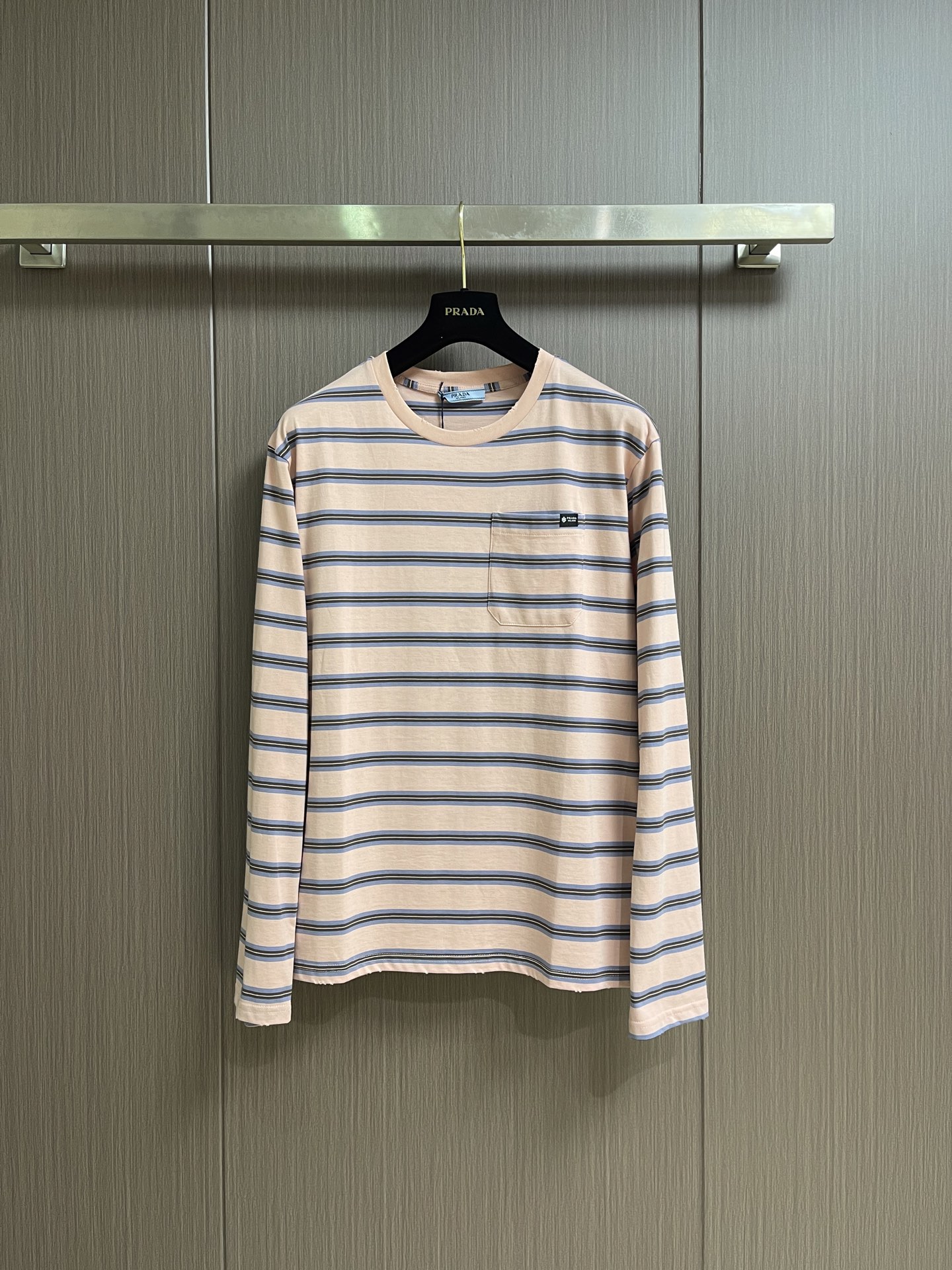NO:935727,Prada  Pink striped round neck long-sleeved T-shirt, the fabric shows the ultimate lightness in craftsmanship and texture. The compact spinning technology eliminates yarn hairiness through airflow concentration, making the yarn body smooth and round, and the surface of the fabric presents a delicate and high-end texture. The yarn-dying process is the core of this striped T-shirt; the yarn has been pre-dyed as required before weaving.  Blue, white and other colors are then interwoven into striped patterns through a knitting machine. This process is different from weaving first and then dyeing. The colored yarns are interwoven with each other during the weaving process. The stripe boundaries are clear and distinct, and the color fastness is higher. It is not easy to fade or smudge after washing. The 1×1 rib structure gives the fabric extremely high lateral elongation and resilience.  It can be stretched to more than 1.5 times its original length, and can be completely restored to its original shape after release. Positioning and sewing of the entire piece is the most technically difficult process of this T-shirt. The placement of each piece must be strictly aligned with the stripe pattern on the fabric to ensure that the stripes of the entire piece of clothing are continuous and complete after stitching. Cutting  All pieces must be cut in a single layer to ensure that the stripe position of each piece is accurate. When sewing, the stripes at side seams, shoulder seams, armholes and other joints must be completely aligned, which requires the sewing worker to make precise positioning and adjustments during sewing. The overall routing is straight and delicate, the fabric is comfortable and soft, and the colors are consistent without color difference.  Can be matched with the same style to create a fashionable look, to suit various occasions, customized accessories, complete with three standards!  Sizes XS-S-M-L19860909Prada 粉间条纹圆领长袖T恤,面料在工艺与质感上呈现出极致的轻盈感,紧密纺技术通过气流集聚消除纱线毛羽,使纱体光洁圆润,面料表面呈现细腻的高级质感.先染纱工艺是这款条纹T恤的核心；纱线在织造前已预先染成所需的蓝、白等颜色,再通过针织机交织成条纹图案.这种工艺与先织后染不同,色纱在织造过程中相互交织,条纹边界清晰分明,色彩牢度更高,水洗后不易褪色或晕染.1×1罗纹结构赋予了面料极高的横向延伸率与回弹力,横向可拉伸至原长的1.5倍以上,释放后能完全恢复原状.全件定位对线缝制是该款T恤最具技术难度的工艺环节,每一片裁片的摆放位置都必须严格对齐面料上的条纹图案,确保缝合后整件衣服的条纹是连续、完整的.裁剪时所有裁片必须单层裁剪,以保证每一片裁片的条纹位置精确无误.缝制时,侧缝、肩缝、袖窿等拼接处的条纹必须完全对齐,这要求缝纫工在车缝时进行精确的定位与调整.整体走线平直细腻,面料舒适柔软,颜色一致无色差 能与同款搭配营造时尚造型,驾驭各种场合,定制辅料,三标齐全！尺码XS-S-M-L XS码 衣长70 胸围104 肩宽49.0 S码 衣长72 胸围108 肩宽50.5 M码 衣长74 胸围112 肩宽52.0 L码 衣长76 胸围116 肩宽53.5,,prada,tees，t-shirt,,Men's clothing