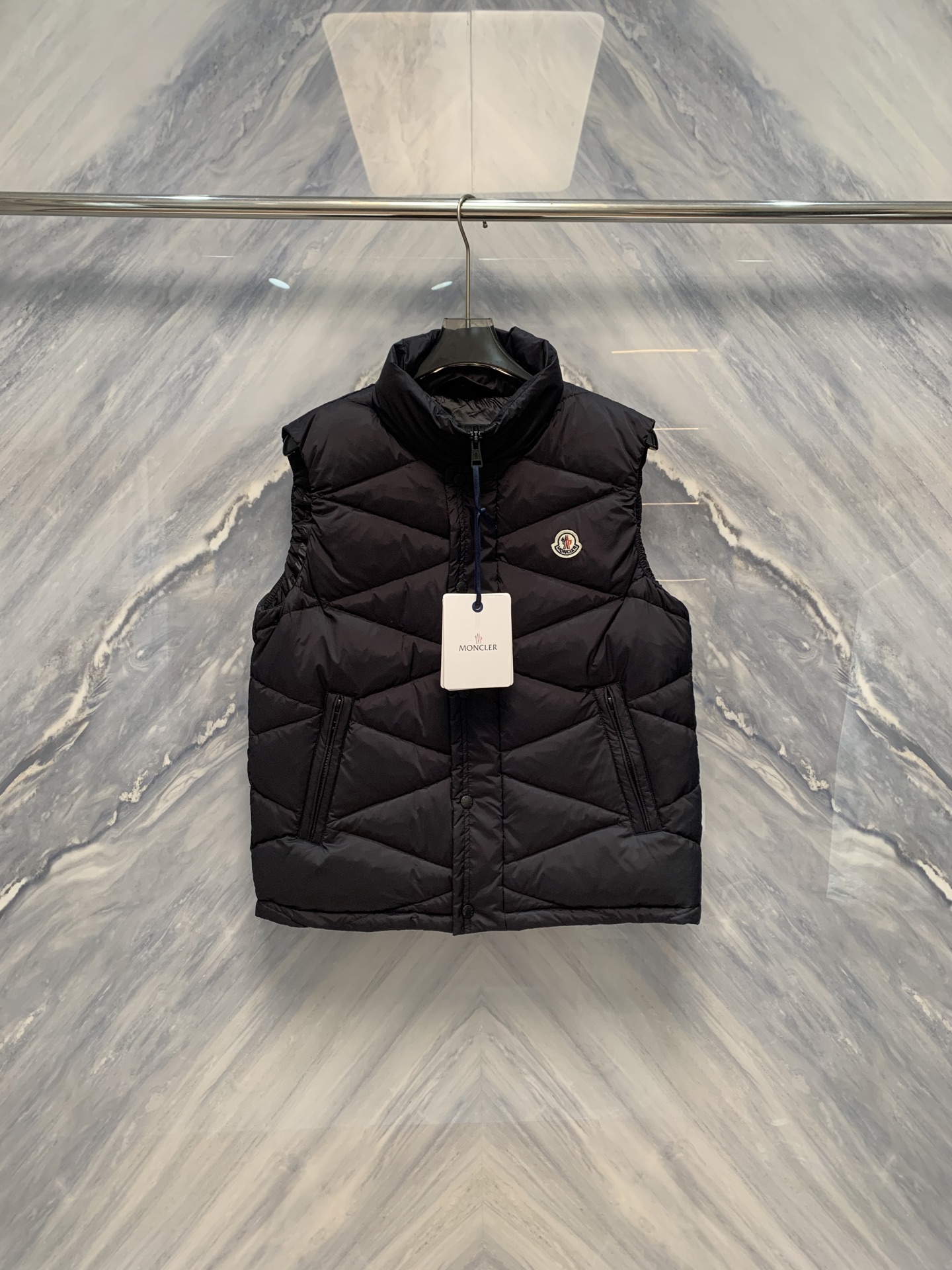 NO:608423,Diamond Realm M Men's Stand Collar Diamond Spliced Goose Down Vest In an extremely cold context, a top-quality vest is not only a barrier for the body, but also a precise crystallization of craftsmanship and aesthetics. This model of M Family's stand-up collar diamond spliced goose down vest is on sale at the same time.  The vest, with its architectural structural aesthetics and ultimate cold-proof technology, weaves the spirit of the Alps' ice and snow into every inch of fabric, creating a down art that can travel through the city and the wilderness. The vest uses M's iconic diamond-shaped quilting rectangle  Array, each grid is precisely calculated, the size is consistent, and the lines are as straight as a ruler, forming a three-dimensional geometric totem with great visual tension. The quilting depth is precisely controlled to ensure that the 90 high fill power European gray goose down is evenly distributed and eliminates cold spots.  .The fill power reaches 800+, it is as light as nothing, but it can lock in abundant warmth and achieve top thermal insulation performance. The inner liner is made of anti-drilling high-density velvet lining, which is treated with Swiss technology to prevent down from escaping. It feels silky and improves wearing comfort.  The outer fabric is made of Japan's Toray 'Gramart' microfiber technical cloth, 7D-grade ultra-thin fiber weaving, with a density close to the process limit, achieving a wearing experience as light as wings and as thin as cicada wings. The surface is treated with Teflon three-proof, waterproof, windproof, and anti-fouling, and rainwater will slip like beads, and wind will  The noise stops outside the fabric. The matte texture is calm and restrained, and the color is as deep as the midnight lake. It only emits a metallic shimmer under the light, highlighting low-key luxury. The stand-up collar design is straight and neat, fitting the curve of the neck, effectively resisting the cold wind. The collar is lined with skin-friendly velvet, which is warm to the touch. The front is double-sided.  The YKK waterproof zipper at the top opens and closes as smoothly as silk. The metal slider is frosted and integrated with the overall tone. The side seam has a hidden diagonal pocket, so that hands can be inserted naturally, which is warm and practical. The inside of the back collar is engraved with an exclusive metal nameplate for the M family. It is simple and unpretentious, with only the brand symbol and origin identification.  Talk about its orthodox origin. The whole garment is hand-sewn in a European workshop, each piece takes more than three hours, and the stitches are as fine as brocade. This vest is a geometric poem and a shield of down. It uses rhombus as its language and goose down as its soul. In the cold season, it covers the wearer with a light and unshakable dignity.  Color: Black Size: 1-5 1: Bust 112, Length 67, Shoulder Width 46 2: Bust 116, Length 68, Shoulder Width 47 3: Bust 120, Length 69, Shoulder Width 48 4: Bust 124, Length 70, Shoulder Width 49 5: Bust 128, Length 71, Shoulder Width 50,,down jacket,alexander wang19860909菱形之境M家男士立领菱形拼接鹅绒马甲在极寒的语境中,一件顶级马甲不仅是躯体的屏障,更是工艺与美学的精密结晶.M家此款柜台同步在售立领菱形拼接鹅绒马甲,以建筑般的结构美学与极致的御寒科技,将阿尔卑斯的冰雪精神织入每一寸面料,成就一件可穿行于都市与旷野的羽绒艺术.马甲采用M家标志性的菱形绗缝矩阵,每一格皆经精密计算,大小一致,线条笔直如尺量,构成极具视觉张力的立体几何图腾.绗缝深度精准控制,确保90高蓬松度欧洲灰鹅绒均匀分布,杜绝冷点.蓬松度达800+,轻若无物,却能锁住丰沛暖流,实现顶级保暖效能.内胆采用防钻绒高密里布,经瑞士技术处理,杜绝羽绒外逸,触感如丝,提升穿着舒适度. 外层面料选用日本东丽“Gramart”超细纤维科技布,7D级超薄纤维编织,密度接近工艺极限,实现轻盈如翼、薄如蝉翼的穿着体验.表面经特氟龙三防处理,防水、防风、防污,雨水滑落如珠,风噪止于布外.哑光质感沉静内敛,色泽深邃如午夜湖面,仅在光线下流转出金属般的微光,彰显低调奢华.立领设计挺拔利落,贴合颈部曲线,有效抵御寒风侵袭.领口内衬亲肤绒布,触感温润.前襟采用双头YKK防水拉链,开合顺滑如丝,金属拉头经磨砂处理,与整体色调浑然一体.侧缝暗藏斜插口袋,手可自然深入,保暖实用.后领内侧,镌刻M家专属金属铭牌,简约无华,仅以品牌符号与产地标识,诉说其正统血统.整衣于欧洲工坊手工缝制,每件耗时逾三小时,针脚细密如织锦.此马甲,是几何的诗,是羽绒的盾.它以菱形为语言,以鹅绒为魂,在寒冷季节里,为穿着者披上一件轻盈而不可撼动的尊严. 颜色:黑色 尺寸:1-5 1:胸围112 衣长67 肩宽46 2:胸围116 衣长68 肩宽47 3:胸围120 衣长69 肩宽48 4:胸围124 衣长70 肩宽49 5:胸围128 衣长71 肩宽50,,down jacket,alexander wang,Men's clothing