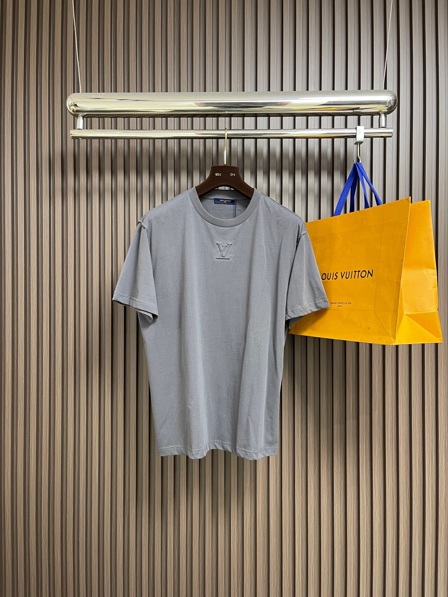 NO:597851,LV concave and embossed round neck short-sleeved T-shirt. The main body is made of 24S special compact cotton to make plain knitted fabric, with a weight of 180g. The high-count combed cotton yarn eliminates most of the short hairiness through the compact spinning process, making the yarn smoother and stronger. The woven fabric structure is extremely dense, flat and soft, with excellent anti-pilling ability and durability, while retaining the natural advantages of pure cotton, breathable and skin-friendly. The neckline is made of 32S  1x1 rib  Weighing 300g, the finer yarn count creates a more delicate and tight thread, which provides better elasticity and deformation resistance than ordinary ribs, ensuring that the neckline can still remain crisp after being put on and taken off many times. It contains an innovative process of silicone lining, and the concave and convex embossing process is heated and shaped by the upper and lower dies, and the rollers press the fabric at a certain temperature, and the production is completed through mechanical embossing.  It creates a three-dimensional layered convex surface. This makes the embroidered pattern not only three-dimensional and full, but also has a unique soft and elastic touch, which is completely different from traditional stiff embroidery. The support of silicone also ensures that the pattern is not easy to wrinkle and deform after washing, achieving a combination of visual novelty and process durability. The overall wiring is straight and delicate, the fabric is comfortable and soft, and the color is consistent without color difference.  It can be matched with the same style to create a fashionable look, and can be used in various occasions. Customized accessories, complete with three standards, same style for men and women!  Size XS-L,,louis vuitton,T-shirt,tees,t-shirt,alexander wang19860909LV 凹凸压花圆领短袖T恤,主体采用24S特纺紧密棉打造平纹针织面料,克重180g.高支数的精梳棉纱通过紧密纺工艺消除了大部分来短毛羽,使得纱线更光滑、强韧.织成的面料结构异常密实、平整且柔软,具有出色的抗起球能力和耐用性,同时保留了纯棉透气亲肤的天然优势.领口则选用32S 1x1罗纹 克重300g,更细的纱支编织出更细腻紧密的螺纹,提供了优于普通罗纹的回弹性与抗变形能力,确保领口历经多次穿脱后仍能保持挺括.内含硅胶衬垫的创新工艺,凹凸压花工艺由上下模加热定型,轧辊在一定温度下压轧织物,通过机械压印来完成产生立体层次凸面.这使得绣出的图案不仅立体饱满,而且触感具有独特的柔软弹性,与传统的硬挺刺绣截然不同.硅胶的支撑也保证了图案洗涤后不易褶皱变形,实现了视觉新颖性与工艺耐用性的结合.整体走线平直细腻,面料舒适柔软,颜色一致无色差 能与同款搭配营造时尚造型,驾驭各种场合,定制辅料,三标齐全,男女同款！尺码XS-L,,louis vuitton,T-shirt,tees，t-shirt,alexander wang,Men's clothing