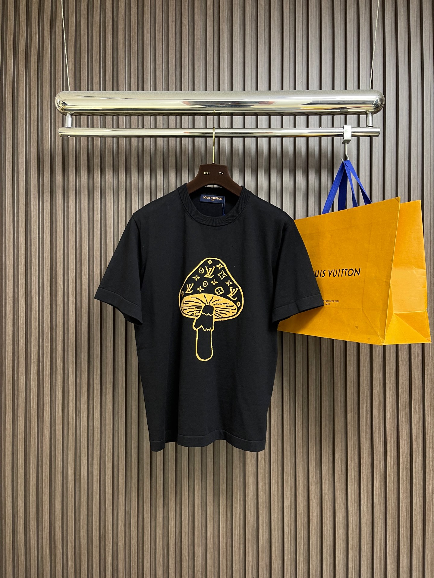 NO:597862,LV  Mushroom knitted intarsia round neck short-sleeved T-shirt. The T-shirt is made of high-quality knitted fabric, with a soft and crisp texture. The black warp adjustment is versatile. The round neck structure is precision seamed and the collar fits the neck and is not easy to deform. The mushroom pattern on the front is made of jacquard knitting technology, and the golden silk thread is in line with the brand's classic  The classic logo is integrated, and the texture is three-dimensional and delicate, highlighting the brand's high recognition. The body is sewn using industrial-grade flat stitching technology, the stitches are smooth and even, and the stitching at the hem and cuffs is fine and firm. From the selection of knitted fabrics to the process control of jacquard patterns, every process embodies Louis  Vuitton's pursuit of technological precision and creative design not only retains the daily practicality of T-shirts, but also shows the brand's light luxury recognition through unique jacquards. It is a fusion of knitting technology and fashion design. The overall routing is straight and delicate, the fabric is comfortable and soft, and the colors are consistent without color difference. It can be matched with the same style to create a fashionable look and control various occasions. Customized accessories, complete three labels, the same style for men and women!  Size S-XL,,louis vuitton,louis vuitton,T-shirt,tees,t-shirt,alexander wang19860909LV 蘑菇针织嵌花圆领短袖T恤,该T恤选用高品质针织面料,质地柔软且挺括,黑色调经百搭.圆领结构经精密锁边工艺,领口贴合颈部且不易变形.正面蘑菇图案采用提花针织工艺,金色丝线与品牌经典标识融合,纹理立体细腻,彰显品牌高辨识度.衣身车缝采用工业级平缝工艺,线迹平整均匀,下摆与袖口处针距细密牢固.从针织面料的甄选到提花图案的工艺把控,每一道工序都体现Louis Vuitton对工艺精度与创意设计的追求,既保留T恤的日常实穿性,又通过独特提花展现品牌的轻奢辨识度,是针织工艺与时尚设计的融合之作.整体走线平直细腻,面料舒适柔软,颜色一致无色差 能与同款搭配营造时尚造型,驾驭各种场合,定制辅料,三标齐全,男女同款！尺码S-XL,,louis vuitton,louis vuitton,T-shirt,tees，t-shirt,alexander wang,Men's clothing