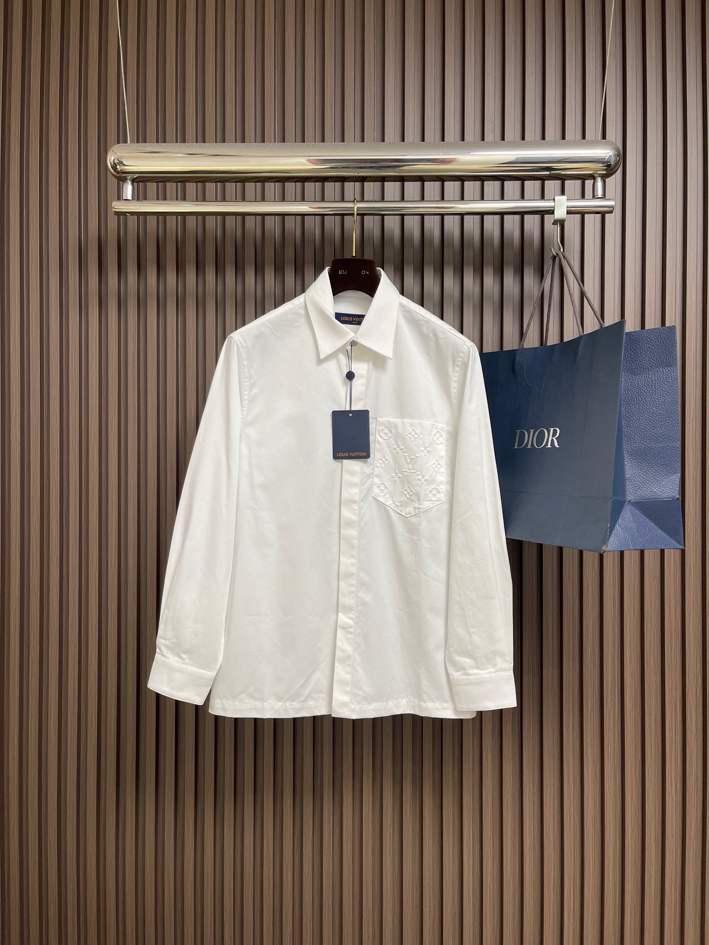 NO:611545,LV  Embossed pocket lapel long-sleeved shirt, twill woven fabric, standard version of peak lapel, hidden front placket, pearlescent buttons at the top, equipped with base, chest pocket with logo embossing, obvious twill texture on the front of the fabric, blurred on the back. Single yarn is used in both the warp and weft directions, the thread density is similar, the warp density of the fabric is slightly higher than the weft density, and the hand feel is relatively soft  Soft. The fabric has excellent stability, is not easy to deform, and prevents bulging; cotton fiber has good hygroscopicity, which keeps the fabric in a water balance state, making people feel comfortable and adding to the sophistication of the fabric. The concave and convex embossing process is heated and shaped by the upper and lower dies, and the rollers press the fabric at a certain temperature, and the production is completed through mechanical embossing.  Produce three-dimensional hierarchical convex surface. The fabric produces a concave and convex pattern with a relief-style three-dimensional effect and a special gloss effect. The three-dimensional shape, pattern and text have a strong three-dimensional effect, adding a decorative art effect, with clear layers, concentrated three-dimensional image, and accurate perspective angle. The collar can be adjusted with buttons for tightness.  Formal feeling and comfort; rear pleats and tabs are classic shirting techniques. The pleats provide additional room for movement, and the ribbons can maintain the shape of the shirt when hanging. The button front adopts custom buttons with matching positioning. These details together ensure the practical function and crisp shape of the shirt. Sizes XS-L, Louis  vuitton,shirts,alexander wang19860909LV 压花口袋翻领长袖衬衫,斜纹梭织面料、翻尖领标准版型、隐藏式前襟、顶端珠光纽扣、配有底座、胸袋呈现标识压纹、织物正面斜纹纹路明显,反面比较模糊.经纬向均用单纱,线密度接近,织物经密略高于纬密,手感比较柔软.面料具有极好的稳定性,不易变形、防鼓包；棉纤维具有较好的吸湿性,使织物保持水平衡状态,使人感觉舒适,增添了面料的精致度.凹凸压花工艺由上下模加热定型,轧辊在一定温度下压轧织物,通过机械压印来完成产生立体层次凸面.织物产生具有浮雕风格的立体效应和特别的光泽效果的凹凸花纹的工艺,制作立体造型图案文字有较强的立体感,增添装饰艺术效果,层次清晰、立体形象浓缩、透视角度准确.衣领可通过纽扣调节松紧,兼顾正式感与舒适度；后部褶裥与袢带是经典衬衫工艺,褶裥提供额外的活动余量,祥带则可在悬挂时保持衬衫形态.纽扣前襟选用定位相符的定制纽扣,这些细节共同确保了衬衫的实用功能与挺括造型.尺码XS-L,,louis vuitton,shirts,alexander wang,Men's clothing