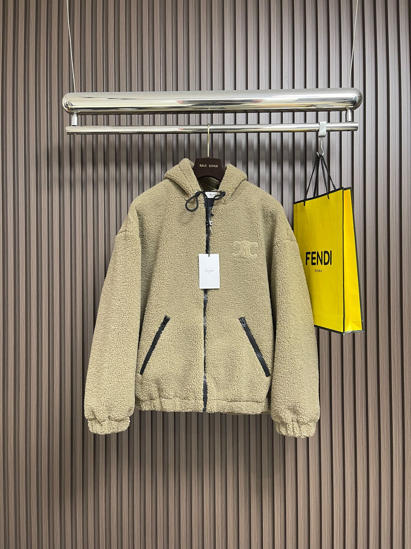 NO:613775,Celine  The suede hooded jacket decorated with the brand logo is made of polyester filament and is knitted through a circular knitting machine. The warp and weft yarns are woven into each other into a double-sided knitted structure. The front and back are flat coils. The fabric is formed after a series of processes such as dyeing, raising, carding, shearing, and polarization. The suede texture is soft.  The fiber characteristics make it almost non-absorbent, and can quickly drain sweat to the outer layer of the fabric and evaporate quickly, maintaining good breathability. The suede surface can lock the air and form a stagnant air layer around the body, effectively preventing heat loss and providing good thermal insulation performance. The inner quilting adopts a quilted cannage pattern, which is precisely adjusted by the seamstress.  The speed and stitch density of the machine make the stitches smooth and even during operation. After completion, regular diagonal quilting lines are formed, which inadvertently improves the overall texture when putting on and taking off. The embroidery patch tightly fixes the fabric and padding material to the frame of the embroidery machine, and the embroidery machine uses sparser stitches along the pattern of the padding layer.  Outline the filling area of the pattern, then run the pattern of the overlay, and use dense stitches to perfectly cover the foam padding layer to form a slightly raised Arc de Triomphe shape. After the final finishing, the edges of the patch are burr-free and the pattern is clear. Sizes S-XL, celine, jackets  & coats,hats,alexander wang19860909Celine 饰品牌标识仔章绒面连帽外套,面料选择涤纶长丝通过针织圆机,将经纱和纬纱相互圈套编织成双面针织结构,正面和背面都是平整的线圈.再通过染色、起毛、梳毛、剪毛、摇粒等一系列流程之后形成的面料.绒面质地柔软,纤维特性使其几乎不吸水,能将汗迅速排到面料外层并快速蒸发,保持良好的透气性.绒面能锁住空气,再身体周围形成一层不流动的空气层,有效防止热量流失,起到良好的保暖性能.内里绗缝采用绗缝藤格纹,缝纫师精确调整机器的速度和针脚密度,作业中线迹平滑、均匀.完成之后形成具有规则的斜向绗缝线条,穿脱时不经意间提升整体质感.绣花贴饰将面料和垫衬材料一同紧绷地固定在绣花机框架上,绣花机沿着垫衬层的版迹运用较稀疏的针迹勾勒出图案的填充区域,紧接着运行覆盖层的版迹,用密集的针迹完美地覆盖在泡沫垫衬层之上,从而形成微凸起的凯旋门形状.最后通过整理之后,贴饰边缘无毛刺,图案清晰.尺码S-XL,,celine,jackets & coats,hats,alexander wang,Men's clothing