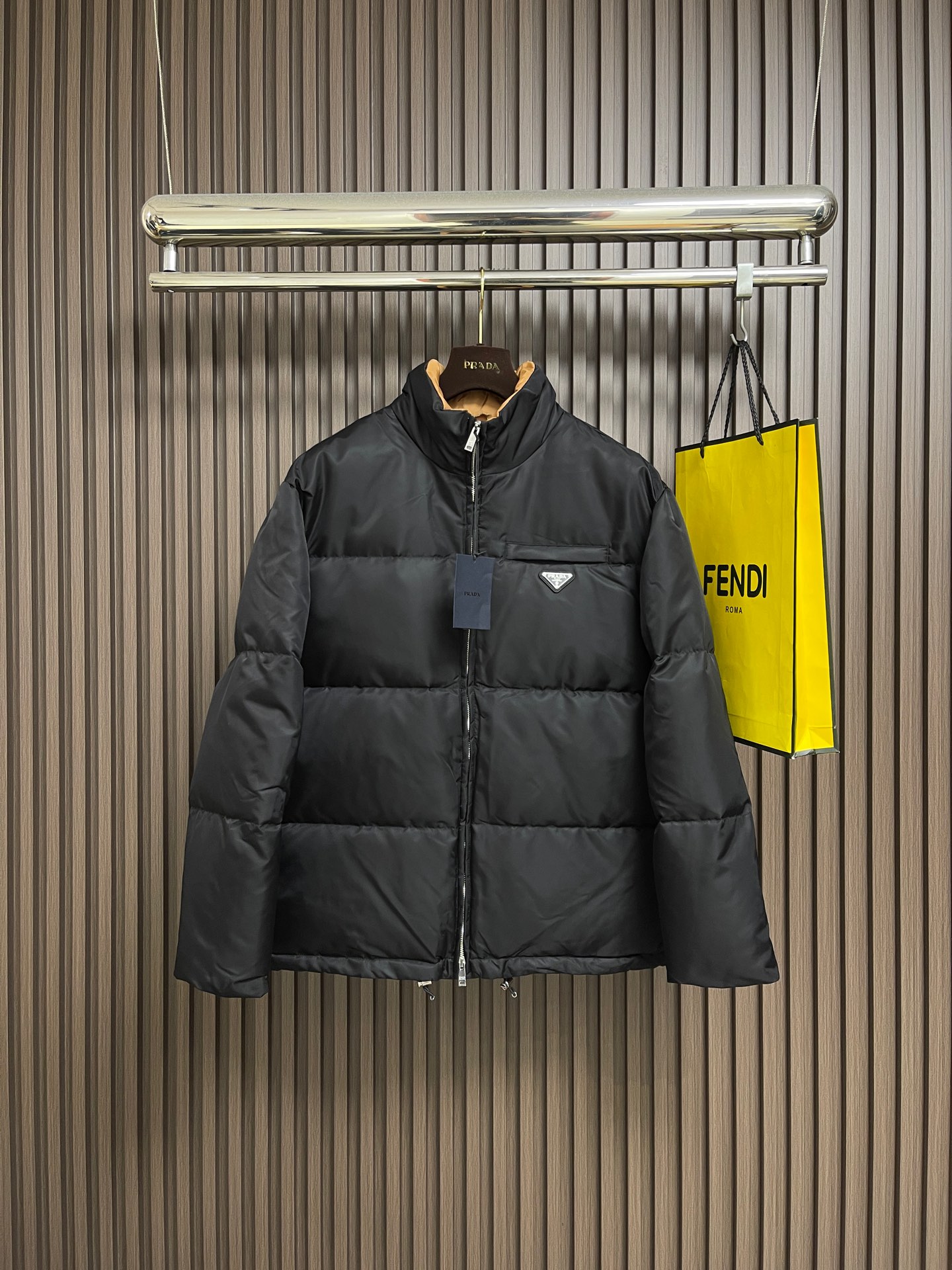 NO:606907,Prada The nylon color-blocked stand-collar down jacket is made of regenerated nylon fabric made of nylon. It is woven into a tight and tough fabric through advanced textile technology. It improves the strength of the frame and effectively blocks the invasion of cold wind and locks in the warm air generated by the down layer. After tight weaving and special processing, it is waterproof and windproof. The surface forms a certain lotus leaf effect, is wrinkle-resistant and not easy to deform, and is easy to take care of daily. The inner lining is made of polyamide woven polyamide. The sugar-brown nylon fabric forms a strong color contrast when folded, just like the molten gold of the setting sun is injected into the deep night sky. Polyamide fiber is known for its extremely high strength and excellent skin-friendly feel. It feels silky and smooth, which avoids the need for heavy wear. Possible friction and discomfort. It works together with the outer nylon to create a breathable, temperature-locking, and extremely comfortable microclimate environment, allowing warmth and care to be online at all times without feeling stuffy or restrictive. It is made of 90 white duck down , the fill power reaches g, ensuring excellent thermal insulation performance. After strict screening and processing, the velvet is not easy to velvet. 6 cm high stand-up collar cut, fits the neck line without oppression, and is as warm as a 'second skin' in the cold wind .The junction between the collar and the zipper adopts bevel splicing technology to avoid the rigid feeling of traditional stand-up collars and make it more flexible when turning the head. Built-in double-sided metal adjustment buckles in the hem can tighten the waistline by gently pulling it down, and restore the loose silhouette by lifting it up - commuting It is neat and slim when you are wearing it, and you are free and unrestrained when you are outdoors. The metal surface of the adjustment buckle is treated with PVD coating, which is wear-resistant and corrosion-resistant, and will last forever. A quilting machine is used to divide the fabric into 8 independent velvet grids, and the stitch length is strictly controlled at 3 stitches cm. The stitch error does not exceed 0.1mm. The sutures are made of high-strength nylon threads. The tensile force test reaches 20N (approximately 2kg load-bearing), which eliminates the risk of suture breakage. Sizes S-XL, prada, jackets & coats,down jacket,alexander wang19860909Prada 尼龙拼色立领外套羽绒服,选用锦纶制成的再生尼龙面料,通过先进的纺织技术,编织成紧密且坚韧的布料,提升骨架强度有效阻挡冷风侵袭,锁住羽绒层产生的暖空气,经过紧密的编织工艺和特殊处理之后使其具备防水防风等功能,表面形成一定的荷叶效应,同时抗皱不易变形,易于日常打理.内衬采用了聚酰胺编织而成的焦糖棕色尼龙面料,翻折时形成强烈色彩对冲,宛如将落日熔金注入深邃夜空.聚酰胺纤维以其极高的强度与卓越的亲肤感著称,触感如丝般顺滑,避免了穿着厚重时可能产生的摩擦不适.它与外层尼龙协同工作,共同构建了一个透气、锁温、且极度舒适的微气候环境,让温暖呵护时刻在线,却毫无闷热与束缚感,选用90白鸭绒,蓬松度达g,确保保暖性能卓越.绒子经过严格筛选与处理之后,不易钻绒.6公分加高立领剪裁,贴合颈部线条却不压迫,,寒风中宛如'第二层肌肤'般温暖.领口与拉链衔接处采用斜角拼接工艺,避免传统立领的呆板感,转头时更显灵动.下摆内置双侧金属调节扣,轻轻下拉即可收紧腰线,上提则恢复宽松廓形﹣﹣通勤时利落修身,户外时自由无拘.调节扣金属表面经PVD镀层处理,耐磨抗腐蚀,历久弥新.采用绗缝机,将面料分割为8个独立绒格,针距严格控制在3针cm,线迹误差不超过0.1mm,缝线选用高强度尼龙线,拉力测试达20N（约2kg承重）,杜绝因缝线断裂导致的.尺码S-XL,,prada,jackets & coats,down jacket,alexander wang,Men's clothing