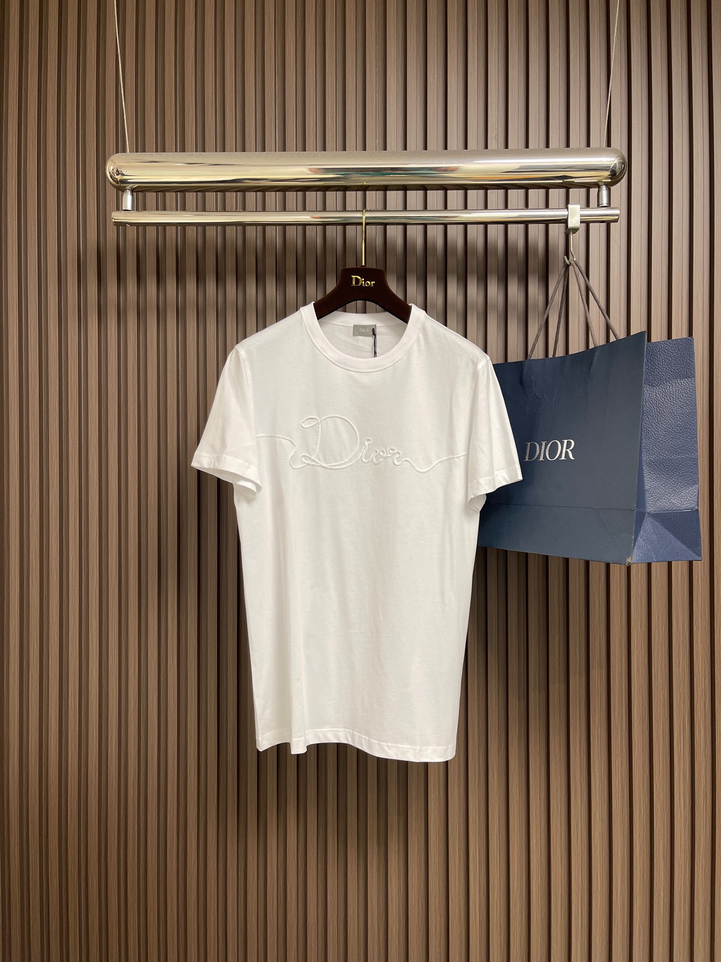 NO:606970,Dior  Satin emblem round neck short-sleeved T-shirt, the main body is made of 24-count special-spun compact cotton, 185gm2 is lightweight to medium, ensuring the lightness, breathability and good drape of the T-shirt. It is suitable for spring alone or as an inner layer. Paired with 32-count 1x1 Luo  texture, 300gm2. Its special spinning and compacting process means that compact spinning technology is used in the spinning process, which effectively reduces the hairiness of the yarn, making the yarn smoother and stronger. The woven fabric therefore has a tight structure, smooth surface, and is not easy to pilling.  Superior characteristics. The final dark gray tone is combined with the simple texture of plain knitting to present a high-end matte texture. The embroidery decoration in the form of a ribbon is specially processed through a process to fix the ribbon on the fabric. The texture brought by this process is usually different from  The woven texture and slight luster of the main knitted fabric form a delicate and accessible visual and tactile focus on the matte dark gray base, which enhances the craftsmanship and uniqueness of the item. The overall routing is straight and delicate, the fabric is comfortable and soft, and the color is consistent without color difference.  It can be matched with the same style to create a fashionable look, and can be used in various occasions. Customized accessories, complete with three standards, same style for men and women!  Size XS-L,,dior,T-shirt,tees,t-shirt,alexander wang19860909Dior 织缎徽章圆领短袖T恤,主体采用24支特纺紧密棉,185gm2的属于轻量至中等,确保了T恤的轻盈、透气与良好的垂坠感,既适合春季单穿,也适合作为内搭.搭配32支1x1罗纹,300gm2.其特种纺织与紧密工艺意味着在纺纱过程中使用了紧密纺技术,有效减少了纱线的毛羽,使纱线更光滑、强度更高.织成的面料因此具有结构紧密、表面光洁、不易起球的优越特性.最终的深灰色调与平纹针织的简约肌理相结合,呈现出一种高级的哑光质感.缎带形式的刺绣装饰,通过工艺特殊处理,使织带固定在面料上.这种工艺带来的质感通常是不同于主体针织面料的梭织质感与轻微光泽,在哑光的深灰色底上形成一个精致而触手可及的视觉与触觉焦点,提升了单品的工艺设计和独特性.整体走线平直细腻,面料舒适柔软,颜色一致无色差 能与同款搭配营造时尚造型,驾驭各种场合,定制辅料,三标齐全,男女同款！尺码XS-L,,dior,T-shirt,tees，t-shirt,alexander wang,Men's clothing