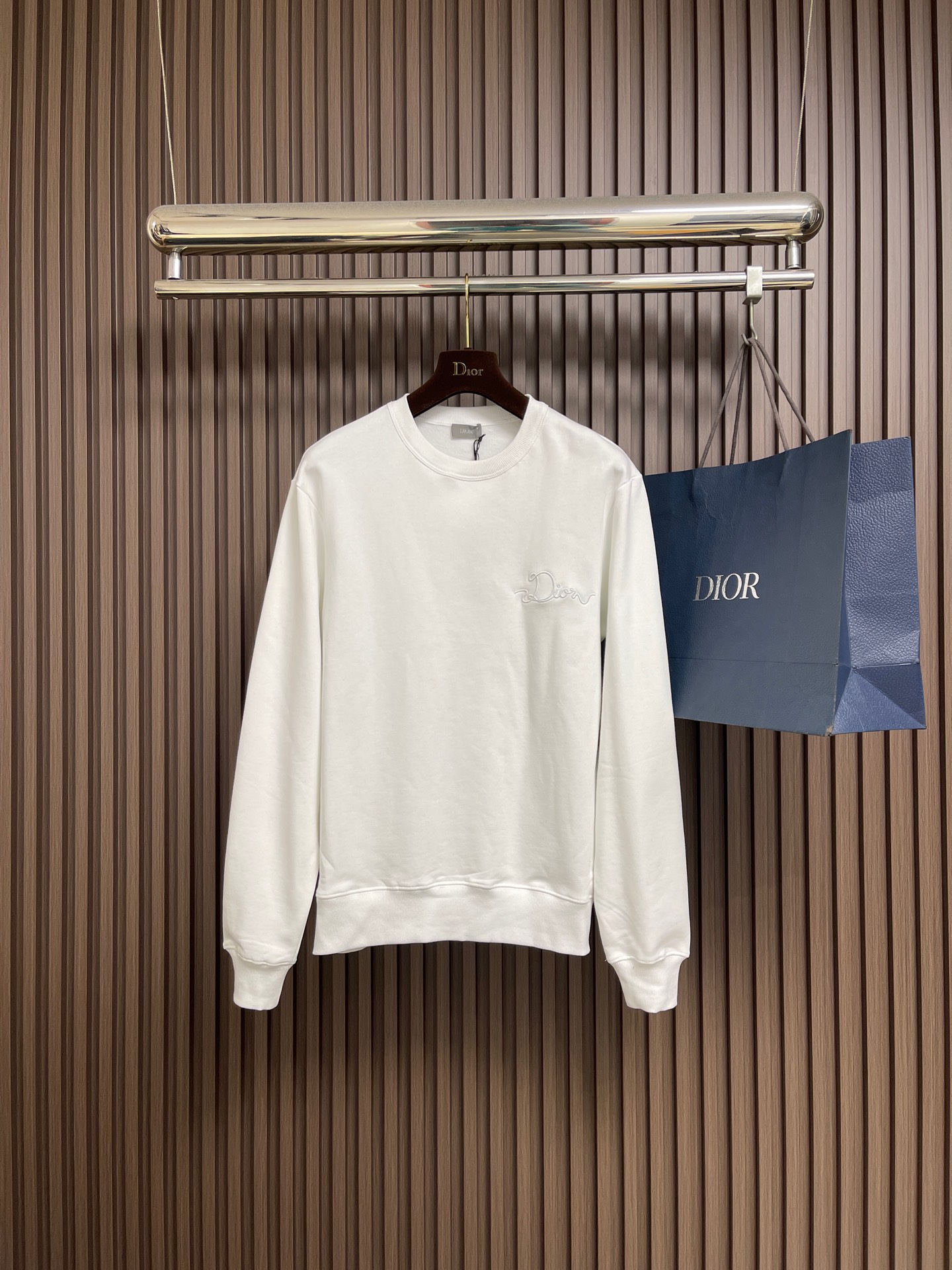 NO:609447,Dior CD Ribbon crew neck sweatshirt, new for the Spring 2026 collection, decorated with Ribbon  The logo pays tribute to the exquisite craftsmanship of the workshop. It is carefully made of white cotton fleece fabric, with ribbed round neck, cuffs and hem. The casual silhouette can be matched with the oversized version. It is made of a composite of 26-count double yarn top layer + 10-count bottom yarn terry  Structure, a uniform suede surface is formed on the inside through precision raising process, achieving a velvet-like skin-friendly touch. The heavy weight gives the fabric a sculpture-like stiffness, perfectly balancing the lazy silhouette and neat lines. The collar and cuffs are made of 21 2x2 reinforced ribs.  , a memory elastic mesh is formed by weaving in both warp and weft directions to ensure that the initial fit is maintained after multiple wears and takeoffs. The process uses laser-cut ribbons and micron-level hot-melt composite technology, and is processed through positioning embroidery. The edges achieve seamless fit with precision, and the decorative belt is fixed on the chest. Its luster forms a subtle light and shadow dialogue with the cotton matte base, and the detailed specifications are restored to the version. Sizes XS-L, dior, hoodie, sweatshirts, alexander  wang19860909Dior CD Ribbon 标志圆领卫衣,二零二六春季系列新品,饰以Ribbon 标志,向工坊的精湛工艺致敬.采用白色棉质起绒面料精心制作,搭配罗纹圆领、袖口和底边.休闲廓形,可与超大版型搭配.采用26支双纱面层＋10支底纱毛圈的复合结构,通过精密起绒工艺在内侧形成均匀绒面,实现天鹅绒般亲肤触感.重磅克重赋予面料雕塑般挺括感,完美平衡慵懒廓形与利落线条.领口袖口采用21支2x2强化罗纹,以经纬双向编织形成记忆弹性网,确保多次穿脱仍保持初始贴合度.工艺采用激光切割缎带与微米级热熔复合技术,通过定位刺绣工艺处理.边缘实现精度的无缝贴合,装饰带固定于前胸,其光泽与棉质哑光基底形成微妙的光影对话,对版还原细节规格.尺码XS-L,,dior,hoodie,sweatshirts,alexander wang,Men's clothing