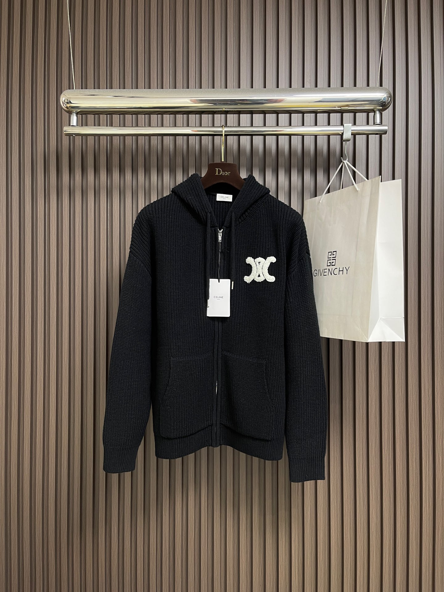 NO:624491,celine  Woolen hooded sweatshirt zipper knitted sweater, main knitted fabric, superfine merino wool, yarn count 26S2 (medium-thick knitting yarn), double-twisted to ensure the fabric is crisp and soft; combing process is used to remove short fibers, the surface is smooth and free of stray hairs, and the hand feels delicate and does not stick to the body. Through the mixed color spinning process (white  Color + dark gray fiber mixed in proportion) to achieve soft gray levels and avoid the monotony of solid colors. The collar, cuffs, and hem are 2x2 tight ribs, using high-elastic spandex) to ensure excellent resilience after stretching, not easy to deform, and fit the body curve. The main knitting process, flat knitting (Flat  Knitting) uses a computerized flat knitting machine (such as the Stoll CMS series) to knit the body and sleeves in one piece to reduce seams and improve comfort. The three-dimensional towel embroidery on the chest uses 8 strands of pure cotton towel thread for the white pattern. It is made with a 3D padded embroidery process through a computer embroidery machine. The stitch density is ≥120 stitches cm2, and the edges are embroidered with overlock (Satin).  Stitch) to close the edges to ensure that the pattern is full and three-dimensional and not easy to fluff. Positioning accuracy, the distance between the center of the pattern and the central axis of the zipper and the edge of the hem needs to be calibrated through the template, with an error of ≤0.5cm to ensure visual symmetry. Main body splicing, seamless  Joining) The main components such as the body and sleeves are knitted with a flat knitting machine. There are only a few seams at the armpits and shoulder lines. The seams are processed with a 3-needle five-thread overlock sewing machine. The seam width is ≤0.8cm. After the edges are trimmed, they are hot-pressed and shaped to ensure that the splices are flat and without bulges. The shoulders are reinforced on the inside of the shoulder line.  Sewn twill silk strips (length 15cm, width 1.5cm), hand-quilted and fixed to enhance the load-bearing capacity of the shoulders and prevent the shoulder line from sagging after long-term wear. Sizes S-XL, celine, hoodie, sweatshirts, sweaters, real  silk,hats,alexander wang19860909celine 毛织连帽卫衣拉链针织毛衣,主体针织面料,超细美利奴羊毛,纱线支数26S2（中粗针织纱）,双股并捻,确保面料挺括且柔软；采用精梳工艺去除短纤维,表面光洁无杂毛,手感细腻不扎身.通过混色纺纱工艺（白色＋深灰色纤维按比例混合）实现柔和的灰度层次,避免纯色单调感.领口、袖口、下摆处为2x2紧密罗纹,采用高弹氨纶）确保拉伸后回弹性能优异,不易变形,且贴合身体曲线.主体针织工艺,横机编织（Flat Knitting)采用电脑横机（如Stoll CMS系列）一体编织衣身、袖子,减少接缝提升舒适度.胸前刺绣立体毛巾绣 白色图案采用8股纯棉毛巾线,通过电脑绣花机以3D垫高绣工艺制作,针脚密度≥120针cm2,边缘用锁边绣(Satin Stitch）收边,确保图案饱满立体、不易起毛.定位精度,图案中心与拉链中轴线、下摆边缘的距离需通过模板校准,误差≤0.5cm,确保视觉对称.主体拼接,无骨缝接（Seamless Joining)衣身、袖子等主要部件采用横机一体编织,仅在腋下、肩线处有少量接缝,接缝处使用3针五线包缝机处理,缝份宽度≤0.8cm,边缘修剪后进行热压定型,确保拼接处平整无凸起.肩部加固肩线内侧加缝斜纹真丝衬条（长度15cm,宽度1.5cm),手工绗缝固定,增强肩部承重能力,防止久穿后肩线下垂.尺码S-XL,,celine,hoodie,sweatshirts,sweaters,real silk,hats,alexander wang,Men's clothing