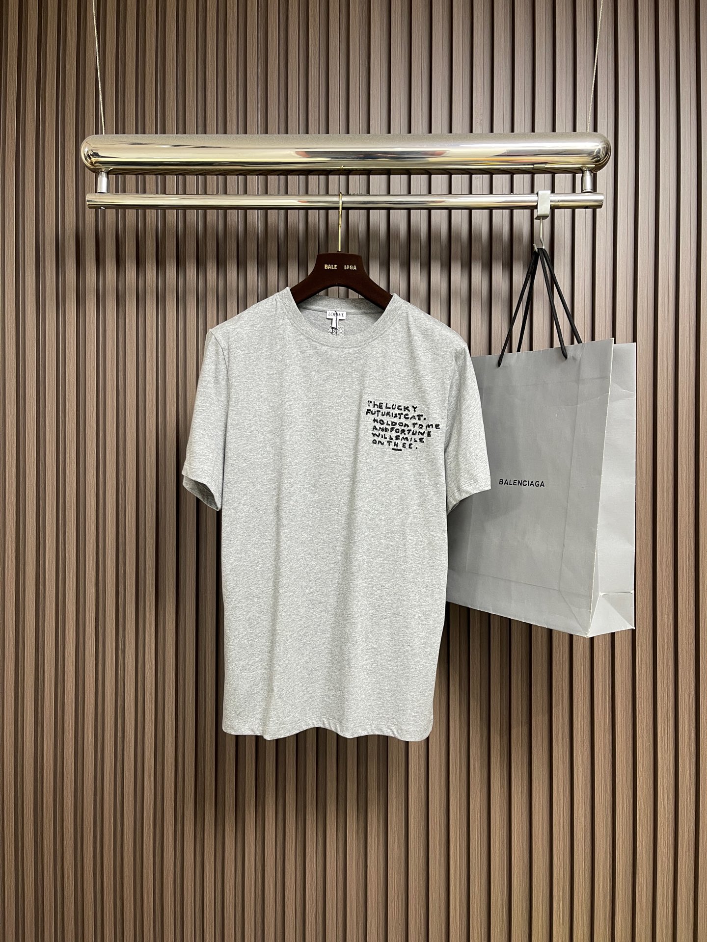 NO:646853,LOEWE  White cat floral gray round neck short-sleeved T-shirt, cotton jersey fabric. The main body is made of 24S special compact cotton to create a jersey fabric with a weight of 180g. The high-count combed cotton yarn eliminates most of the short hairiness through the compact spinning process, making the yarn smoother and stronger. The woven fabric structure is extremely dense, flat and soft, with excellent anti-pilling ability and durability, while retaining the natural advantages of pure cotton, breathable and skin-friendly. The neckline is made of 32S  1x1 rib  The weight is 300g, and the finer yarn count creates a more delicate and tight thread, which provides better elasticity and anti-deformation than ordinary ribs, ensuring that the neckline can still remain crisp after being put on and taken off many times. Multiple embroideries are combined, and the embroidered letters on the chest are chain embroidered.  The stitching is three-dimensional and full, with a unique woven texture and a soft touch; the craftsmanship ensures that the outline of the letters is clear, strong and durable. Its function is to highlight the brand or design theme on the front in a simple and exquisite way, and form a contrast between the primary and secondary and the traditional and simple with the more complex patterns on the back.  Futurist  Cat cross-stitch is a computer embroidery process that simulates traditional hand-made cross-stitch. A pixelated pattern is formed through the precise arrangement of countless 'X'-shaped stitches. Its function is to create a unique retro feel, a hand-made feel and a rich texture effect, forming an interesting space-time dialogue with the futuristic theme, giving the pattern profound artistic value and unique visual impact. Anagram embroidery uses three-dimensional embroidery technology, and is filled with multiple layers of embroidery thread to make the logo clear, full and protruding from the surface of the fabric. Classic trademark letters  Design, embroidery is fine and dense, the fonts are clear and have a strong sense of lines and three-dimensionality. Simple vertical round neck short-sleeved version, the pattern is developed to be extremely straight cut, the knitted material has certain stretchability, and the upper body will not be tight. The round neck is stitched with ribs of the same color at the neckline, and the back  The inner striping process of the collar effectively prevents the neckline from deforming after repeated wear and washing. The fitted shoulder line, bottom hem and cuffs are trimmed with special machines and open stitching. Sizes XS-L, loewe, T-shirt, tees, t-shirt, alexander  wang19860909LOEWE 白猫花灰圆领短袖T恤,棉质平纹针织面料,主体采用24S特纺紧密棉打造平纹针织面料,克重180g.高支数的精梳棉纱通过紧密纺工艺消除了大部分短毛羽,使得纱线更光滑、强韧.织成的面料结构异常密实、平整且柔软,具有出色的抗起球能力和耐用性,同时保留了纯棉透气亲肤的天然优势.领口则选用32S 1x1罗纹 克重300g,更细的纱支编织出更细腻紧密的螺纹,提供了优于普通罗纹的回弹性与抗变形能力,确保领口历经多次穿脱后仍能保持挺括.多刺绣结合处理,胸前的刺绣字母采用链式绣工艺,链式绣的线迹立体、饱满,带有独特的编织纹理,触感较为柔软；工艺处理确保字母轮廓清晰、牢固耐用.其作用在于以简洁而精致的方式在正面点明品牌或设计主题,与背面更复杂的图案形成主次和繁简的对比. Futurist Cat十字绣这是一种模拟传统手工十字绣的电脑刺绣工艺.通过无数个'X'形针脚的精确排列,来构成像素化的图案.它的作用是创造出独特的复古感、手工感和丰富的肌理效果,与未来主义主题形成有趣的时空对话,赋予图案深厚的艺术价值和独特的视觉冲击力.Anagram刺绣采用立体刺绣工艺,通过多层绣线填充,使标识清晰、饱满且凸出于面料表面.经典商标字母设计,刺绣精细针法绵密,字体清晰且线条感和立体感强.简约垂直圆领短袖版型,对版纸样开发极简直身剪裁,针织材质具有一定延展性能,上身不会紧紧束身.圆领同色罗纹拼接领口,后领口内贴条工艺,有效防止多次穿洗后领口变形,合身肩线,底摆与袖口专机坎车明线收边.尺码XS-L,,loewe,T-shirt,tees，t-shirt,alexander wang,Men's clothing