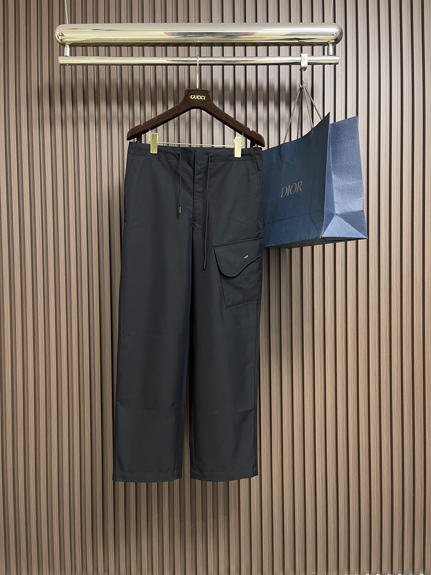 NO:744009,Dior  Black cotton twill overalls, made of a blend of double-ply combed cotton and polyester fiber, interwoven with the '31 right twill' weaving method. The twill angle is 45° and contains 8-10 weave points per centimeter, forming a fine and tight texture. The fabric weighs 280gm2 and is moderately thick but not bloated. The surface has been 'enzyme washed' to remove loose hair and give it a slightly aged texture.  .The hollow structure of cotton fiber accelerates air circulation, and combined with the breathable pores of twill weave, you will not feel stuffy and sweaty when wearing it in summer; the abrasion resistance of polyester fiber makes the fabric washable and durable, and it is not easy to pill and snag due to daily friction. There are three-dimensional saddle-shaped flap pockets on the outside of the trouser legs, with a smooth arc design. The edge of the flap adopts 'double-needle topstitching' technology, with even stitch spacing (10 stitches every 3cm), both  The reinforced edge forms a decorative line. The top of the flip cover is inlaid with the metal Dior logo in the center. It is made of zinc alloy and processed by electroplating process. It has a uniform color and is not easy to oxidize. The waist has a double-layer thickened waistband and a high-density nylon drawstring. The rope end is decorated with a metal bell, which can be pulled smoothly and is not easy to loosen. The tightness can be adjusted freely according to the waistline, taking into account comfort and fit, to avoid  The tightness of traditional overalls. The front placket adopts an invisible zipper, which is double-fastened with metal hooks. The zipper teeth are fine and smooth, and the zipper teeth are smooth and silent when pulled. The opening and closing are convenient and firm, ensuring that it is not easy to open accidentally during wearing. There are classic diagonal slit pockets on both sides of the trousers, and the edges of the pockets are made with 'edging + double needle' technology to prevent threading. Sizes 46-52,, dior,19860909Dior 黑色棉质斜纹工装裤,采用双股精梳棉与聚酯纤维混纺而成,经'31右斜纹'织法交织而成,斜纹角度45°,每厘米含8-10个织点,形成细密紧实的纹路.面料克重达280gm2,厚度适中却不臃肿,表面经'酵素水洗'处理,去除浮毛并赋予轻微做旧肌理.棉纤维的中空结构加速空气流通,配合斜纹织法的透气孔道,夏季穿着不闷汗；聚酯纤维的耐磨性使面料耐洗耐穿,日常摩擦不易起球勾丝.裤腿外侧缀立体马鞍形翻盖口袋,袋口呈流畅的弧形设计,翻盖边缘采用'双针明线'工艺,针距均匀（每3cm10针）,既加固边缘又形成装饰性线条.翻盖顶部中央镶嵌金属Dior标志,采用锌合金材质,经电镀工艺处理,色泽均匀,不易氧化.腰部内置双层加厚腰头,内藏高密度尼龙抽绳,绳头缀有金属吊钟,拉动顺畅且不易松脱.可根据腰围自由调节松紧,兼顾舒适与贴合,避免传统工装裤的紧绷感.前门襟采用隐形拉链,配合金属钩扣双重固定,拉链齿细密光滑,拉动时静音顺畅；开合便捷且牢固,确保穿着过程中不易意外敞开.裤身两侧为经典斜插式开缝口袋,袋口边缘采用'包边＋双针'工艺,防止脱线.尺码46-52,,dior,,Men's clothing