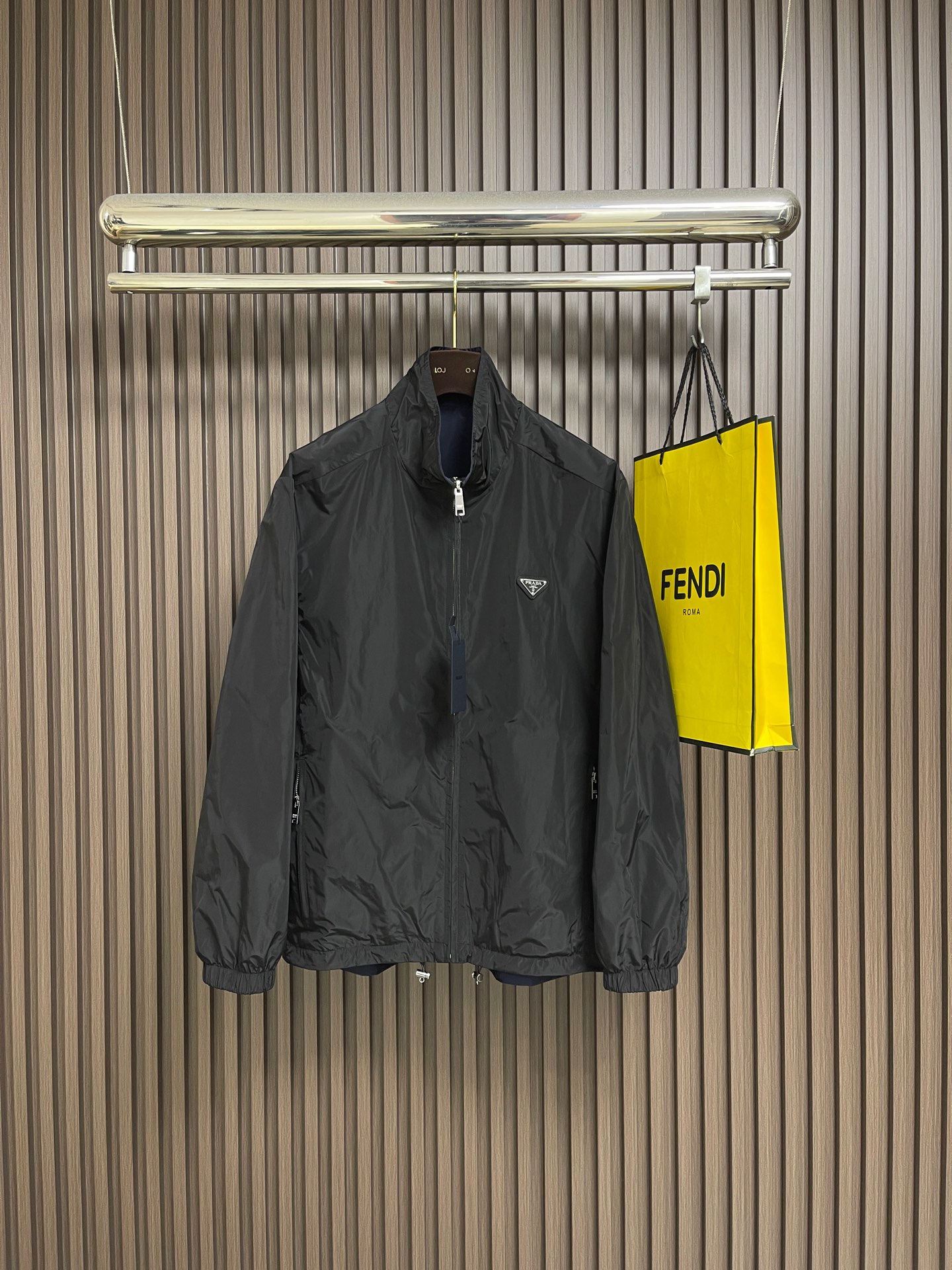 NO:759443,PRADA  The regenerated nylon double-sided stand-collar jacket is made of iconic nylon fabric on both sides. On the basis of the same performance as traditional nylon, the yarn breaking strength reaches 500N, which is far higher than ordinary nylon fabrics. The wear resistance is improved by 30, and it can cope with daily friction and stretching without stress. It weighs only 90g per square meter, making it light and burdenless to wear. The structure is stable and can still be worn after multiple folds.  Quickly restores flatness; has excellent moisture absorption and quick-drying performance, and the water evaporation rate is 2 times faster than ordinary nylon, making daily care easy. One side is classic black, and the other side is deep navy blue, both using matte dyeing technology, with uniform and full color. Both sides can be worn independently, realizing the practical value of 'one garment, two outfits'. All seams are made of 0.4cm wide bias-cut fabric strips  When wrapping, the latitude and longitude slope of the fabric strips is accurate to 45° to ensure no wrinkles during stretching. The edges of the two layers of fabrics are aligned and then folded and stitched. The seams are completely hidden in the interlayer. No raw edges are exposed on the inner and outer sides, and the touch is smooth and delicate. In areas prone to stress such as shoulder seams and armholes, they are manually fixed through 'anchoring points' every 10cm to prevent the two layers of fabrics from facing each other during wearing.  Sliding to ensure a stable shape. Even if the jacket is worn on both sides, it can still maintain a crisp outline and avoid deformation. The stand-up collar is made of double-layer nylon fabric, with a 0.2mm thin strip added to the inner layer. The collar shape is fixed through 3 lines of open stitching. The collar height is controlled at about 7cm, which not only fits the neck curve, but also maintains a three-dimensional crispness, taking into account warmth and neatness. Size S-XL  Size S, shoulder width 51, bust 120, size M, shoulder width 52, bust 124, size L, shoulder width 53, bust 128, size L, shoulder width 53, bust 128, size XL, shoulder width 54, bust 132, length 79.5,,prada,jackets & coats,19860909PRADA 再生尼龙双面穿立领夹克,两面均采用标志性尼龙面料,与传统尼龙同等性能的基础上纱线断裂强度达500N,远超普通尼龙面料,耐磨损性能提升30,应对日常摩擦与拉伸无压力.每平方米重量仅90g,穿着轻盈无负担；结构稳定,多次折叠后仍能快速恢复平整；吸湿速干性能优异,水分蒸发速率比普通尼龙快2倍,日常打理便捷.一面为经典黑色,另一面为深邃藏青色,均采用哑光染色工艺,色泽均匀饱满,两面均可独立穿着,实现'一衣双搭'的实用价值.所有缝份均采用0.4cm宽斜裁布条包裹,布条经纬向斜度精确至45°,确保拉伸时无褶皱.两层面料边缘对齐后折叠缝合,缝线完全隐藏于夹层,内外两面均无毛边外露,触感光滑细腻.在肩缝、袖窿等易受力部位,通过每10cm一处的'锚定点'手工固定,防止两层面料在穿着中相对滑动,确保版型稳定.使夹克即使双面穿着,仍能保持挺括轮廓,避免变形.立领采用双层尼龙面料,内层添加0.2mm薄型衬条,通过3道辑明线固定领型,领高控制在7cm左右,既贴合颈部曲线,又保持立体挺括,兼顾保暖与利落感.尺码S-XL S码肩宽51胸围120 衣长75 M码 肩宽52胸围124 衣长76.5 L码肩宽53胸围128 衣长78 XL码 肩宽54胸围132 衣长79.5,,prada,jackets & coats,,Men's clothing