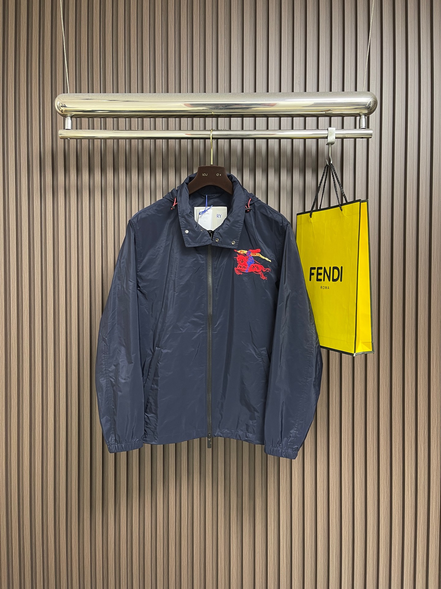 NO:759437,Burberry  War Horse Embroidered Hooded Jacket, the outer layer and inner lining are made of polyamide fabric. The plain high-density weaving process gives the fabric light and crisp characteristics. The weight is only 120g per square meter, making it easy to wear. The high-density weaving of the fabric makes it waterproof to a certain extent and prevents water droplets.  It condenses and slides off quickly after being touched. The lining is made of polyamide plain cloth of the same color, which is smooth to the touch, reducing friction with the inner clothing and improving wearing comfort. The embroidery is composed of 'multi-color layered embroidery + towel embroidery', using red nylon thread to flatly embroider the dynamic outlines of knights and horses, with a stitch density of up to  8 stitches per centimeter ensure smooth lines and capture the tension of the galloping horse. The horse body and the knight's clothing are filled with red and blue terry embroidery. The stacking of yarns creates a full texture, simulating the real touch of fur and fabric. The knight's cloak is integrated with golden metallic yarn.  The chain embroidery presents an elegant and dynamic look, which contrasts sharply with the dark blue fabric and enhances the visual impact. The overall wiring is straight and delicate, the fabric is comfortable and soft, and the color is consistent without color difference. It can be matched with the same style to create a fashionable look, and can be used in various occasions. Customized accessories, complete with three standards, the same style for men and women!  Sizes S-XL,,burberry,jackets & coats,jackets & coats,hats,19860909Burberry 战马绣花连帽夹克外套,外层与内衬均采用聚酰胺面料,通过平纹高密度织造工艺,赋予面料轻薄挺括的特性,每平方米重量仅120g,穿着无负担.面料的高密度编织使其具有一定的防水性,水滴接触后可迅速凝结滑落.内衬采用同色系聚酰胺平布,触感光滑,减少与内搭衣物的摩擦,提升穿着舒适度.刺绣采用'多色分层绣＋毛巾绣'复合,以红色锦纶线平绣骑士与骏马的动态轮廓,针脚密度达每厘米8针,确保线条流畅,捕捉马匹奔腾的张力.马身与骑士服饰部分采用红色与蓝色毛巾绣填充,通过纱线的堆叠形成饱满的肌理感,模拟皮毛与织物的真实触感.骑士披风处融入金色金属感纱线,以链式绣呈现飘逸动态,与深蓝色面料形成鲜明对比,增强视觉冲击力.整体走线平直细腻,面料舒适柔软,颜色一致无色差能与同款搭配营造时尚造型,驾驭各种场合,定制辅料,三标齐全,男女同款！尺码S-XL,,burberry,jackets & coats,jackets & coats,hats,,Men's clothing