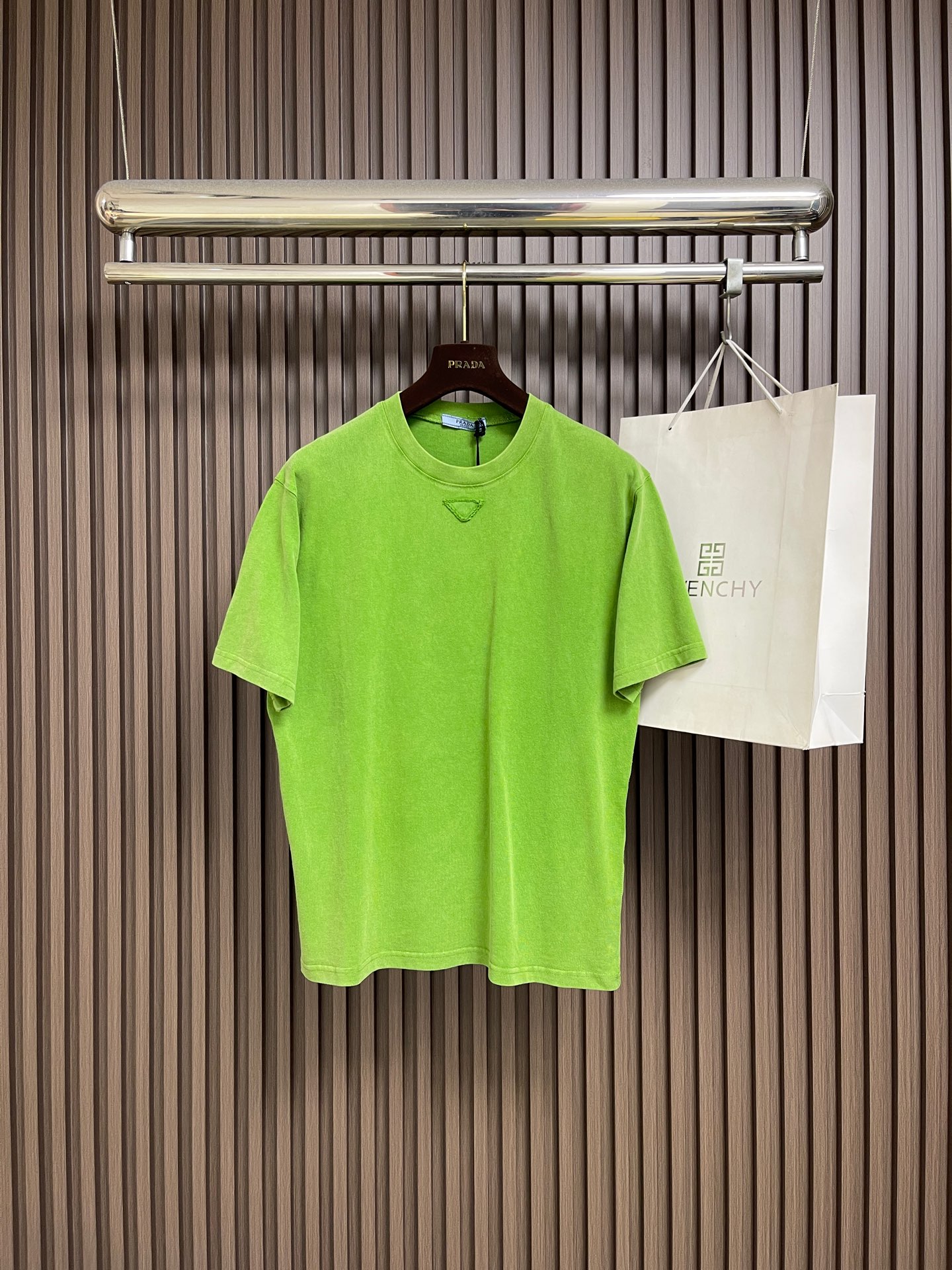 NO:773729,Prada  Triangle logo round neck short-sleeved T-shirt, pure cotton plain fabric, made of 12-count fine cotton jersey fabric, weight 230gm2; with 32-count double yarn high rib, weight 350gm2. The 12-count yarn is relatively thick, giving it a smooth surface  The material has a rustic texture, solid thickness and excellent durability. The combing process makes the cotton fibers neatly arranged, removes short fibers and impurities, and ensures the fabric's softness, skin-friendliness and surface finish. The weight of the fabric is medium to heavy, ensuring that  The T-shirt has good stiffness, drape and wrinkle resistance, and is not easy to collapse and deform. Double yarn high-weight ribs are used on the neckline to provide solid collar support for the roving base, ensuring that the collar shape remains stiff after being worn and washed many times. A conceptual triangle logo is sewn to the  Pre-cut fabrics of the same color but with different textures are cut into precise triangles. Through high-density seam embroidery processing, this triangular patch is accurately sewn to the body. The stitching method must not only firmly fix the patch, but also form a delicate  Decorative outline. On a minimalist solid color base, a pure geometric figure and subtle material and texture contrast are used to create a striking visual focus and architectural sense. Washing and fading is a unique technology that simulates the natural old feel through controlled stone grinding, enzyme washing and other processes. The original dye in the cotton fiber is partially removed, forming uneven fading traces on the dark base, thereby creating a soft, retro grayscale visual effect. Giving the fabric a unique nostalgic charm and softness  and layering, while also significantly improving the feel of the fabric and avoiding the stiffness of new fabrics. The round neck, square, dropped shoulders and short sleeves have a box-shaped silhouette, straight shoulder lines, and similar bust and waist widths. This kind of tailoring creates a neat, retro and slightly  The loose silhouette with an oversized feel complements the tough geometric shape of the triangle. The straight bottom edge further strengthens this neat feeling. The hem is not curved and remains horizontal and straight, highlighting the architectural aesthetics. Sizes S-XL  Size S, bust 110, shoulder width 50, length 71, size M, bust 114, width 52, length 72, size L, size bust 118, width 54, length 73, size XL, size chest 122, width 56, length 74, prada, versace, T-shirt, tees, t-shirt,19860909Prada 三角徽标圆领短袖T恤,纯棉质平纹面料,采用12支精棉平纹针织面料,克重为230gm2;搭配32支双纱高罗纹,克重为350gm2.12支纱线相对较粗,赋予面料质朴的肌理感、扎实的厚度和优异的耐用性.精梳工艺使棉纤维排列整齐,去除了短纤维和杂质,确保了面料的柔软亲肤性和表面光洁度.面料克重属于中等偏重磅,确保了T恤良好的挺括感、垂坠性和抗皱性,不易软塌变形.双纱高克重罗纹用于领口,为粗纱基底提供坚实的领部支撑,确保多次穿洗后领型仍保持挺括.缝制概念三角形徽标,将预先裁剪好的同色系,但具有质感差异的面料切割成精确的三角形.通过高密度锁边绣工艺处理,将这块三角形贴片精准缝制于衣身.其针法既要牢固固定贴片,又形成精致的装饰轮廓.在极简的纯色基底上,通过一个纯粹的几何图形和微妙的材质与肌理对比,创造出引人注目的视觉焦点和建筑感.洗水褪色做旧处理,通过控制性的石磨、酶洗等工艺,模拟自然旧化感的独特技术.部分去除棉纤维中的原身染料,在深色基底上形成不均匀的褪色痕迹,从而营造出柔和、复古的灰度视觉效果.赋予织物独特的怀旧韵味与柔和层次感,同时更能显著改善面料手感,避免了新面料的生硬感.圆领方正落肩短袖版型,衣身呈箱型轮廓,肩线平直,胸围和腰围宽度相近.这种剪裁营造出利落、复古且略带oversized感的宽松轮廓,与三角形的硬朗几何造型相得益彰.平直底边进一步强化了这种利落感,下摆不做弧度处理,保持水平直线,凸显建筑美学.尺码S-XL S码 胸围110肩宽50衣长71 M码胸围114肩宽52 衣长72 L码 胸围118肩宽54 衣长73 XL码胸围122肩宽56 衣长74,,prada,versace,T-shirt,tees，t-shirt,,Men's clothing