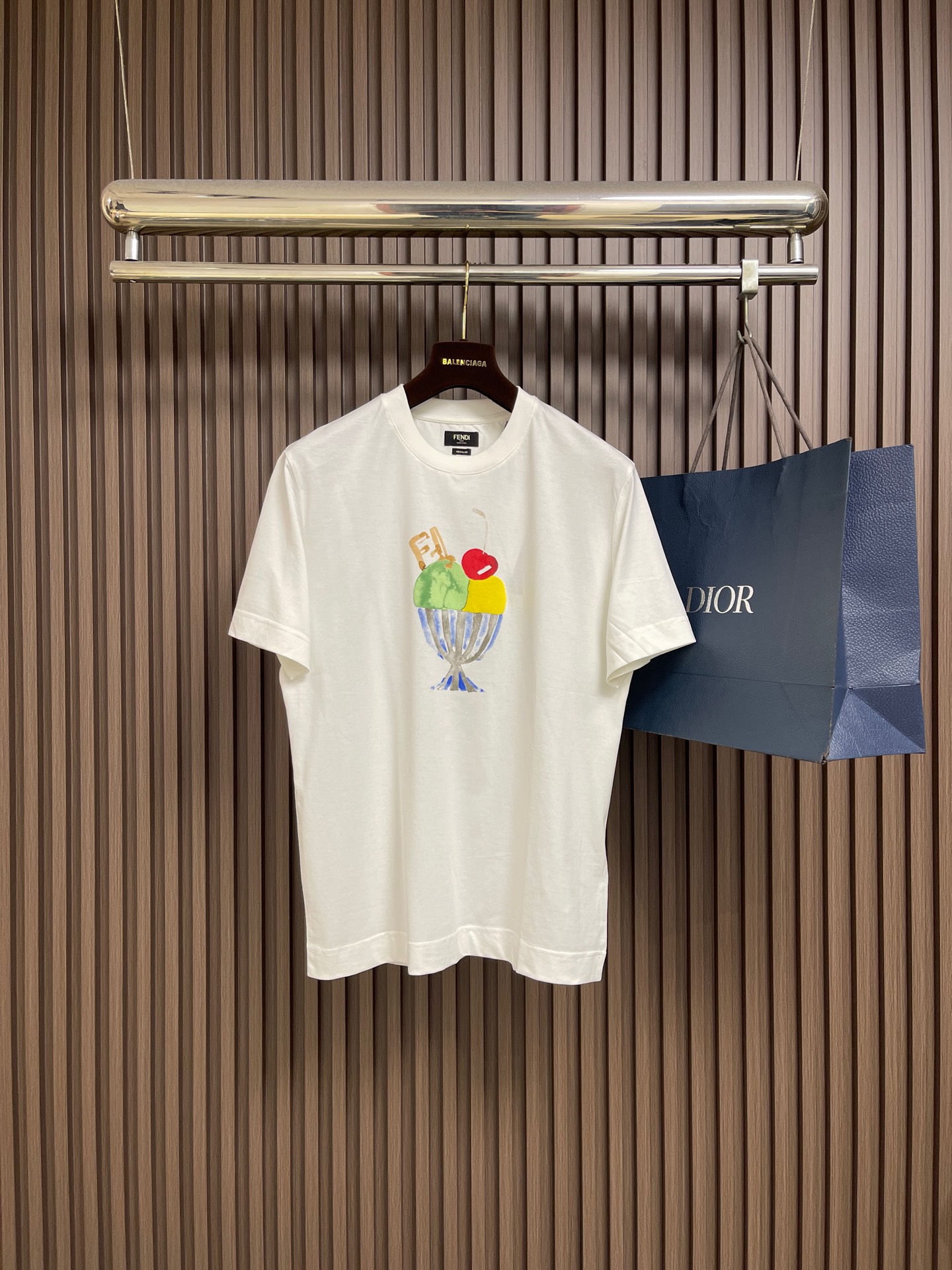 NO:773709,FENDI  Ice cream sundae printed short-sleeved T-shirt, made of imported high-count combed double-ply cotton fabric, with fine texture and skin-friendly texture, soft and breathable, with excellent drape and anti-wrinkle properties. The upper body is comfortable and not sweaty, and will not deform easily after long-term wear. It is perfectly suitable for daily commuting, leisure travel and other scenarios; classic round neck design, double-layer rib reinforcement technology is used on the neckline, which fits the neck without tightening and can be worn for a long time.  It is not easy to baggage, and its simple and elegant style is suitable for various styles. The front of the garment uses high-precision digital direct-injection printing technology to present a fun sundae pattern. The colors are full and bright, and the brushstrokes are flexible and natural. The details of the ice cream ball, cherry and cup body are lifelike, which not only adds an artistic sense and visual layer to the simple garment, but also highlights the brand's creative design concept. Size XS-L  XS size bust 102 shoulder width 44.5 length 70 size S chest size 106 shoulder width 46 length 72 size M chest size 110 shoulder width 47.5 length 74 L size chest size 114 shoulder width 49 length 76, fendi, T-shirt, tees, t-shirt,19860909FENDI 圣代冰淇淋印花短袖T恤,采用进口高支精梳双股棉面料,质地细腻亲肤,触感柔软透气,兼具出色的垂坠感与抗皱性,上身舒适不闷汗,久穿不易变形,完美适配日常通勤、休闲出行等多种场景；经典圆领设计,领口做双层罗纹加固工艺,贴合颈部不勒肉,久穿不易松垮,简约大气适配各种穿搭风格；衣身正面采用高精密数码直喷印花工艺,呈现趣味圣代冰淇淋图案,色彩饱满鲜亮,笔触灵动自然,冰淇淋球、樱桃与杯身细节栩栩如生,既为简约衣身增添了艺术感与视觉层次,又彰显了品牌的创意设计理念.尺码XS-L XS码胸围102肩宽44.5衣长70 S码 胸围106肩宽46 衣长72 M码胸围110 肩宽47.5衣长74 L码 胸围114 肩宽49 衣长76,,fendi,T-shirt,tees，t-shirt,,Men's clothing