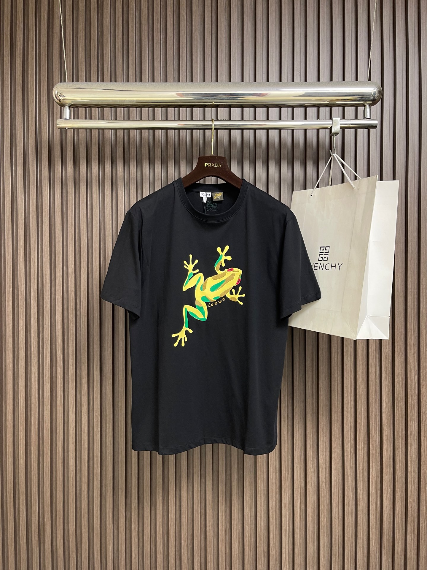NO:827432,Loewe The frog printed round neck short-sleeved T-shirt is made of 24-count special-spun compact cotton, 185gm2; with 32-count 1x1 rib, 340gm2. It is a medium-thick knitted fabric that is both stiff and comfortable. In the finishing stage before embroidery, the fabric is tentered and shaped by a high-temperature setting machine, and the warp and weft yarns are restored through tension control. The fabric is straight and has the same width, eliminating wrinkles and internal stress caused by the previous process. The compact spinning technology itself has made the fibers arranged parallel, hairiness significantly reduced, and the surface smooth and clean; the shaped fabric has both stiffness and softness, with a moderate drape. The frog pattern on the front is printed with environmentally friendly elastic glue, and then positioned A composite process for embellishment with needle embroidery. The combination of the two processes makes the pattern have the full color blocks of glue printing and the three-dimensional texture of embroidery. The background color of the frog is printed on the surface of the fabric through environmentally friendly elastic glue. The glue has excellent elasticity and adhesion, can extend synchronously with the stretching of the fabric, and is not easy to crack and fall off. At the same time Comply with environmental protection standards. The frog's eyes, patterns and other details are embellished and embroidered using positioning needle embroidery technology. The needle embroidery is a stitching method in which short stitches are closely arranged. The stitches are flat and the edges are sharp, which can accurately present the exquisite details of the frog pattern. The overall wiring is straight and delicate, the fabric is comfortable and soft, and the colors are consistent without color difference. It can be matched with the same style to create a fashionable look, and can be used in various occasions. Customized accessories, complete with three standards, same style for men and women! Sizes XS-L19860909Loewe 青蛙印绣圆领短袖T恤,采用24支特纺紧密棉,185gm2；搭配32支1x1罗纹,340gm2.属于兼具挺括与舒适的中厚型针织面料.在刺绣前的整理阶段,面料经高温定型机进行拉幅定形,通过张力控制使经纬纱恢复平直、门幅一致,消除前道工序产生的褶皱与内应力.紧密纺技术本身已使纤维排列平行、毛羽显著减少,表面光洁平滑；定形后的面料兼具挺括性与柔软度,垂坠感适中.正面青蛙图案采用环保弹力胶浆印花打底后,再以定位挨针刺绣进行点缀的复合工艺.两种工艺结合,使图案既有胶浆印花的饱满色块,又有刺绣的立体质感.青蛙的底色通过环保弹力胶浆印于面料表面,该胶浆具有优异的弹性与附着力,能随面料拉伸而同步延展,不易开裂脱落,同时符合环保标准.采用定位挨针刺绣工艺对青蛙的眼睛、花纹等细节进行点缀刺绣.挨针刺绣是一种短针脚紧密排列的针法,针迹平整、边缘锐利,能精准呈现青蛙图案的精致细节.整体走线平直细腻,面料舒适柔软,颜色一致无色差 能与同款搭配营造时尚造型,驾驭各种场合,定制辅料,三标齐全,男女同款！尺码XS-L XS码胸围104肩宽47 衣长71 S码 胸围108肩宽48.5 衣长73 M码胸围112 肩宽50 衣长75 L码 胸围116 肩宽51.5衣长77,,loewe,T-shirt,tees，t-shirt,,Men's clothing