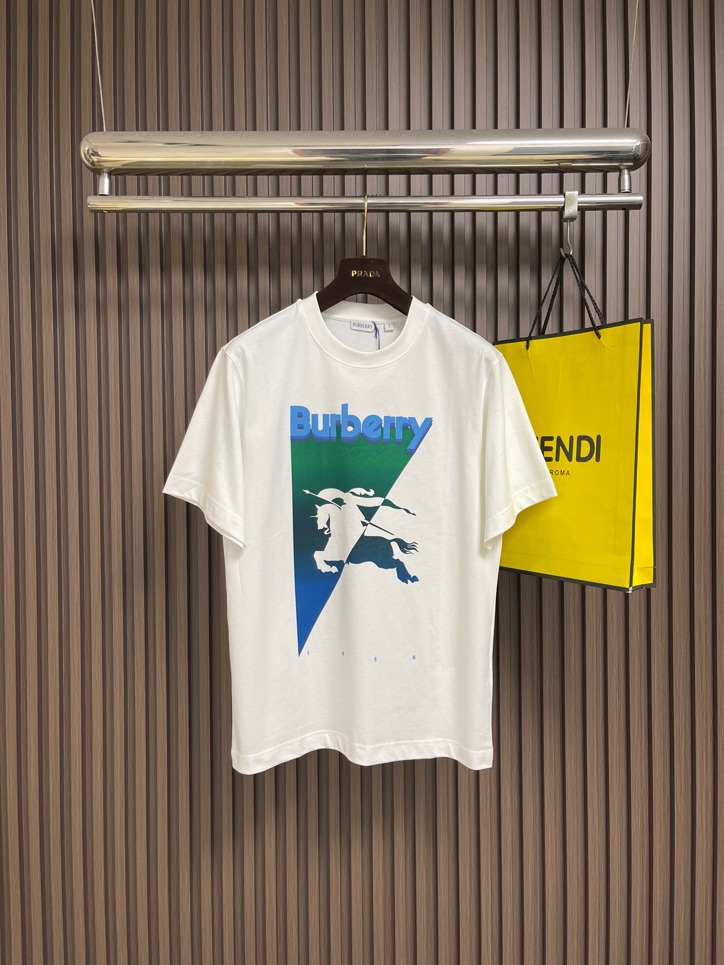 NO:839864,Burberry  Gradient inverted triangle round neck short-sleeved T-shirt, made of 15-count special-spun compact cotton, 230g㎡; paired with 32-count 1×1 rib, 340g㎡. The fabric is a heavy-gauge fabric with strong texture and crisp texture. Because the 15-count yarn is thicker, the shaping process is particularly important.  It can eliminate the internal stress generated during the weaving process of thick yarns and prevent pattern misalignment due to fabric shrinkage during subsequent multi-layer printing. The collar is a high-density tight rib made of cotton. The cotton rib is elastic through high-density weaving and has a more pure and natural touch. The two-color equestrian knight logo and  The brand logo adopts three superposition processes of penetration printing + thick plate printing + suede printing, so that the logo has the delicate gradient of penetration printing, the three-dimensional outline of thick plate printing, and the rich tactile layers of suede printing. As the bottom layer, the water-based slurry penetrates into the fiber to form a pattern.  The basic contours and color levels of the pattern present a watercolor-like blooming effect, with a soft and glue-free feel. Stacked printing in specific areas creates a raised three-dimensional relief feeling. Through repeated printing many times, the slurry is accumulated to the point. The overall wiring is straight and delicate, the fabric is comfortable and soft, and the colors are consistent and without color difference.  It can be matched with the same style to create a fashionable look, and can be used in various occasions. Customized accessories, complete with three standards, same style for men and women!  Size XS-L19860909Burberry 渐变倒三角圆领短袖T恤,用15支特纺紧密棉,230g㎡；搭配32支1×1罗纹,340g㎡.面料属于粗针重克重面料,肌理感强、质地挺括.由于15支纱线较粗,定形工序尤为重要,它能消除粗支纱线织造过程中产生的内应力,防止后续多层印花时因面料收缩导致图案错位.衣领属于全棉高密度紧实罗纹,全棉罗纹通过高密度织造实现弹性,触感更加纯粹自然.双色马术骑士徽标和品牌徽标采用渗透印花+厚板印花+绒面印花三种工艺叠加,使徽标既有渗透印花的细腻渐变,又有厚板印花的立体轮廓,还有绒面印花的丰富触觉层次.作为底层水性浆料渗透至纤维内部,形成图案的基础轮廓与色彩层次,呈现类似水彩的晕染效果,且手感柔软无胶感在特定区域堆叠印出凸起的立体浮雕感,通过多次重复印刷使浆料堆积至.整体走线平直细腻,面料舒适柔软,颜色一致无色差 能与同款搭配营造时尚造型,驾驭各种场合,定制辅料,三标齐全,男女同款！尺码XS-L XS码胸围102肩宽46.5衣长71 S码 胸围106肩宽48衣长73 M码胸围110 肩宽49.5衣长75 L码 胸围114 肩宽51衣长77,,burberry,T-shirt,tees，t-shirt,,Men's clothing