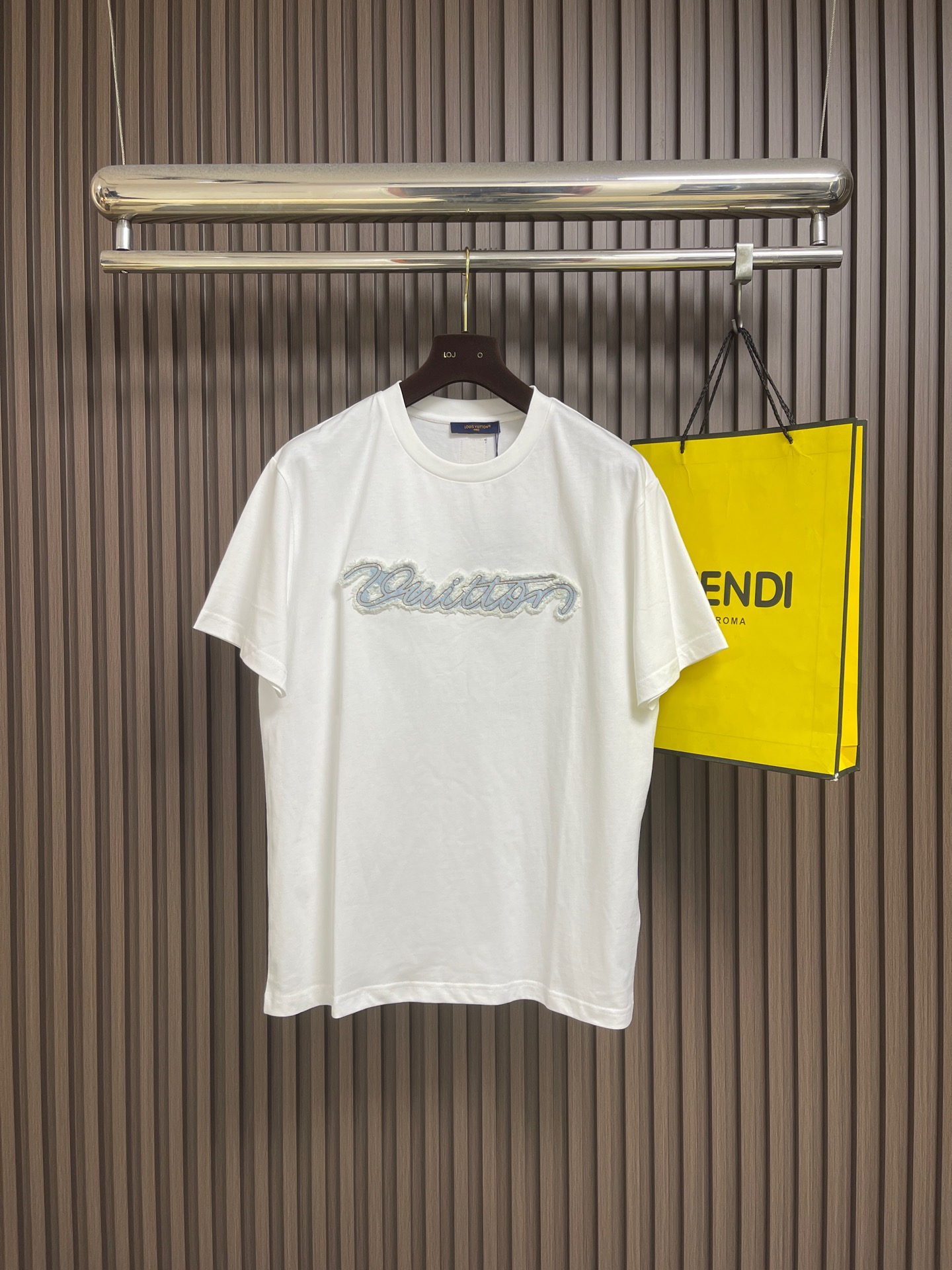 NO:848725,LV Denim appliqué embroidered round neck short-sleeved T-shirt, made of 15-count special-spun compact cotton with a weight of 230g㎡; paired with 32-count 1×1 rib; a weight of 340g㎡. The fabric is a medium-thick knitted fabric, the 15-count yarn is thicker, the fabric has a strong texture and a crisp texture. The cotton fiber cross-section of the fabric is round, Significantly enhances the gloss and smoothness. Mercerizing can improve the adsorption uniformity of dyes and make the fabric background color fuller and more uniform. It is then stretched and set by a high-temperature setting machine, and the warp and weft yarns are restored to straightness through tension control, eliminating wrinkles and internal stress. The 32-count rib neckline retracts to its optimal elastic state, and the ribbing The tight structure is fully stabilized during this process, forming a snug fit without being stretched. The patch itself is a piece of denim fabric. The pattern is precisely laser cut according to the outline of the handwriting to form a letter-shaped patch. It undergoes independent washing and distressing before sewing. Pumice and low-concentration bleach are added. Through mechanical friction and chemical action, the surface of the denim will produce irregular color fading, whitening and slight yarn breakage. This treatment simulates the natural fading and wear effects of denim after years of wearing, giving the patch a texture. The overall wiring is straight and delicate, the fabric is comfortable and soft, and the color is consistent without color difference. It can be matched with the same style to create a fashionable look, and can be used in various occasions. Customized accessories, complete with three standards, same style for men and women! Sizes XS-L19860909LV 牛仔贴布绣圆领短袖T恤,采用15支特纺紧密棉,克重为230g㎡；搭配32支1×1罗纹；克重为340g㎡.面料属于中厚型针织面料,15支纱线较粗,织物肌理感强,质地挺括.面料棉纤维截面圆润,显著增强光泽度与平滑感,丝光能提升染料的吸附均匀性,使面料底色更加饱满匀净.后经高温定型机拉幅定形,通过张力控制使经纬纱恢复平直,消除褶皱与内应力.32支罗纹的领口回缩至最佳弹性状态,罗纹的紧实结构在此过程中充分稳定,形成贴合而不勒的贴饰本身是一块牛仔布料,对版按照手写体轮廓进行精密的激光切割裁切,形成字母形态的贴饰.缝制前先经历了独立的洗水做旧处理.加入浮石和低浓度漂白剂,通过机械摩擦和化学作用,使牛仔布表面产生不规则的色落、磨白和轻微的纱线断裂.这种处理模拟了牛仔布经年穿着后的自然褪色和磨损效果,赋予贴饰纹理感.整体走线平直细腻,面料舒适柔软,颜色一致无色差 能与同款搭配营造时尚造型,驾驭各种场合,定制辅料,三标齐全,男女同款！尺码XS-L XS码胸围110肩宽49 衣长70 S码 胸围114肩宽50.5衣长72 M码胸围118肩宽52衣长74 L码 胸围122肩宽53.5衣长76,,louis vuitton,T-shirt,tees，t-shirt,,Men's clothing