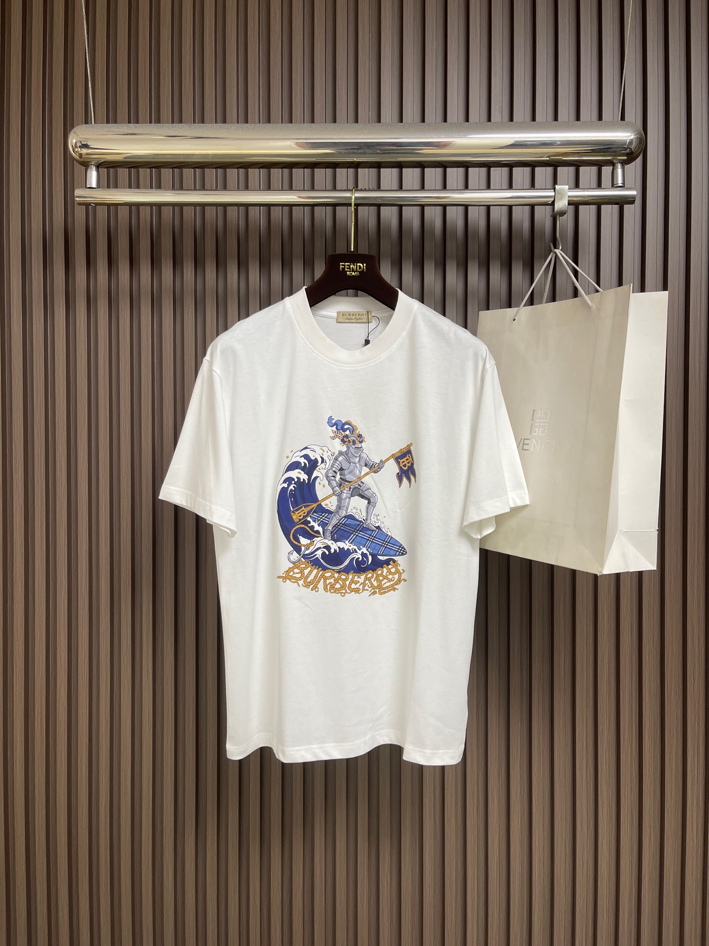 NO:847367,Burberry The knight printed round neck short-sleeved T-shirt is made of 15-count special compact cotton plain knit fabric with a weight of 230g㎡; 32-count high-weight 1x1 rib with a weight of 340g㎡. The 15-count yarn is thicker, the fabric has a strong texture and a crisp texture. In the finishing stage before printing, mercerization is a key process. The fabric significantly enhances the gloss and Smooth feeling; at the same time, mercerization can improve the uniformity of dye adsorption and make the fabric background color fuller and more uniform. The neckline uses 32 high-weight 1x1 ribs. The woven structure makes the rib tissue denser and has excellent elastic recovery rate, which can effectively prevent the neckline from loosening and deforming after repeated wearing and taking off. The hand-painted artistic pattern uses dot paste printing + suede foam printing process Combining art with art to achieve a rich visual effect. First, dot paste printing uses a fine screen to overprint the color paste in the form of dots to form a gradient and breathable translucent effect, which is used to express the texture and light and shadow levels of the plaid lounge chair. Suede foam printing prints foamed paste on specific areas of the pattern, and the foamed microspheres in the paste expand when baked at high temperature. It forms a three-dimensional raised and soft-touch suede texture. The combination of the two processes not only ensures the clarity and color saturation of the pattern details, but also vividly reproduces the lazy atmosphere of the leisurely scene through the concave and convex touch of the foam printing, forming a rigid and soft contrast with the stiffness of the medium-thick fabric. The overall wiring is straight and delicate, the fabric is comfortable and soft, and the colors are consistent without color difference. It can be matched with the same style to create a fashionable look, and can be used in various occasions. Customized accessories, complete with three standards, same style for men and women! Sizes XS-L19860909Burberry 骑士印花圆领短袖T恤,采用15支特纺紧密棉平纹针织面料,克重为230g㎡；32支高克重1x1罗纹,克重为340g㎡.15支纱线较粗,织物肌理感强,质地挺括.在印花前的整理阶段,丝光处理是关键工序.面料显著增强光泽度与平滑感；同时,丝光能提升染料吸附均匀性,使面料底色更加饱满匀净.领口采用32支高克重1x1罗纹,编织结构使罗纹组织更加致密,弹性恢复率优异,能有效防止领口在反复穿脱后松垮变形.手绘艺术图案采用网点浆印花+绒面发泡印花工艺结合,实现层次丰富的视觉效果.首先,网点浆印花通过细密网版将色浆以网点形式叠印,形成渐变、透气的半透明效果,用于表现格纹躺椅的纹理与光影层次.绒面发泡印花将发泡浆料印于图案特定区域,经高温烘烤时浆料中的发泡微球膨胀,形成立体隆起、触感柔软的绒面质感.两种工艺结合,既保证了图案细节的清晰度与色彩饱和度,又通过发泡印花的凹凸触感,生动再现了悠闲景致的慵懒氛围,与中厚面料的挺括形成刚柔对比.整体走线平直细腻,面料舒适柔软,颜色一致无色差 能与同款搭配营造时尚造型,驾驭各种场合,定制辅料,三标齐全,男女同款！尺码XS-L XS码肩宽48 胸围104衣长70  S码肩宽50 胸围110衣长72  M码 肩宽52 胸围116衣长74 L码 肩宽54 胸围120衣长76,,burberry,T-shirt,tees，t-shirt,,Men's clothing