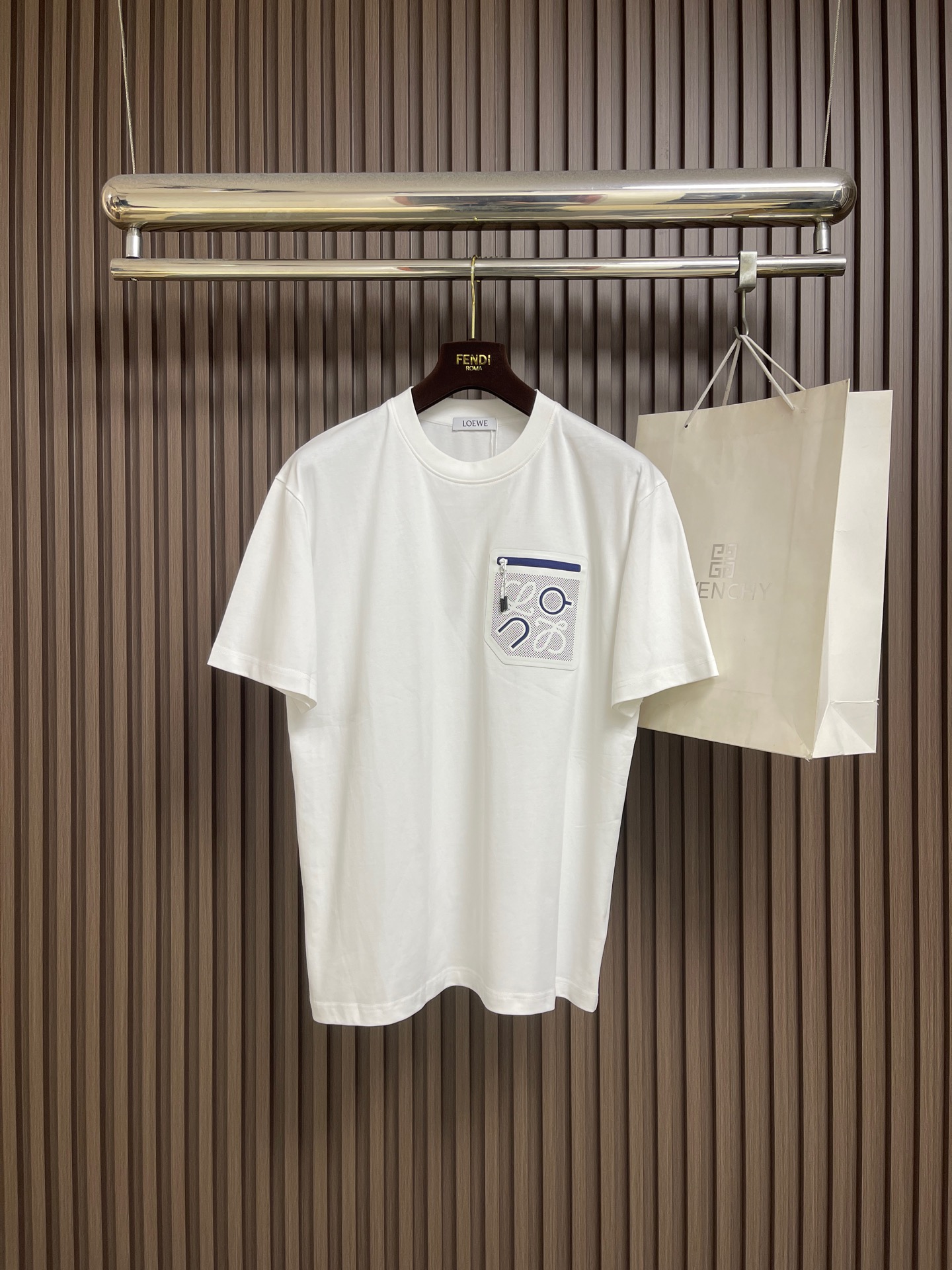 NO:847394,Loewe x  on's co-branded laminated pocket logo short-sleeved T-shirt is made of high-count and high-density plain cotton, which is soft and breathable to the touch and has a neat silhouette. The iconic pocket on the chest uses precision laser hollowing technology to accurately cut out the brand's Anagram totem.  The edge is smooth and burr-free, giving it a full three-dimensional feel; paired with a contrasting web zipper, the contrasting colors of blue, white, orange and black break the monotony, and the neat lines collide to create a sense of vitality and high-end. It integrates the brand's iconic details with functional design, showing ingenuity in a low-key manner. Size XS-L  XS size shoulder width 48, chest size 104, length 70, size S, size shoulder width 50, chest size 110, length 72, size M, size shoulder width 52, size chest 116, length 74, size L, size shoulder width 54, chest size 120, length 76,,loewe,T-shirt,tees,t-shirt,19860909Loewe x on昂跑联名压胶口袋logo短袖T恤,甄选高支高密平纹棉料,触感软糯透气,自带利落廓形.胸前标志性口袋采用精密激光镂空工艺,精准切割出品牌Anagram图腾,边缘光滑无毛刺,立体感十足；搭配撞色织带拉链,蓝白橘黑撞色打破单调,利落线条碰撞出活力与高级感,将品牌标志性细节与功能性设计融为一体,低调中尽显巧思.尺码XS-L XS码肩宽48 胸围104衣长70  S码肩宽50 胸围110衣长72  M码 肩宽52 胸围116衣长74 L码 肩宽54 胸围120衣长76,,loewe,T-shirt,tees，t-shirt,,Men's clothing