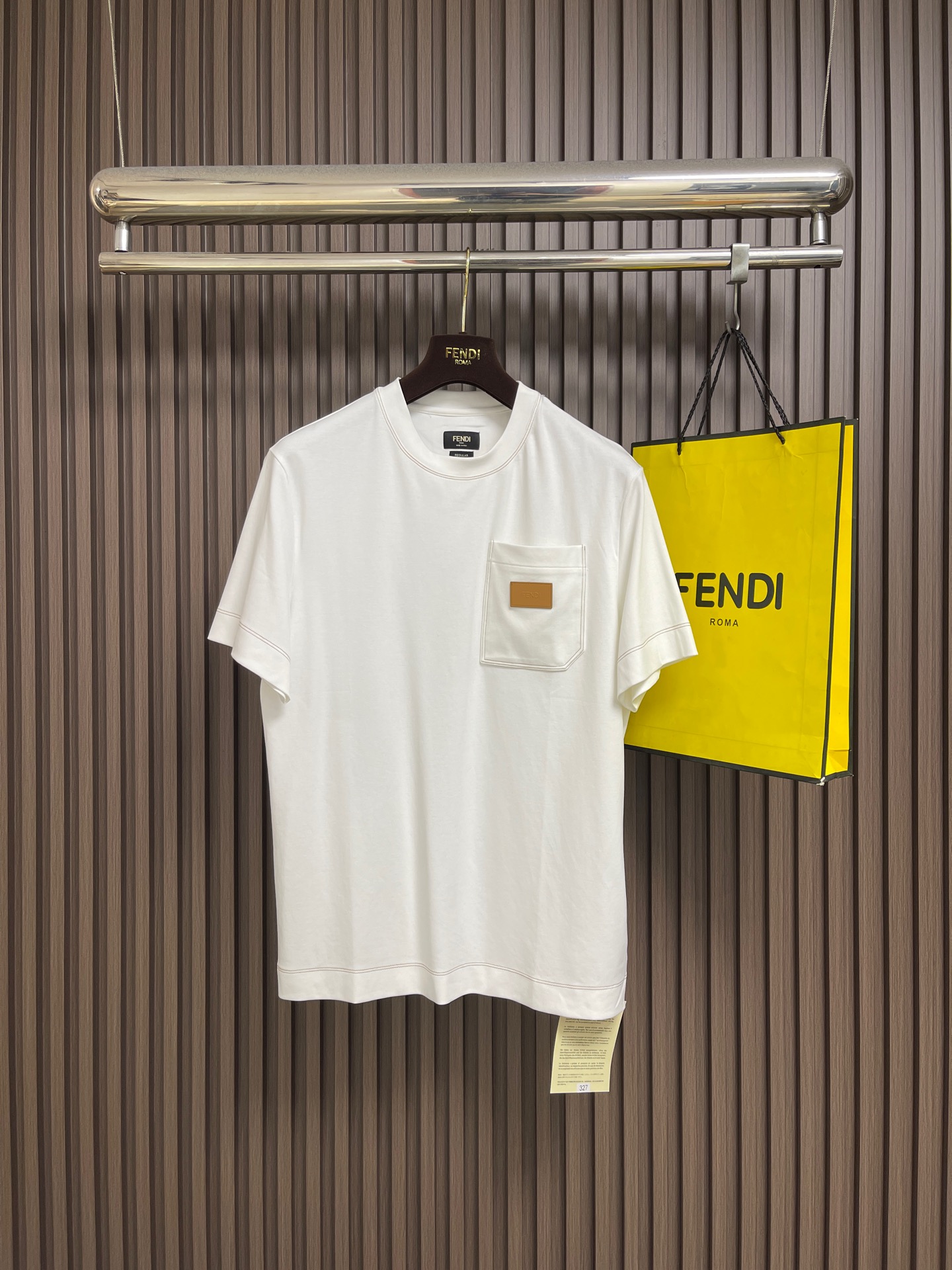 NO:875285,Fendi  Short-sleeved T-shirt with leather patch. The fabric is made of high-count combed long-staple cotton. The fiber is fine and compact, and the cloth surface is smooth and smooth. The cotton fiber has excellent breathability, good moisture absorption and perspiration, and the upper body is soft and skin-friendly, not stuffy or sticky. After the fabric is pre-shrunk, sanded and anti-wrinkle shaping process, it drape and stiffness is not easy to collapse, and it is not easy to deform or pill after being washed for a long time.  , does not fade, and highlights the solid texture. The details are sewn with vintage brown and yellow contrasting topstitching, and the double-needle chain sewing process is used throughout. The collar, cuffs, hem, breast pockets, and back collar are all evenly routed. The contrasting color thread and the white background form a natural transitional visual hierarchy. The stitch spacing is even and regular, and the double lines are parallel and straight and smooth, which not only strengthens the structural shape,  The firmness of the garment body is reinforced to prevent cracking, and extremely simple lines are used to outline a high-end texture. The chest patch pocket is three-dimensionally cut, and the bag mouth is shaped by high temperature. The bag body is flat and compliant, and the edges of the bag are double-needle overlock seamed, which is strong and wear-resistant. Customized leather is used for the details of the patch pocket. The leather is flexible and shiny, and the edges are polished and sealed, and the letters are engraved using high-temperature embossing technology.  The logo and font are clear and neat. The edges of the leather label are precision sewn and fixed to the bag body, and the lines are dense and neat. The back of the collar is sewn with square decorative stitches using special wood pulp fiber sutures. The wood pulp fiber threads are tough, not easy to break, and have a warm color. The square lines are neat and symmetrical, echoing the contrasting topstitching style throughout the body, and are both decorative and reinforcing. Sizes S-XL  Size S, shoulder width 46, bust 104, length 68, size M, shoulder width 47, bust 108, length 69.5, size L, shoulder width 48, bust 112, length 71, size XL, shoulder width 49, bust 116, length 72.5, fendi, T-shirt, tees, t-shirt,19860909Fendi 饰皮革贴片短袖T恤,面料甄选高支精梳长绒棉面料织造,纤维细腻紧实,布面平整顺滑.棉纤维自带优良的透气性,吸湿排汗性俱佳,上身柔软亲肤,不闷不粘.面料经过预缩、磨毛与抗皱定型工艺处理之后,垂坠挺括不易软塌,久洗不易变形、不起球、不褪色,凸显扎实的质感.细节采用复古棕黄撞色明线精工缝制,全程采用双针链式车缝工艺,领口、袖口、下摆、胸袋、后领无一例外均匀走线.撞色线与白底色形成自然过渡的视觉层次,针脚间距均匀规整,双线平行笔直流畅,不仅强化结构定型,加固衣身牢固度,不易崩线开裂,更用极简明线勾勒出高级质感.胸贴袋采用立体剪裁,袋口经过高温定型,袋身平整服帖,袋边双针包边锁缝,牢固耐磨；贴袋点缀的细节选用定制皮革,皮料柔韧有光泽,边缘经打磨封边,再采用高温压印工艺刻印字母标识,字体清晰工整.皮标边缘精密车缝固定于袋身,走线密实工整.衣领背部采用木浆纤维专用缝线缝制方形装饰线迹,木浆纤维线材韧性强、不易断裂、色泽温润,方形走线工整对称,与全身撞色明线风格呼应,兼具装饰性与加固作用.尺码S-XL  S码 肩宽46 胸围104 衣长68 M码肩宽47 胸围108 衣长69.5 L码 肩宽48 胸围112 衣长71 XL码 肩宽49 胸围116 衣长72.5,,fendi,T-shirt,tees，t-shirt,,Men's clothing