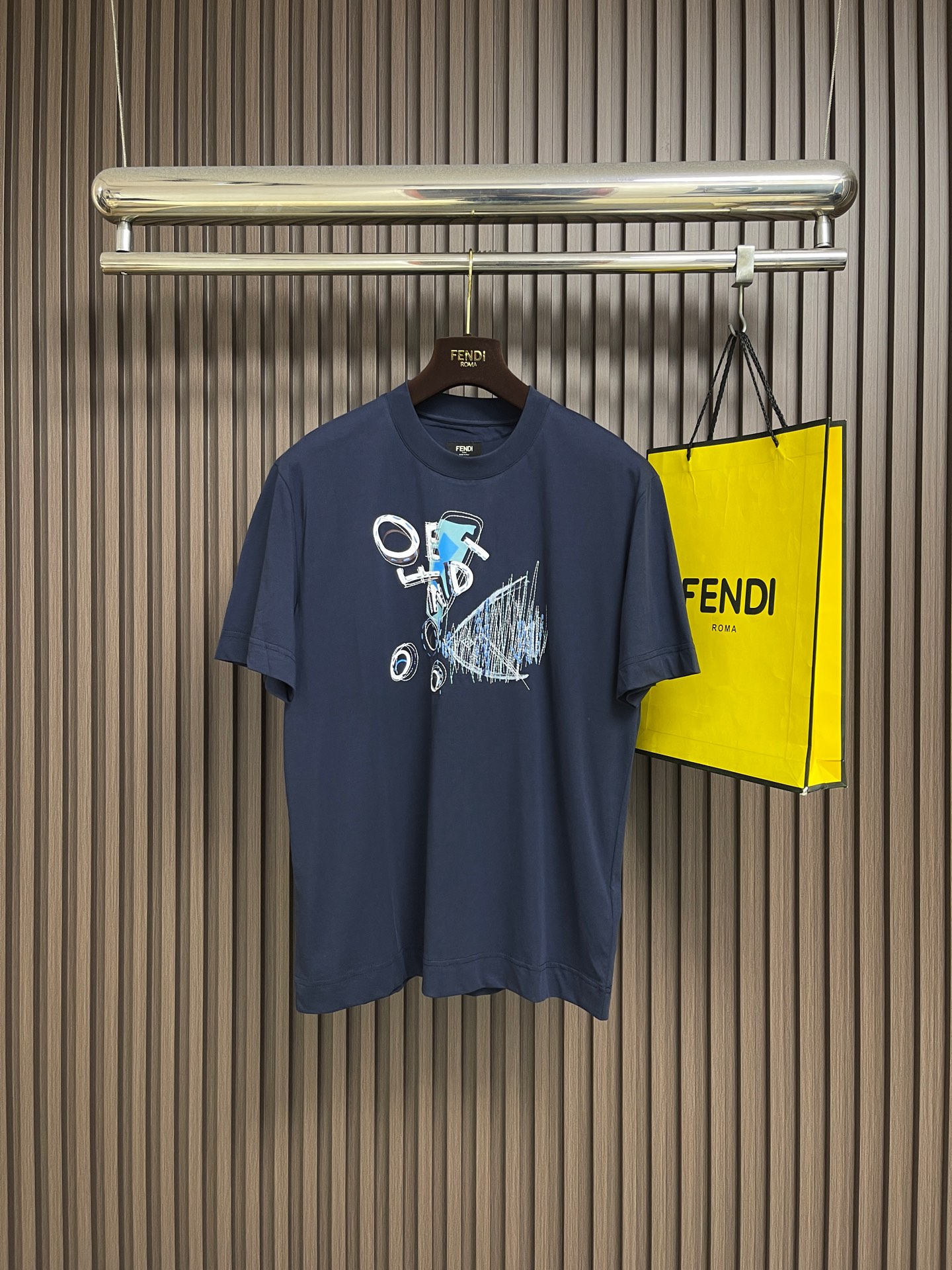 NO:856162,Fendi  The goldfish print embroidery round neck short-sleeved T-shirt is made of 24-count double-sided knitting, 250gm pure cotton fabric, with 24-count 1×1 rib, 200gm. The 24-count double-sided knitting is a medium-to-high fine yarn count, the yarn is thin, and the cloth surface is delicate and smooth. The double-sided knitting structure consists of two front loops nested in each other.  , with a front-facing appearance on both sides. The weight of the fabric is in the medium-thick range, which gives the fabric a soft and crisp feel. It has the unique fluffy feel of double-sided knitting without losing the drape support, and the upper body is not soft. High color fastness reactive dye dyeing ensures that the dark blue color remains full after multiple washings.  The goldfish pattern on the front achieves the coexistence of two-dimensional colors and three-dimensional textures through environmentally friendly elastic glue + dot printing and the precise cooperation of printed multi-color rice grain embroidery. The water-based polyurethane-based printing slurry forms a film with a very high elongation at break after curing, and can be stretched synchronously with the expansion of double-sided knitting.  It will not crack after repeated washing. Dot printing transfers the slurry to the fabric in the form of micron-level dots through a high-mesh screen plate, which can achieve photo-level grayscale gradient and half-tone effects, avoiding the common color block faults of glue printing. The overall wiring is straight and delicate, the fabric is comfortable and soft, and the color is consistent without color difference.  Can be matched with the same style to create a fashionable look, to suit various occasions, customized accessories, complete with three standards!  Size XS-L19860909Fendi 金鱼印绣圆领短袖t恤,选用了24支双面针织,250gm的纯棉面料,搭配24支1×1罗纹,200gm.24支双面针织属于中高细纱支,纱线较细,布面细腻光滑.双面针织结构由两个正面线圈相互嵌套,具有两面皆为正面的外观.面料克重属于中厚范围,赋予了面料柔软的挺括感；既有双面针织特有的蓬松手感,又不失垂坠支撑力,上身不软塌.高色牢度的反应性染料染色,确保深蓝色在多次洗涤后依然饱满.正面的金鱼图案通过环保弹力胶浆+网点印花与对印花多色米粒绣的精密配合,实现了平面色彩与立体肌理的共.水性聚氨酯基印花浆料,其固化后形成的薄膜断裂延伸率极高,能跟随双面针织的延展而同步拉伸,反复洗涤后不龟裂.网点印花通过高目数网版将浆料以微米级点阵形式转移到面料上,能够实现照片级的灰度渐变和半色调效果,避免了胶浆印花常见的色块断层.整体走线平直细腻,面料舒适柔软,颜色一致无色差 能与同款搭配营造时尚造型,驾驭各种场合,定制辅料,三标齐全！尺码XS-L XS码肩宽47 胸围104衣长69.5  S码肩宽48.5 胸围108衣长71.5  M码 肩宽50 胸围112衣长73.5 L码 肩宽51.5胸围116衣长75.5,,fendi,T-shirt,tees，t-shirt,,Men's clothing