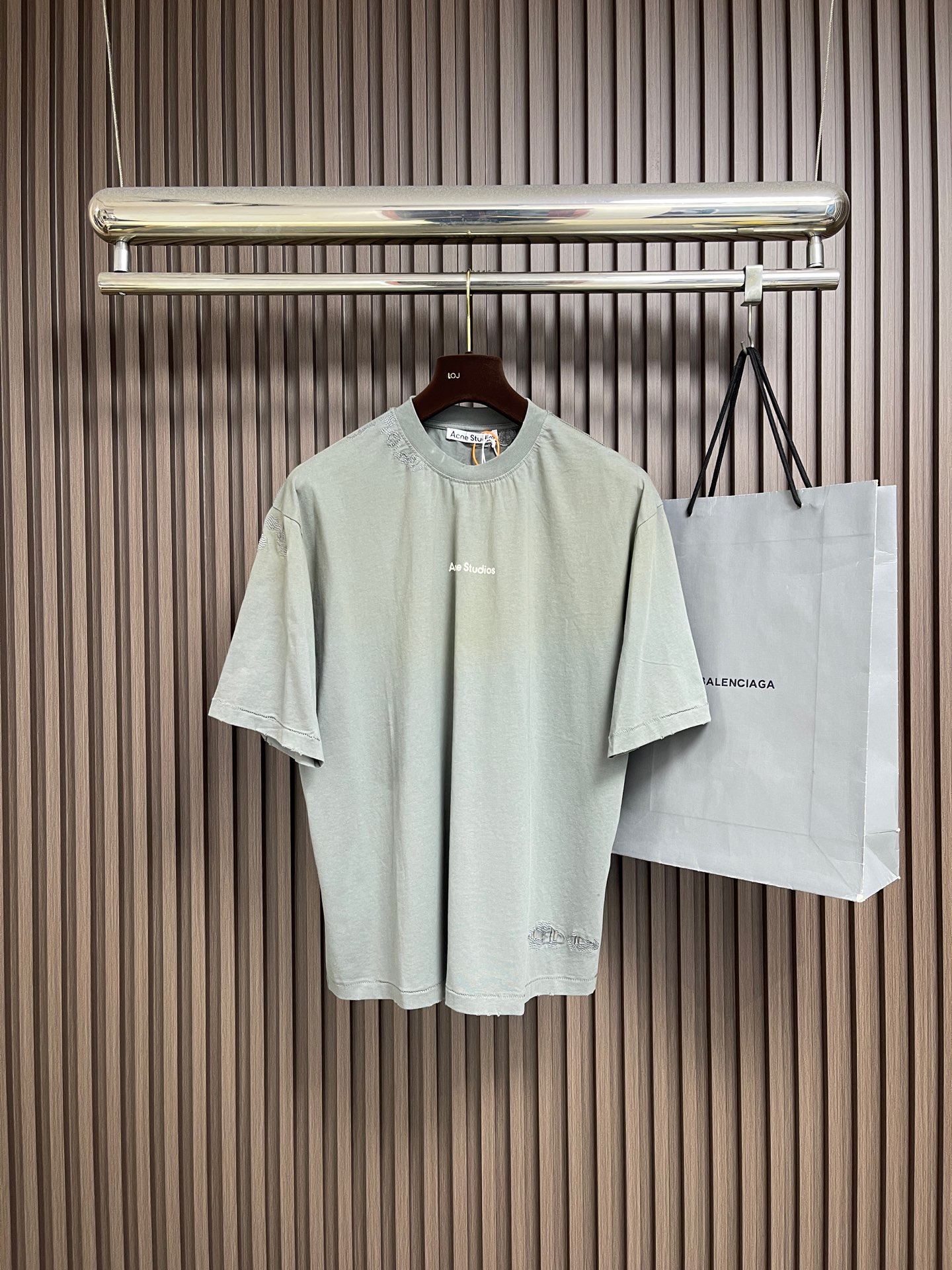 NO:911624,acne studios  Patch patch round neck short-sleeved T-shirt, coarse-grained pure cotton retro cotton fabric, using 12-count fine cotton plain fabric, with a weight of 230gm; paired with 32-count double yarn rib, with a weight of 350gm. The diameter of the 12-count yarn is thicker, and the natural hairiness on the surface is richer. The woven fabric will show a grainy and grainy texture visible to the naked eye.  Slightly undulating texture. Fine cotton means that cotton fibers have been combed to remove short velvet and impurities, ensuring that even with a thick count, the fabric is still pure, skin-friendly, and will not scratch people. The double-yarn rib provides strong structural support, and the high elasticity ensures that the round neck can fit the neck without being pinched. The rice grain repair effect is achieved through rice grain embroidery.  Mimicry technology. The rice grain embroidery process requires the embroiderer to arrange dense dots on the surface of the fabric with extremely short stitches. These stitches do not pursue smoothness, but deliberately form irregular, tiny protrusions, simulating the rough stitch marks on the edges of hand-stitched patches. The embroidery machine is controlled through computer programming to make the rice grain stitches appear  It seems to be random but is actually scattered in an orderly manner; the three-dimensional graininess is more delicate and the touch is richer. Paired with customized striped patch fabrics, the patches can be firmly attached to rough fabrics and will not be easily snagged like long stitches, which not only meets the aesthetic requirements, but also takes into account durability. The core feature of environmentally friendly glue printing is high covering power  And soft feel. Compared with penetration printing, glue covers the surface of the fabric to form a thin layer, the color is saturated and completely opaque, suitable for dark fabrics. The cracking problem is solved by adding high-elastic resin, so that the printing can stretch with the fabric, wear-resistant and washable, and has excellent artistic expression. Retro fading, washing, hole-making and old-fashioned technology, old and faded  Color treatment: Put the printed garments into an industrial washing machine and use a slight stone washing process. The surface of the fabric and the edges of the printed pattern will be unevenly stripped of color, resulting in natural fading and an old feeling of edge wear. The old and faded treatment makes the printed pattern show irregular mottled feelings, cracks and color differences. The center color remains darker,  The edge and raised parts become lighter in color, even revealing the fabric background and hole effect. It has a loose and neutral casual fit. This T-shirt is defined as a unisex style, casual fit, and hip length. Its style logic pursues a genderless wrapping feeling and extended proportions. The key point is that the length of the shirt is hip-length, which is not only to cover the buttocks, but also to  In order to make use of the elongated body and the drape of the fabric, it creates a lazy and flowing silhouette. In terms of process execution, the side seams need to maintain a straight hem to avoid the long body from looking like a straight bucket. Overall, it is a hybrid that combines the functional details of workwear with the relaxed feel of high fashion. Sizes S-M-L-XL  Size S, shoulder width 51, bust 110, length 68, size M, shoulder width 52.5, bust 114, length 70, size L, shoulder width 54, bust 118, length 72, size XL, shoulder width 55.5, bust 122, length 74,,acne studios,dior,T-shirt,tees,t-shirt,19860909acne studios 补丁贴布圆领短袖T恤,粗纹纺织纯棉复古棉面料,选用了12支精棉平纹面料,克重为230gm；搭配32支双纱罗纹,克重为350gm.12支纱线直径更粗,表面天然毛羽更丰富,织出的面料会呈现出一种肉眼可见的颗粒感与微起伏的肌理.精棉代表棉纤维经过精梳处理,剔除了短绒与杂质,确保了即使在粗支数下,面料依然纯净、亲肤,不会扎人.双纱罗纹提供了强有力的结构性支撑,高弹力确保了圆领能贴合颈部却不勒人.米粒修补效果通过米粒刺绣进行的拟态工艺.米粒刺绣工艺要求刺绣师以极短的针迹在面料表面进行密集的点状排列.这些针迹不追求平滑,而是刻意形成不规则的、微小的凸起,模拟出手工缝线补丁边缘粗糙的针脚痕迹.通过电脑编程控制刺绣机,使米粒针迹呈现出看似随意、实则有序的散布；立体颗粒感更细腻,触感更丰富.搭配定制的条纹补丁面料,能使补丁牢固地附着在粗犷的面料上,不会像长针迹那样容易被勾丝,既满足了美学要求,也兼顾了耐用性.环保胶浆印花的核心特点在于高遮盖力和柔软手感.相比渗透印花,胶浆覆盖在面料表面形成薄层,色彩饱和且完全不透底色,适用于深色面料.通过加入高弹树脂解决开裂问题,使印花能随面料拉伸,耐磨耐水洗,兼具艺术表现力优异.复古褪色洗水破洞做旧工艺,做旧褪色处理将印花后的成衣放入工业水洗机,采用轻微石洗工艺处理.面料表面和印花图案边缘会被不均匀地剥离颜色,形成自然落色、边缘磨损的陈旧感.做旧褪色处理使得印花图案呈现出不规则的斑驳感、裂纹和色差.中心颜色保留较深,边缘和凸起部位颜色变浅、甚至露出面料底色和破洞效果,宽松中性休闲版型,这款T恤定义为中性风格、休闲版型、衣长及臀；其版型逻辑追求的是无性别的包裹感与延长的比例.关键点在于衣长及臀,这不仅是为了遮住臀部,更是为了利用加长的衣身配合面料的垂坠感,营造出一种慵懒、流动的廓形.在工艺执行上,侧缝需要保持笔直的下摆,以避免长衣身显得像直筒水桶.整体来看,它是一个结合了工装功能细节与高级时装松弛感的混合体.尺码S-M-L-XL S码肩宽51 胸围110衣长68 M码 肩宽52.5 胸围114衣长70 L码肩宽54胸围118 衣长72 XL码 肩宽55.5 胸围122衣长74,,acne studios,dior,T-shirt,tees，t-shirt,,Men's clothing