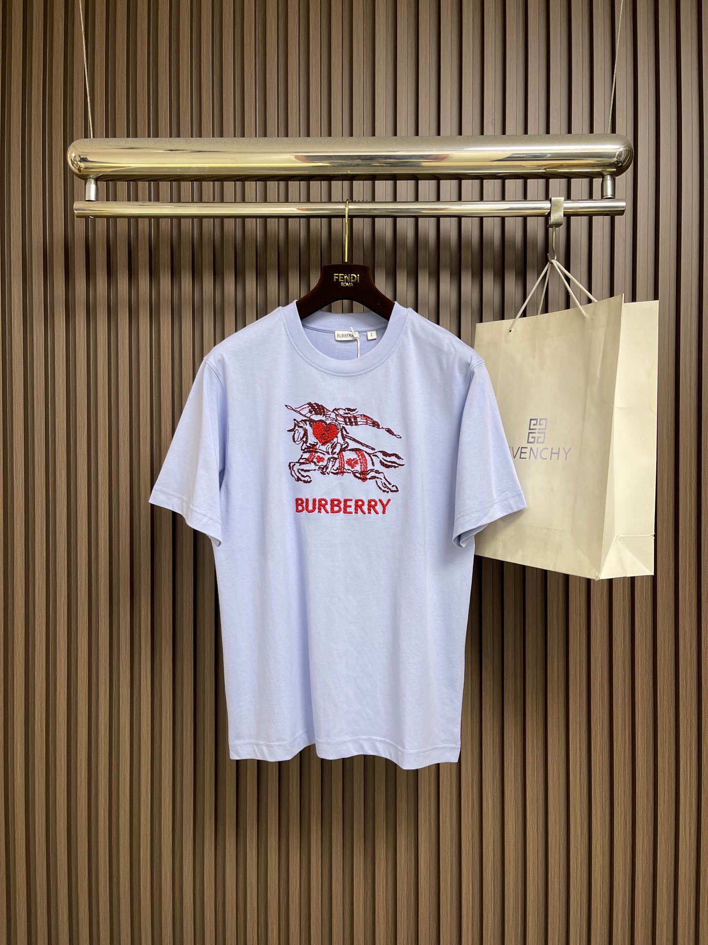 NO:914552,Burberry  The Love Shield War Horse round-neck short-sleeved T-shirt is made of 15-count special-spun compact cotton with a weight of 230g㎡. It is paired with 32-count high-weight 1x1 ribs for the neckline and has a weight of 349g㎡. The special-spun compact cotton uses compact spinning technology in the spinning process, which effectively reduces  The yarn hairiness is reduced, making the fabric structure denser, the surface smoother, and the pilling resistance better. The weight of the fabric is medium to heavy, ensuring that the T-shirt has good stiffness and drape, and is not easy to collapse and deform. Its high count and high weight characteristics ensure excellent elastic recovery of the collar.  Strength, thickness and resistance to deformation are the hallmarks of high-quality T-shirts. Multi-thread rice grain embroidery is an embroidery process characterized by short, dense granular stitches. The embroidery threads are arranged layer by layer in oval-shaped small units that approximate rice grains, and are interwoven and superimposed by multi-color, multi-strand threads  , forming a full and textured surface effect. Each stitch rises and falls independently, leaving a slight gap between stitches, making the embroidery surface show a natural roughness and three-dimensional layering similar to grain accumulation. The overall wiring is straight and delicate, the fabric is comfortable and soft, and the color is consistent without color difference.  Can be matched with the same style to create a fashionable look, to suit various occasions, customized accessories, complete with three standards!  Size XS-L19860909Burberry 爱心盾牌战马圆领短袖T恤,采用15支特纺紧密棉,克重为230g㎡；搭配32支高克重1x1罗纹用于领口,克重为349g㎡.特纺紧密棉在纺纱环节应用了紧密纺技术,有效减少了纱线毛羽,使得面料结构更密实、表面更光洁、抗起球性更佳.面料克重属于中等偏重磅,确保了T恤良好的挺括感和垂坠性,不易软塌变形.其高支高克重特性确保了领型极佳的弹性恢复力、厚实感和抗变形能力,是高品质T恤的标志.多线米粒绣是一种以短促、密集的颗粒状针迹为特征的刺绣工艺.绣线以近似米粒的椭圆形小单元层层排列,通过多色、多股线的交织叠加,形成饱满而富有肌理感的表面效果.每一针均独立起落,针迹之间留有细微间隙,使绣面呈现出类似谷物堆积的天然粗糙感与立体层次.整体走线平直细腻,面料舒适柔软,颜色一致无色差 能与同款搭配营造时尚造型,驾驭各种场合,定制辅料,三标齐全！尺码XS-L XS码胸围103肩宽47衣长71 S码 胸围107肩宽48.5衣长73 M码胸围111 肩宽50衣长75 L码 胸围115肩宽51.5 衣长77,,burberry,T-shirt,tees，t-shirt,,Men's clothing
