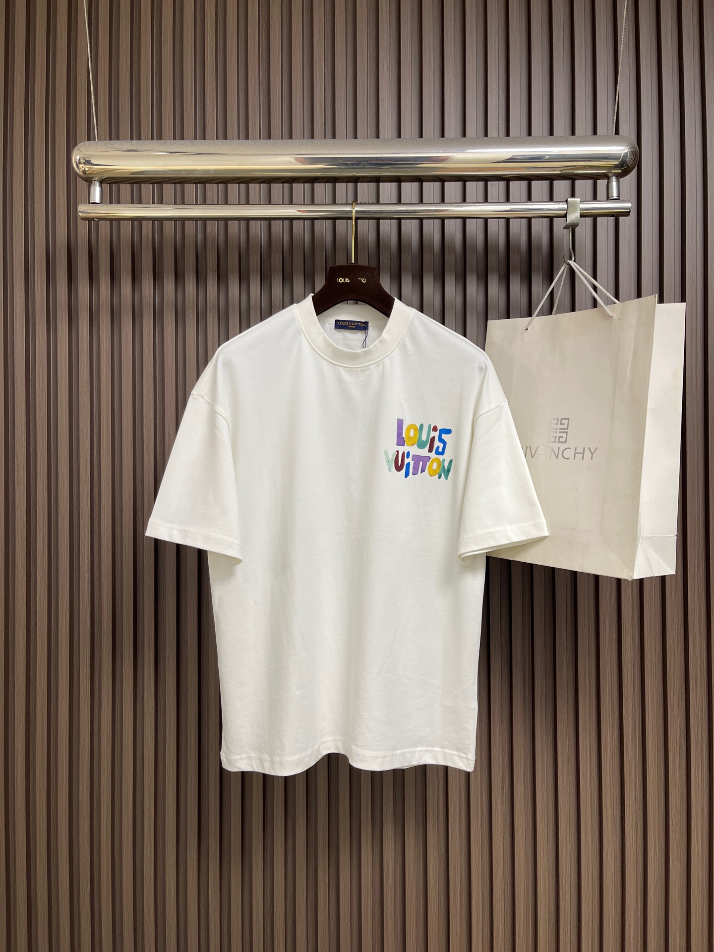 NO:945817,LV  Printed logo short-sleeved T-shirt, made of 15S fine cotton jersey fabric, with a weight that balances softness and skin-friendliness with moderate bone texture. The combing process makes the fibers closely arranged, and the cloth surface presents a delicate and smooth texture. The neckline is matched with 32S double yarn high-density ribbing, which gives it excellent resilience and anti-deformation capabilities, ensuring that the neckline remains stiff after long-term wear and washing. The pattern uses environmentally friendly elasticity  Glue printing technology, through the combination of water-based environmentally friendly slurry and polymer cross-linking agent, realizes the elastic combination of the printing layer and the fabric base. The process makes the pattern appear matte texture and old tone, with high tensile resilience, ensuring that the printing will not crack with the movement of the fabric. It feels flexible and smooth without glue film, maintaining the original breathability of the fabric while giving the pattern a retro texture. Size M-XXL  M size bust 108 shoulder width 55 length 68.5 L size bust 112 shoulder width 57 length 70.519860909LV 印花标识短袖T恤,采用15S精棉平纹针织面料,克重平衡了柔软亲肤性与适度骨感.精梳工艺使纤维排列紧密,布面呈现细腻光洁的质感.领口搭配32S双纱高密罗纹,赋予其卓越的回弹性与抗变形能力,确保领口在长期穿洗后仍保持挺括形态.图案运用环保弹力胶浆印花技术,通过水性环保浆料与高分子交联剂配合,实现印花层与面料基底的弹性结合.工艺使图案呈现哑光质感与做旧色调,具备高拉伸回弹性,确保印花随面料活动不开裂.触感柔韧平滑无胶膜感,保持面料原有透气性,同时赋予图案复古肌理.尺码M-XXL M码 胸围108 肩宽55 衣长68.5 L码 胸围112 肩宽57 衣长70.5 XL码胸围116 肩宽59 衣长72.5 XXL码 胸围120 肩宽60 衣长74.5,,louis vuitton,T-shirt,tees，t-shirt,,Men's clothing