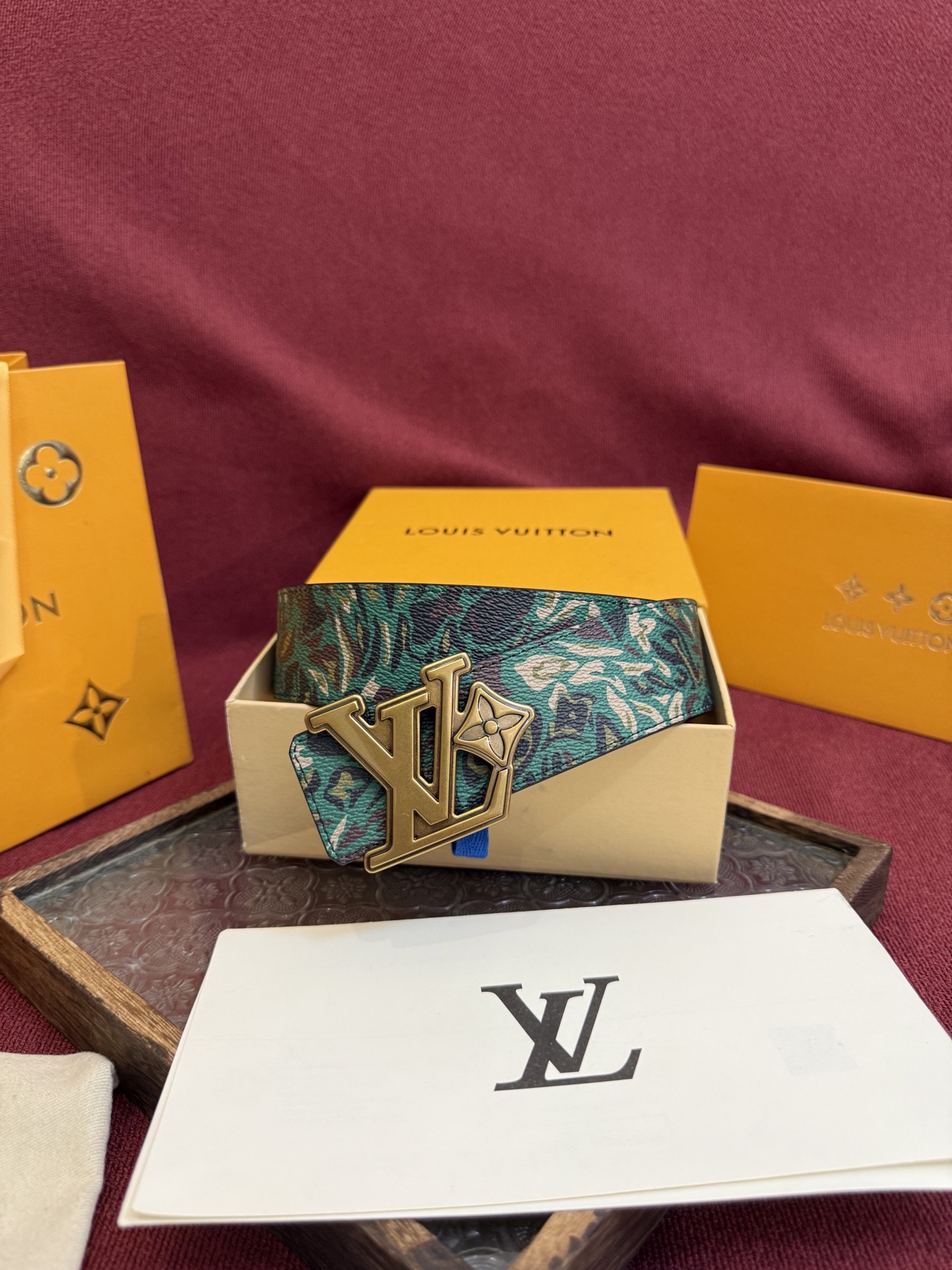 LV花卉迷彩40mm可翻转腰带是对户外爱好者长期青睐的男性主题的一次巧妙重新诠释。柔和的色调被转化为漩涡形状与品牌标识的融合。作为一款时尚优雅的替代品，反面的材质则是黑色皮革。带有花卉标识的银色扣子既适合前卫时尚的选择，也完全契合整体风格。P160