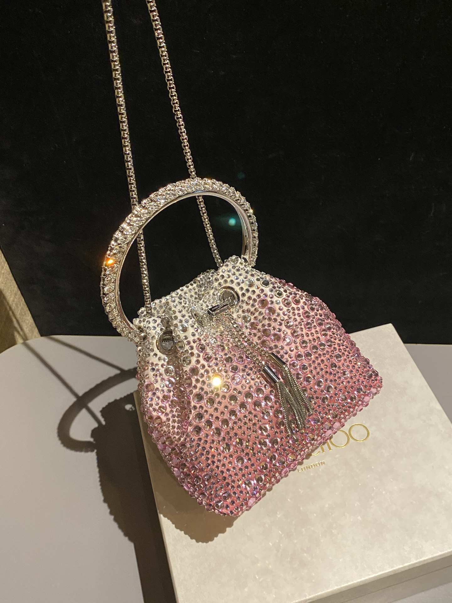 JIMMY CHOO
BON BON系列标志款手提包，光滑缎面铺嵌渐变水晶制作。
设计灵感源于软硬质感及甜美与张扬气质的强烈对比，点睛配以标志性金属流苏，成就如BON BON之名般个性别致又优雅迷人的时尚包袋。现代感桶包廓形，配以手环造型顶部提手，提手饰有百粒经三天精工颗颗细嵌的水晶，精美雅致，招牌奢华包袋当属本款BON BON手提包。
缎面烫钻水晶手嵌水晶饰手环提手Jimmy Choo logo压印金属流苏开合链条肩带内层口袋包袋尺寸：16（长）x15（高）x9.5（宽）厘米肩带长度：55厘米提手长度：9厘米 20259 