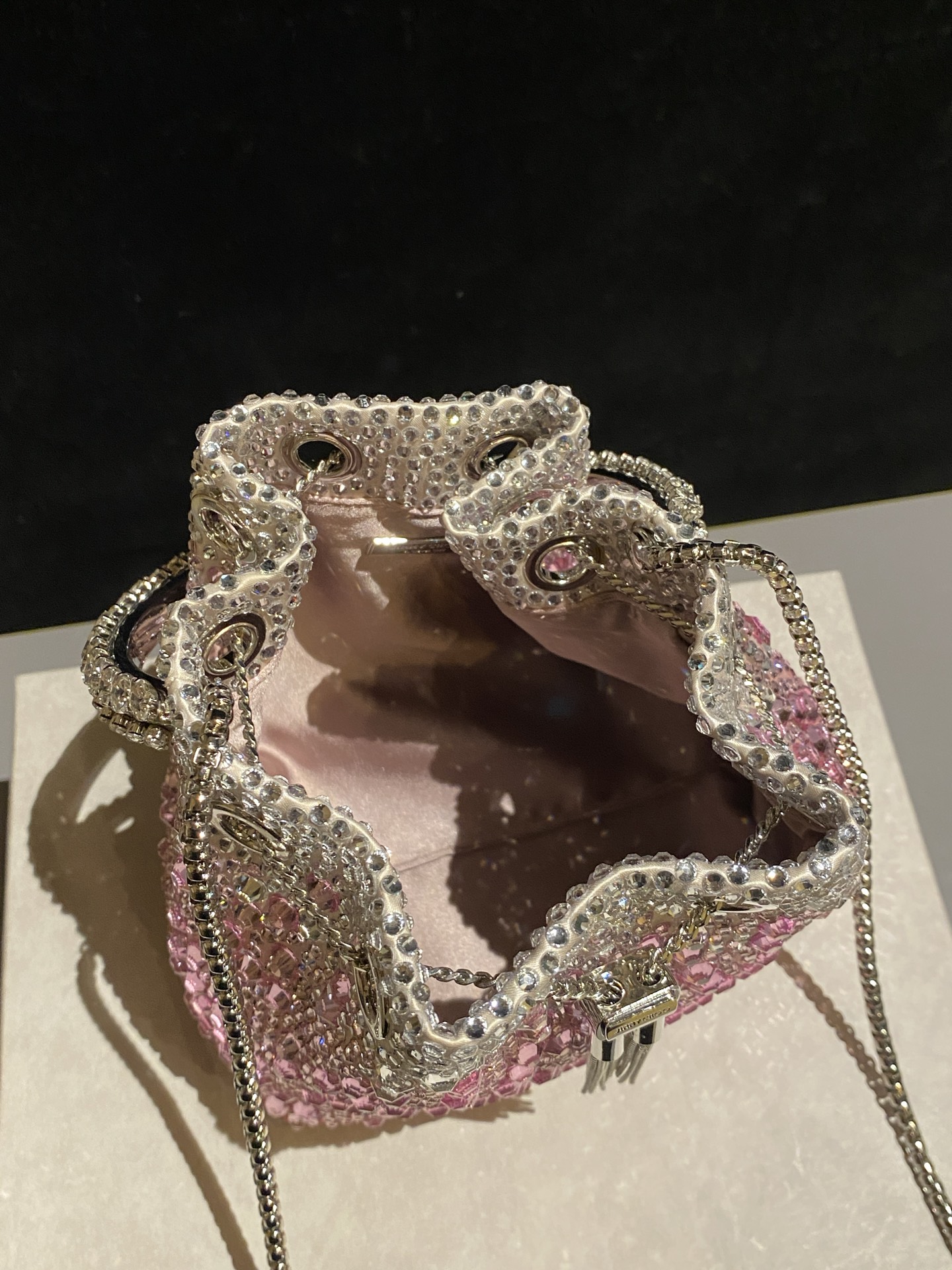 JIMMY CHOO
BON BON系列标志款手提包，光滑缎面铺嵌渐变水晶制作。
设计灵感源于软硬质感及甜美与张扬气质的强烈对比，点睛配以标志性金属流苏，成就如BON BON之名般个性别致又优雅迷人的时尚包袋。现代感桶包廓形，配以手环造型顶部提手，提手饰有百粒经三天精工颗颗细嵌的水晶，精美雅致，招牌奢华包袋当属本款BON BON手提包。
缎面烫钻水晶手嵌水晶饰手环提手Jimmy Choo logo压印金属流苏开合链条肩带内层口袋包袋尺寸：16（长）x15（高）x9.5（宽）厘米肩带长度：55厘米提手长度：9厘米 20259 