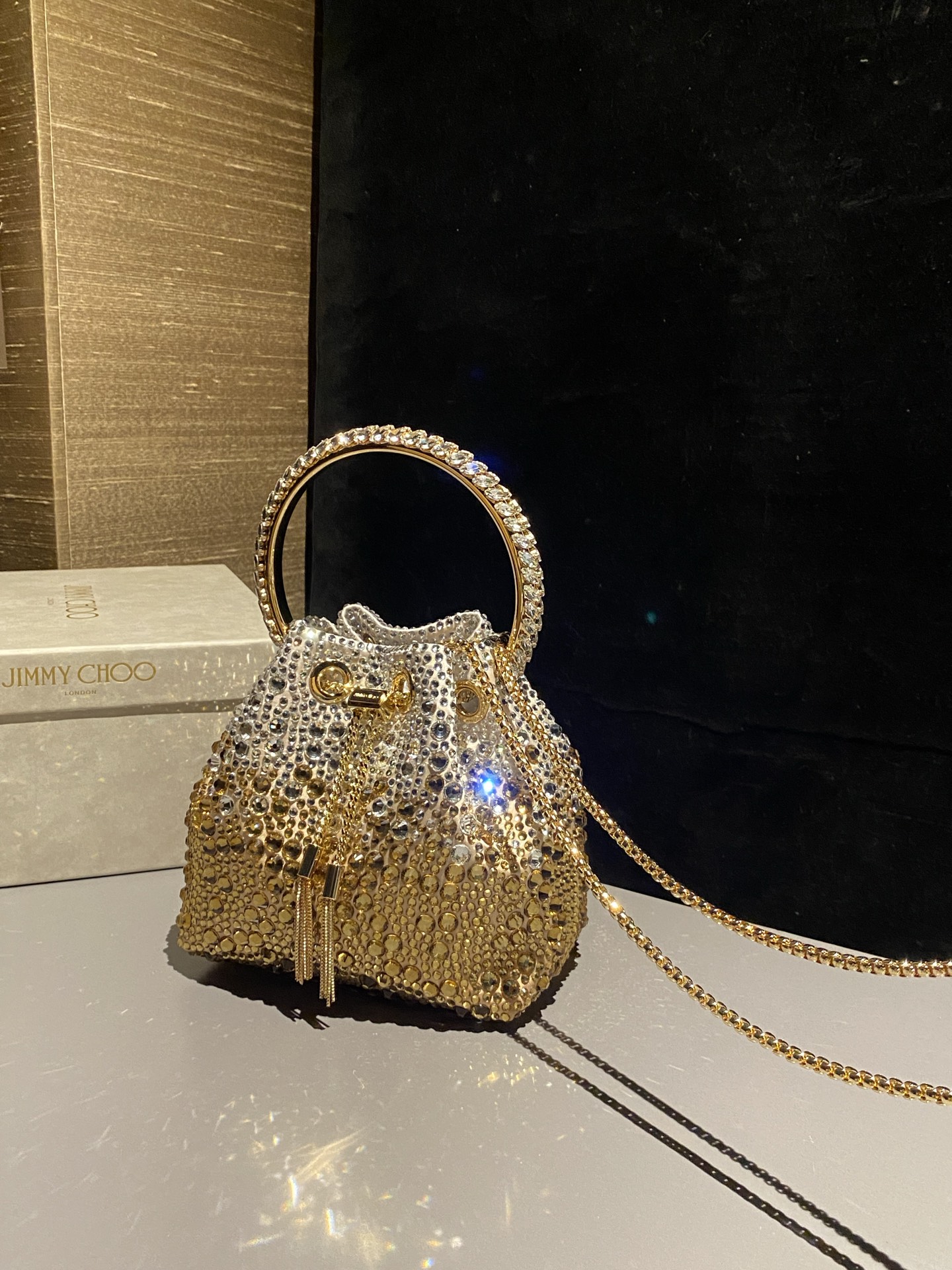 JIMMY CHOO
BON BON系列标志款手提包，光滑缎面铺嵌渐变水晶制作。
设计灵感源于软硬质感及甜美与张扬气质的强烈对比，点睛配以标志性金属流苏，成就如BON BON之名般个性别致又优雅迷人的时尚包袋。现代感桶包廓形，配以手环造型顶部提手，提手饰有百粒经三天精工颗颗细嵌的水晶，精美雅致，招牌奢华包袋当属本款BON BON手提包。
缎面烫钻水晶手嵌水晶饰手环提手Jimmy Choo logo压印金属流苏开合链条肩带内层口袋包袋尺寸：16（长）x15（高）x9.5（宽）厘米肩带长度：55厘米提手长度：9厘米 20259 