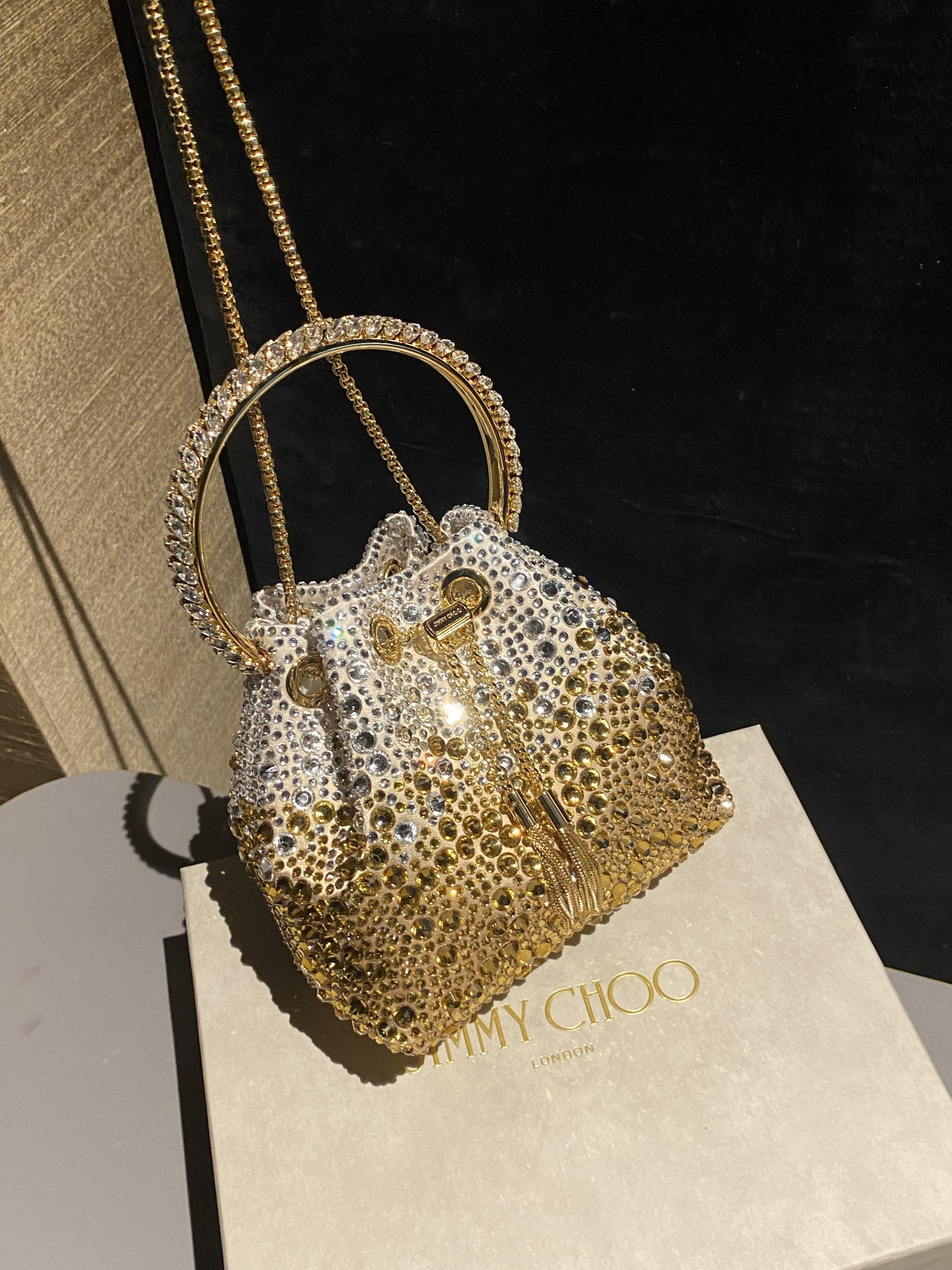 JIMMY CHOO
BON BON系列标志款手提包，光滑缎面铺嵌渐变水晶制作。
设计灵感源于软硬质感及甜美与张扬气质的强烈对比，点睛配以标志性金属流苏，成就如BON BON之名般个性别致又优雅迷人的时尚包袋。现代感桶包廓形，配以手环造型顶部提手，提手饰有百粒经三天精工颗颗细嵌的水晶，精美雅致，招牌奢华包袋当属本款BON BON手提包。
缎面烫钻水晶手嵌水晶饰手环提手Jimmy Choo logo压印金属流苏开合链条肩带内层口袋包袋尺寸：16（长）x15（高）x9.5（宽）厘米肩带长度：55厘米提手长度：9厘米 20259 