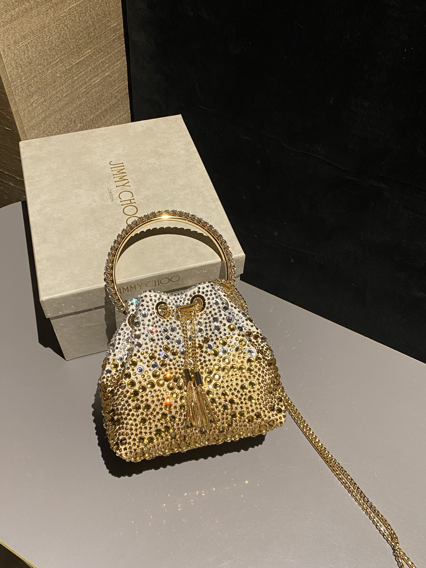 JIMMY CHOO
BON BON系列标志款手提包，光滑缎面铺嵌渐变水晶制作。
设计灵感源于软硬质感及甜美与张扬气质的强烈对比，点睛配以标志性金属流苏，成就如BON BON之名般个性别致又优雅迷人的时尚包袋。现代感桶包廓形，配以手环造型顶部提手，提手饰有百粒经三天精工颗颗细嵌的水晶，精美雅致，招牌奢华包袋当属本款BON BON手提包。
缎面烫钻水晶手嵌水晶饰手环提手Jimmy Choo logo压印金属流苏开合链条肩带内层口袋包袋尺寸：16（长）x15（高）x9.5（宽）厘米肩带长度：55厘米提手长度：9厘米 20259 