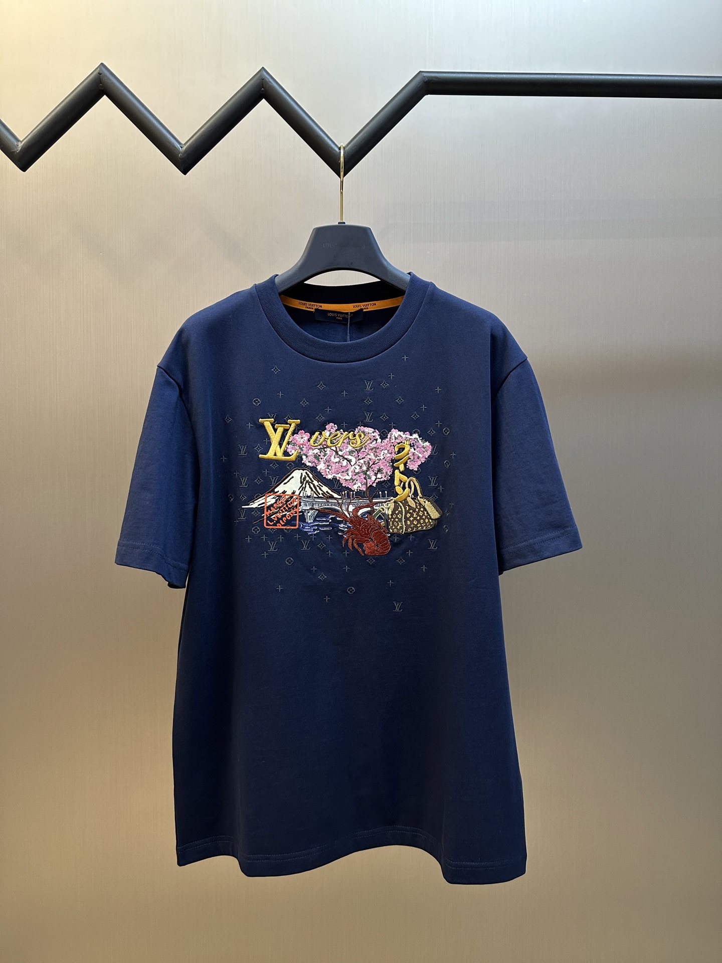 NO:845745,Lv Nigo series lobster embroidered round neck short sleeves  Plain weave pure cotton high-quality cotton fabric, using 15S plain weave high-quality cotton, 230g; with 32S double yarn stretcher thread, 300g. The fabric is a high-quality pure cotton fabric woven in a plain weave. The characteristics of this fabric include vertical intersection of warp and weft yarns, clear texture of warp and weft yarns on the cloth surface, soft hand feel, comfortable wearing, good hygroscopicity, strong air permeability, not easy to deform, washable and durable, etc.  The front pattern is formed by a combination of multiple complex processes; 21 colors of line trimming are processed with high precision. Environmentally friendly elastic glue printing High-quality environmentally friendly elastic glue not only has good printing performance and adhesion, but also ensures the clarity and color brightness of the printed pattern. Excellent elasticity and environmental protection performance can form long-lasting and bright printing effects on various fabrics. White ink digital printing  It is a printing process that uses digital printing equipment to directly spray white ink onto the fabric. The ink droplets form dense dots on the fabric to form a complete pattern. The printing effect is bright in color, delicate in pattern, and strong in layering. Tatami and towel embroidery process Tatami embroidery requires precise control of stitch length; towel embroidery requires high tension to ensure consistent terry height. The concave and convex texture of tatami and the three-dimensional sense of towel embroidery will form dynamic shadows under side light, enhancing the effect of light and shadow utilization.  Tatami embroidery uses regular geometric arrangements to form concave and convex textures, filling large-area background color blocks; it provides a stable base for the pattern and enhances the regularity of the overall structure. Towel embroidery forms a three-dimensional plush effect through embroidery thread circles, which is soft to the touch and suitable for expressing fluffy elements; as the visual focus of the pattern, it highlights the three-dimensional sense and soft texture. sizes m l,, louis vuitton, T-shirt,19860909Lv Nigo系列 龙虾刺绣圆领短袖 平织纯棉优质棉面料,采用15S平织优质棉,230g；搭配32S双纱拉架螺纹,300g.面料采用平纹组织方式织造的品质优良的纯棉面料.这种面料的特点包括经纬纱线垂直相交,布面经纬纱线纹理清晰,手感柔软,穿着舒适,吸湿性好,透气性强,不易变形,耐洗耐穿等. 前幅图案采用多种复杂工艺结合形成；21色修线高精准处理. 环保弹力胶浆印 优质的环保弹力胶浆不仅具有良好的印刷性能和附着力,还能确保印花图案的清晰度和色彩鲜艳度.优良的弹性和环保性能,能够在各种织物上形成持久、鲜艳的印花效果. 白墨数码印花 使用数码印花设备将白色墨水直接喷射到织物上进行印花的工艺.墨滴在织物上形成密集的网点,从而构成完整的图案.印花效果色彩鲜艳、图案细腻、层次感强. 榻榻米与毛巾刺绣工艺结 榻榻米刺绣需精准控制针距；毛巾刺绣需调高张力,确保毛圈高度一致.榻榻米的凹凸纹理与毛巾刺绣的立体感在侧光下会形成动态阴影,光影利用效果增强. 榻榻米刺绣以规则的几何排列形成凹凸肌理,填充大面积背景色块；为图案提供稳定的基底,增强整体结构的规整感. 毛巾刺绣通过绣线绕圈形成立体毛绒效果触感柔软,适合表现蓬松元素；作为图案的视觉焦点,突出立体感和柔软质感. sizes m l,,louis vuitton,T-shirt,,Men's clothing