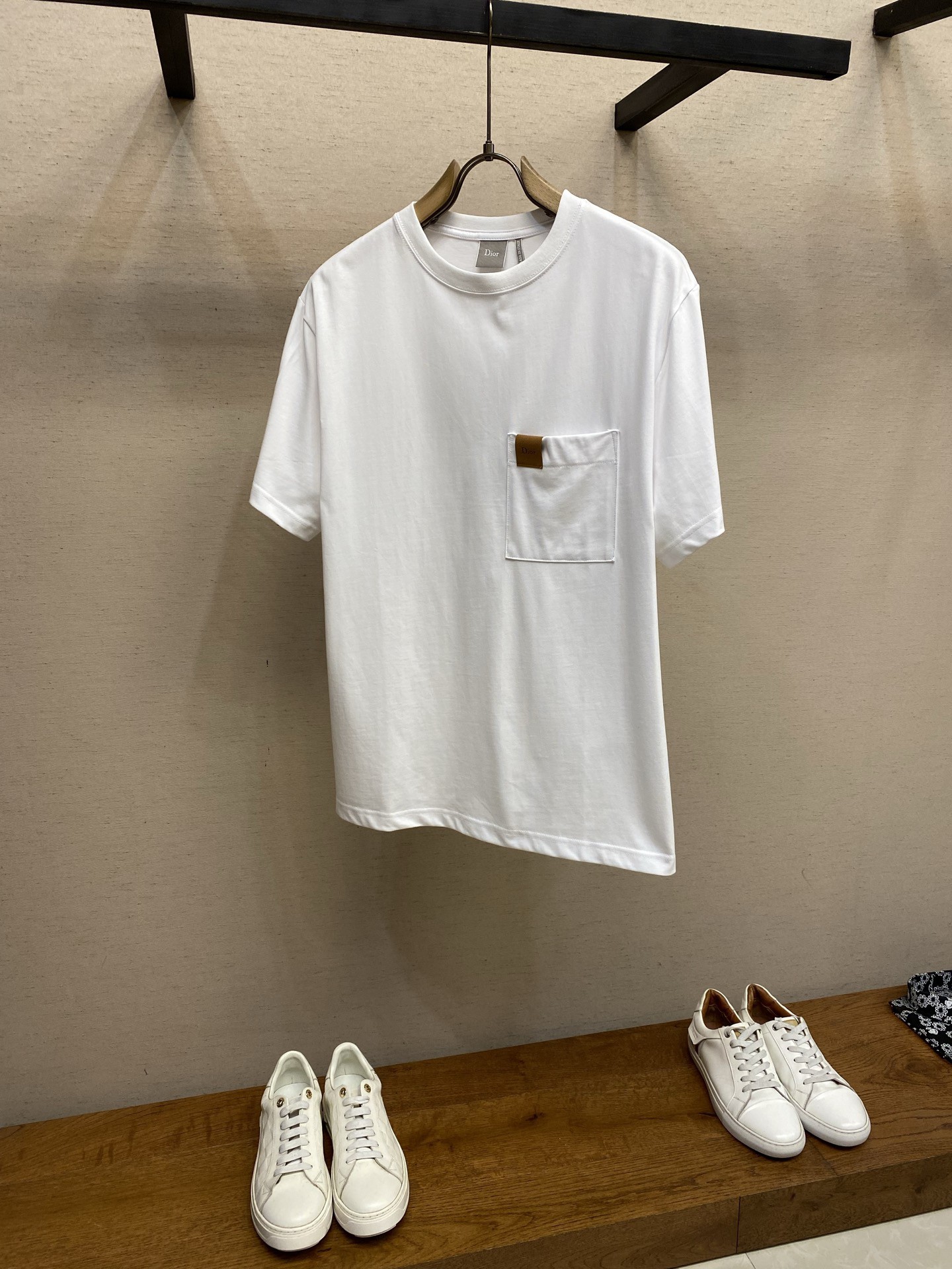 NO:845715,Dior Leather Logo Round Neck Short Sleeve. Available in white color. Original purchase: 700. Cotton jersey fabric, logo leather patch on the front, chest patch pocket decoration, black washed distressed craftsmanship, ribbed round neck, new accessories. #cotton jersey fabric. This product is made of  15-count special-spun compact cotton plain knitted fabric with a weight of 230g/㎡; paired with 32-count 1×1 high-elastic ribs with a weight of 340g/㎡. The special-spun compact cotton uses compact spinning technology in the spinning process, which effectively reduces yarn hairiness, making the fabric structure denser and the surface smoother.  It has better pilling resistance. The fabric is medium to heavy, which ensures the T-shirt has good stiffness, drape and wrinkle resistance, and is not easy to collapse and deform. High-elastic ribbing is used on the neckline, which provides excellent elastic recovery, thickness and deformation resistance, and is the key to ensuring that the neckline of high-quality T-shirts remains stiff for a long time.  # Chest patch pocket and Dior leather patch. A chest patch pocket is sewn into the front chest of the T-shirt as a classic square pocket. It adds layering to the style and workwear or college-style details, breaking the monotony of the solid color basic style.  The Dior leather patch is a high-quality calfskin patch made by laser cutting, edge processing and brand logo embossing. It is fixed on the patch pocket through precision sewing. On the soft cotton base, the crisp and glossy leather material is introduced to form a strong texture contrast, which instantly enhances the sophistication and brand recognition of the T-shirt and becomes the finishing touch of the overall look. # Black washed fade effect  A unique technology that simulates the natural old feel through controlled stone grinding, enzyme washing and other processes. The original dye in the cotton fiber is partially removed, forming uneven fading marks on the dark base, thereby creating a soft, retro grayscale visual effect.  Not only can it give the fabric a unique nostalgic charm and soft layering, but it can also significantly improve the feel of the fabric, making it appear soft and relaxed after wearing, avoiding the stiffness of new fabrics. Each finished product has a slightly different fading distribution, ensuring the uniqueness of the single product. # Standard round neck straight fit  The straight three-dimensional tailoring achieves a balance between looseness and lines by optimizing the shoulder line structure. In response to the load-bearing requirements of the front patch pocket, an anti-stretch support layer is formed to effectively offset the impact of the weight of the leather on the cotton base. All seams are completed with a three-needle five-thread interlock sewing machine, combined with ultrasonic cutting and hot-melt edge sealing pre-treatment to ensure that the seams are smooth and burr-free, achieving zero-touch wearing comfort.  Size S-L,,dior,T-shirt,tees,t-shirt,cowhide,19860909Dior 皮革标志圆领短袖 发售色系白色 原,700购买；棉质平纹针织面料、正面饰以标志皮革补丁、胸前贴袋装饰、黑色洗水做旧工艺、罗纹圆领、新款辅料配备 # 棉质平纹针织面料 本品采用 15支特纺紧密棉平纹针织面料,克重为230g/㎡；搭配32支1×1高弹罗纹,克重为340g/㎡.特纺紧密棉在纺纱环节应用了紧密纺技术,有效减少了纱线毛羽,使得面料结构更密实、表面更光洁、抗起球性更佳.面料重属于中等偏重磅,确保了T恤良好的挺括感、垂坠性和抗皱性,不易软塌变形.高弹罗纹用于领口,提供了卓越的弹性恢复力、厚实感和抗变形能力,是保证高品质T恤领口长久挺括的关键. # 胸前贴袋与Dior皮革补丁 胸前贴袋在T恤前胸位置缝制一个贴袋为经典方形口袋.增加款式的层次感和工装或学院风细节,打破了纯色基础款的单调. Dior皮革补丁将经过激光切割、边缘处理及品牌标识压印工艺制成的优质小牛皮补丁,通过精密缝制的方式,固定在贴袋上.在柔软的棉质基底上,引入挺括且富有光泽感的皮革材质,形成强烈的质感对比,瞬间提升T恤的精致度和品牌辨识度,成为整体造型的点睛之作. # 黑色水洗褪色效果 通过控制性的石磨、酶洗等工艺,模拟自然旧化感的独特技术.部分去除棉纤维中的原身染料,在深色基底上形成不均匀的褪色痕迹,从而营造出柔和、复古的灰度视觉效果. 不仅能赋予织物独特的怀旧韵味与柔和层次感,更能显著改善面料手感,使其预先呈现穿着后的柔软与松弛状态,避免了新面料的生硬感.每一件成品均拥有细微差异的褪色分布,确保了单品的独一性. # 标准圆领直身版型 直身立体剪裁,通过优化肩线结构实现宽松度与线条感的平衡.针对前幅贴袋承重需求,形成抗拉伸支撑层,有效抵消皮革重量对棉质基底的下坠影响.所有缝接位均以三针五线绷缝机完成,配合超声波切割与热熔封边预处理,确保缝份平整无毛刺,达成零触感穿着舒适度. 尺码S-L,,dior,T-shirt,tees，t-shirt,cowhide,,Men's clothing