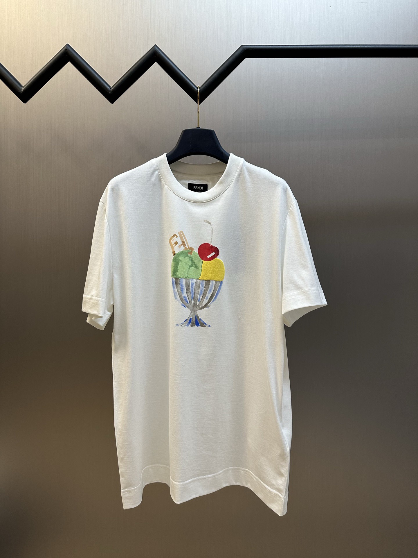 NO:845734,FD Sundae Ice Cream Round Neck Short Sleeve Pure cotton mercerized fabric, using 50-count double-strand mercerized cotton, with a weight of 165g/㎡; paired with 32-count double-yarn rib, with a weight of 300g/㎡. The fabric is a high-count, light knitted fabric, and the 50-count yarn is extremely fine. The double-strand twisting makes the yarn structure tight and even, giving the fabric a silky smooth feel and high-end luster. Mercerization is the core process of cotton fiber cutting. The surface is rounded, which significantly enhances the gloss and dyeing depth, while improving the strength and dimensional stability. After mercerization, it feels silky smooth, providing a flat, highly absorbent base fabric for subsequent water slurry printing, ensuring natural color transitions and clear boundaries for the color matching watercolor effect. The double yarn structure makes the rib tissue denser and fuller, with excellent elastic recovery rate, which can effectively prevent the collar from loosening and deforming. Color-blocking watercolor effect ice cream printing pattern, the front ice cream printing uses a combination of dot paste printing + suede foam printing process to achieve the dual expression of color-blocking watercolor effect and three-dimensional touch. Dot paste printing uses a fine screen to overprint the color paste in the form of dots, and uses the size and density changes of the dots to simulate the gradient, blooming and overlapping effects of watercolor painting. The colors are rich in layers and breathable without clumping. Suede foam printing is used in specific areas of the ice cream. When baked at high temperatures, the foamed microspheres expand to form a three-dimensional bulge that feels soft and fluffy. The combination of the two processes makes the pattern have the romantic hazy feeling of watercolor painting and a touchable three-dimensional interest. Standard loose fit, using standard fit design, the shoulder line accurately falls on the acromion point, the sleeve shape is standard short sleeves, the body is straight cut, and the bust and hem circumferences are similar. The delicate drape characteristics of mercerized cotton make the standard fit show a clean and neat line sense; the neckline area presents a delicate and solid touch, which plays a visual convergence effect. sizes m l,, T-shirt,19860909FD 圣代雪糕圆领短袖 纯棉质丝光面料,采用50支双股丝光棉,克重为165g/㎡；搭配32支双纱罗纹,克重为300g/㎡.面料属于高支轻薄型针织面料,50支纱线极细,双股加捻使纱线结构紧密、条干均匀,赋予面料丝般顺滑的触感与高级光泽.丝光处理是核心工序棉纤维截面圆润,显著增强光泽度与染色深度,同时提升强度与尺寸稳定性.经丝光后触感如丝般顺滑,为后续水浆印花提供平整、高吸附性的底布,确保拼色水彩效果的色彩过渡自然、边界清晰.双纱结构使罗纹组织更加致密饱满,弹性恢复率优异,能有效防止领口松垮变形. 拼色水彩效果冰淇淋印花图案,正面冰淇淋印花采用网点浆印花+绒面发泡印花工艺结合,实现拼色水彩效果与立体触感的双重表达. 网点浆印花通过细密网版将色浆以网点形式叠印,利用网点的大小与密度变化模拟水彩画的渐变、晕染与透叠效果,色彩层次丰富且透气不板结. 绒面发泡印花用于冰淇淋的特定区域,经高温烘烤时发泡微球膨胀,形成立体隆起、触感柔软如绒毛的质感.两种工艺结合,使图案既有水彩画的浪漫朦胧感,又有可触摸的立体趣味性. 标准宽松版型,采用标准版型设计,肩线精准落在肩峰点,袖型为标准短袖,衣身呈直筒剪裁,胸围与下摆围度相近.丝光棉的细腻垂坠特性,使标准版型呈现出干净利落的线条感；领口区域呈现精致扎实的触感,起到视觉收敛作用. sizes m l,,T-shirt,,Men's clothing