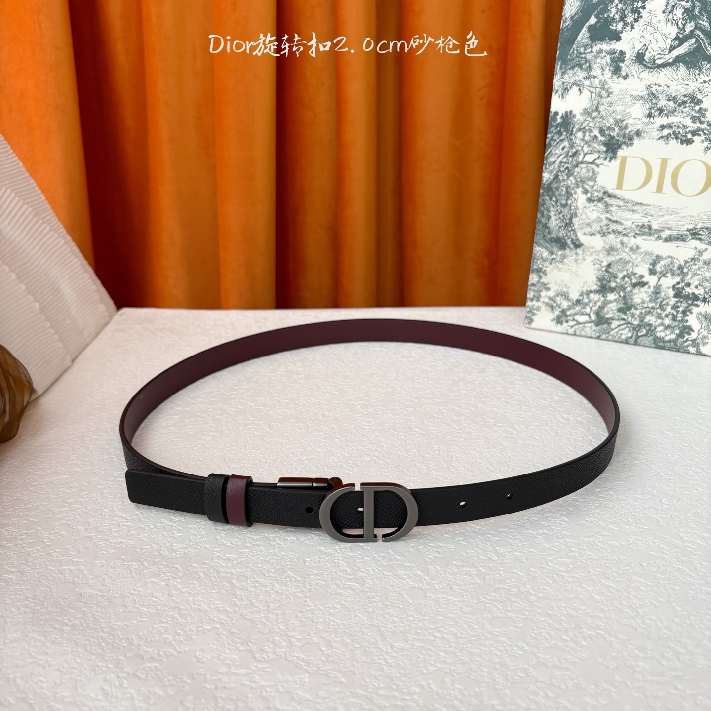 Dior新款腰带一面为黑色颗粒小牛皮,另一面为酒红色光滑小牛皮,缀以经典的亮面金色饰面金属CD扣环。此款