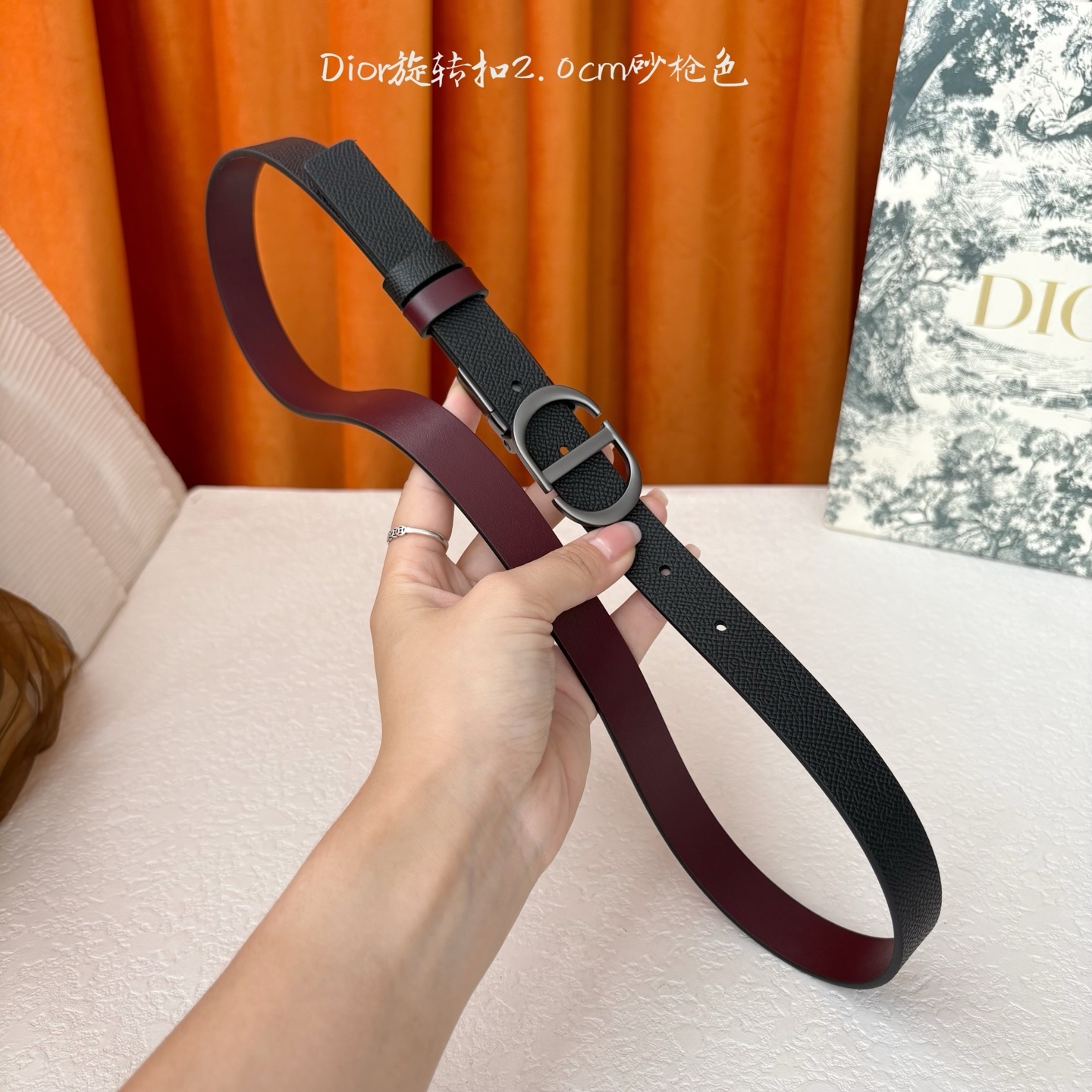 Dior新款腰带一面为黑色颗粒小牛皮,另一面为酒红色光滑小牛皮,缀以经典的亮面金色饰面金属CD扣环。此款