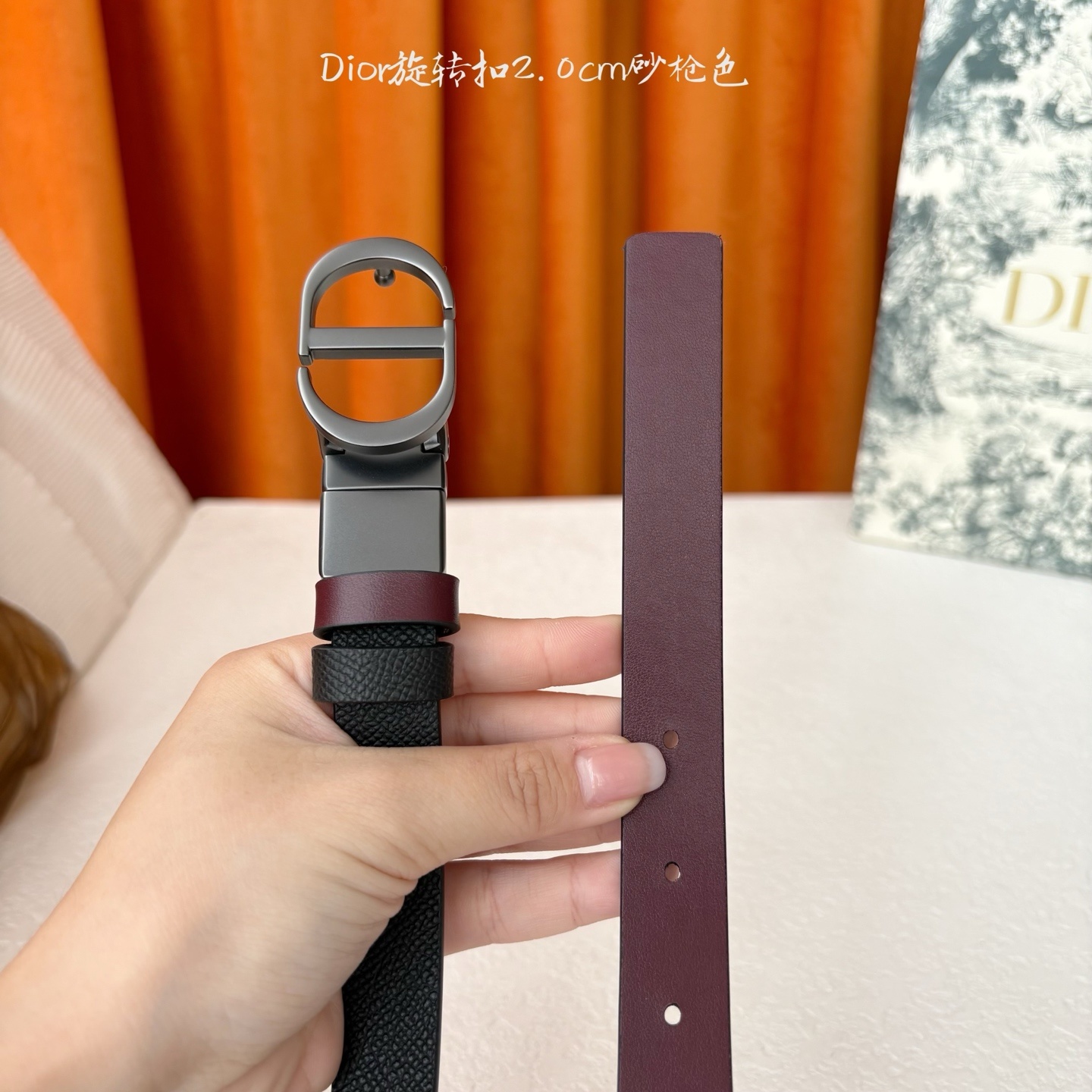 Dior新款腰带一面为黑色颗粒小牛皮,另一面为酒红色光滑小牛皮,缀以经典的亮面金色饰面金属CD扣环。此款