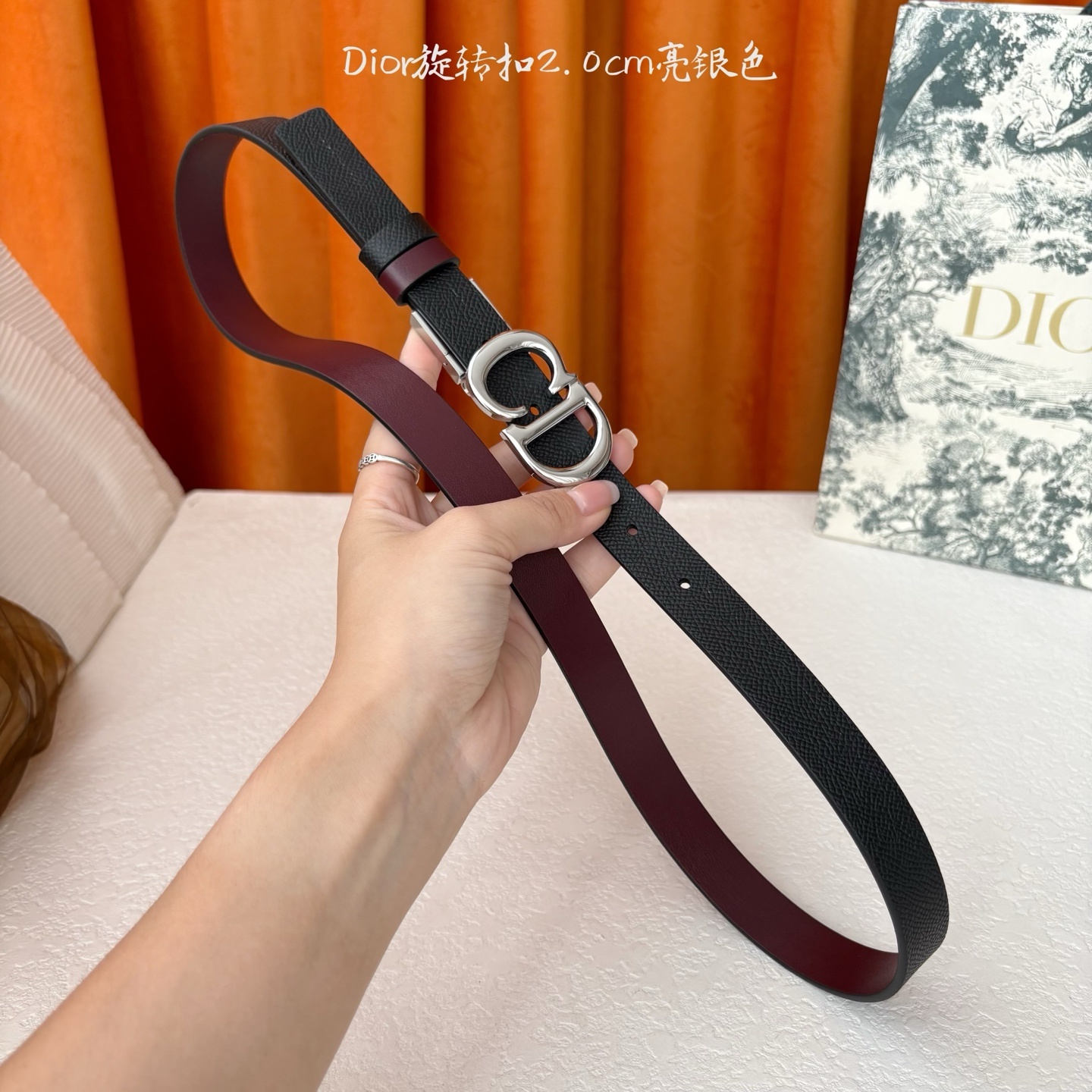 Dior新款腰带一面为黑色颗粒小牛皮,另一面为酒红色光滑小牛皮,缀以经典的亮面金色饰面金属CD扣环。此款