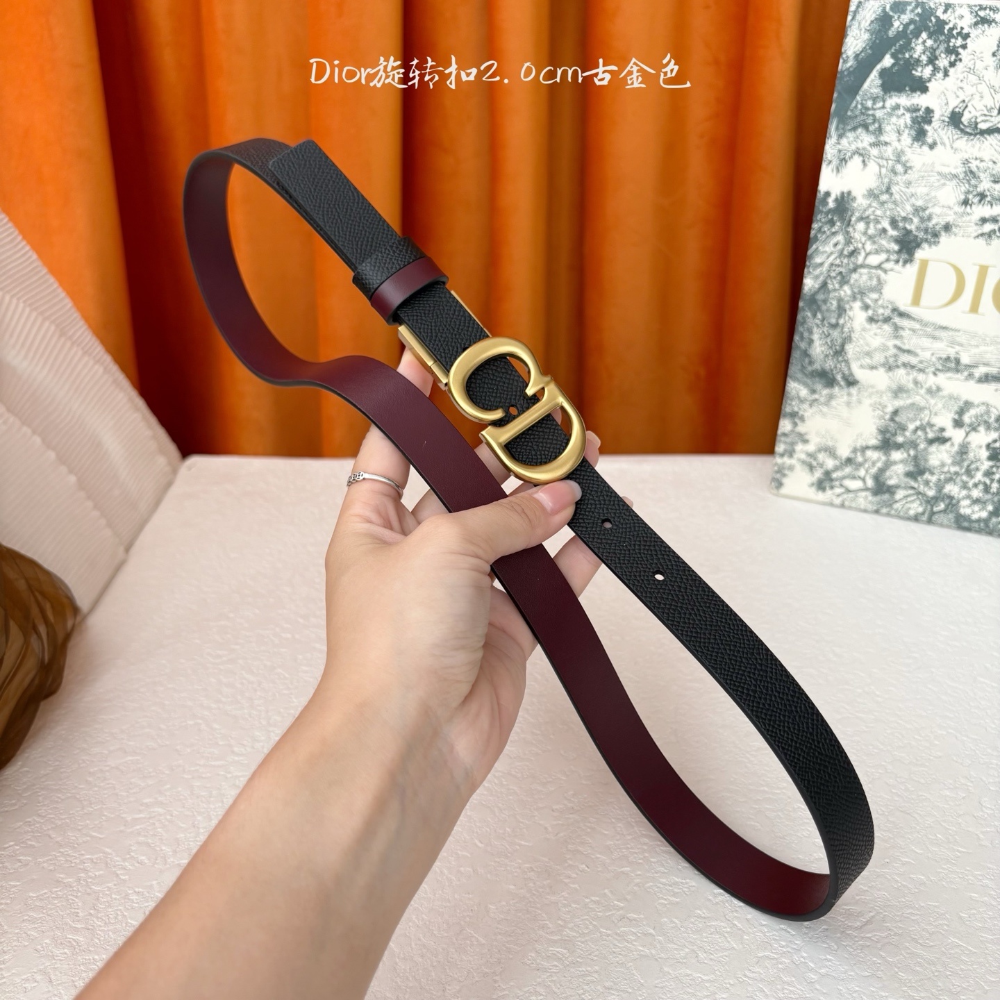 Dior新款腰带一面为黑色颗粒小牛皮,另一面为酒红色光滑小牛皮,缀以经典的亮面金色饰面金属CD扣环。此款