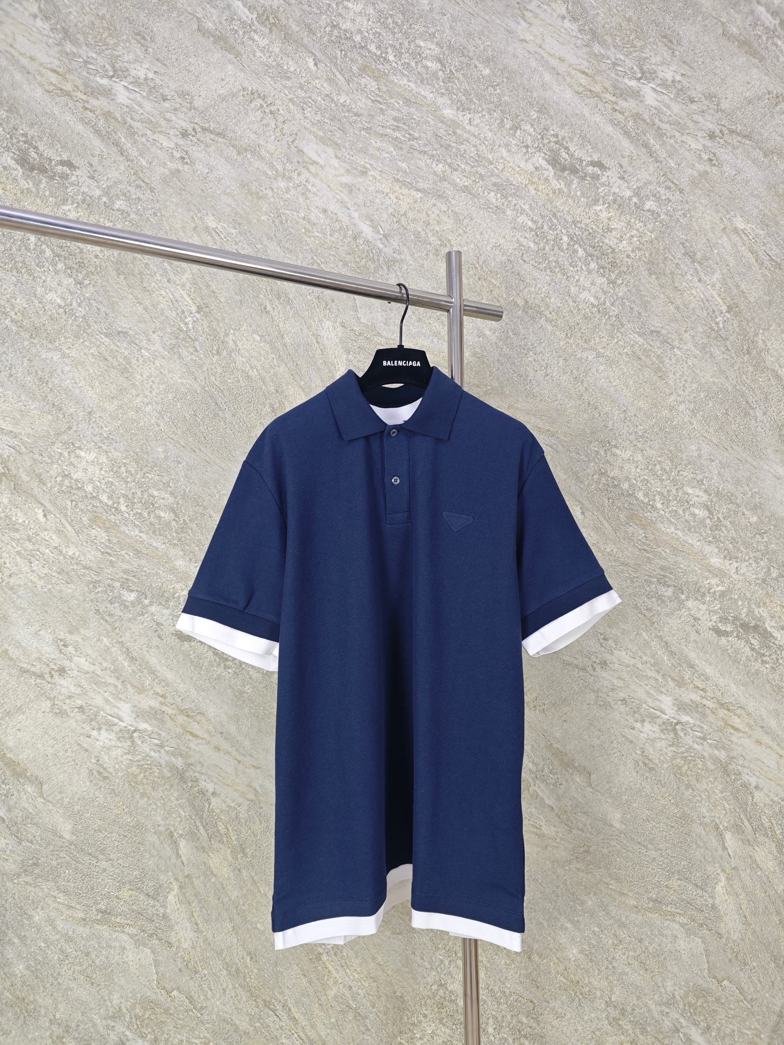 NO:824454,Top-quality Prada embellished contrast fabric triangle logo POLO shirt. Fabric selection: Pique fabric woven from cotton fiber. Cotton fiber gives the fabric the characteristics of moisture absorption, breathability, and skin-friendliness. The surface of the pique structure has uneven holes, shaped like a honeycomb, which promotes air circulation and has excellent heat dissipation efficiency. Because the elasticity of cotton yarn is enhanced after pique weaving, it can still rebound after repeated stretching. Process 1 The rib knitted neckline is knitted using a double needle bed, so that the loops are alternately formed on the front and back, forming a 1*1 rib with longitudinal concave and convex patterns. The elastic structure makes the neckline fit the neck naturally, avoiding a sense of restraint, and the double-layer sewing process links the body, significantly reducing the probability of the neckline expanding into a 'ruffle' and collapsing, and maintaining the initial shape for a long time. Process 2 By actively interfering with the shrinkage potential of cotton fibers, the fabric is able to transition from changeable to stable, improving dimensional stability while being less prone to deformation and wrinkles. Features: Contrast-colored jersey trim gives a sense of layering and enhances visual beauty. Accessories: One-to-one fabric triangle label One-to-one front button Size: S M L XL, Prada-Clothing, prada, prada,19860909顶级品质 Prada饰撞色织物三角标POLO衫 面料选择 选用棉纤维编织而成的珠地布.棉纤维赋予面料吸湿透气,亲肤等特点.珠地结构表面呈现凹凸疏孔,形似蜂巢,促进空气循环,散热效率优良.因棉纱经珠地编织后弹性增强,反复拉伸仍可回弹. 工艺1 罗纹针织领口使用双针床编织,使线圈在正反面交替成圈,形成纵向凹凸纹路的1*1罗纹.弹性结构使领口自然贴合颈部,避免束缚感,加之双层缝纫工艺链接衣身,显著降低领口外扩成“荷叶边”的概率与塌陷,保持长久初始形态. 工艺2 通过主动干预棉纤维收缩潜能,实现了面料从易变到稳定的跨越,提升了尺寸稳定性,同时不易变形,褶皱. 特点 撞色平纹针织饰边赋予层次感,同时强化视觉美感. 辅料一比一织物三角标  一比一前襟纽扣 Size: S M L XL,普拉达-服装,prada,prada,,Women's clothing