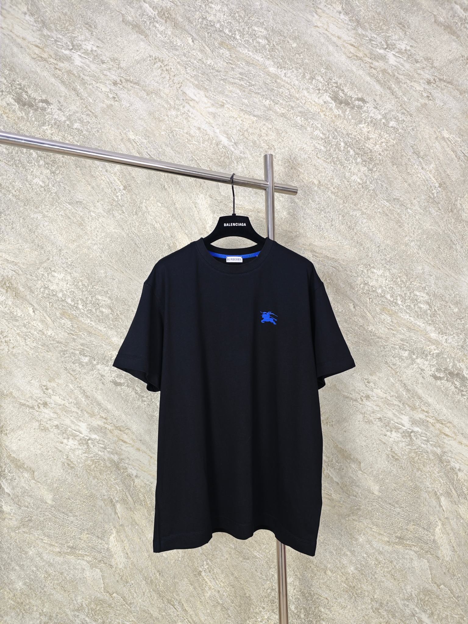 NO:824321,Top Quality BURBERRY War Horse Embroidered Round Neck T-Shirt Fabric Choice  A compact plain cotton fabric made of cotton. The gram weight reaches 200g/m. The fabric is thick and drapey. It is not thin and fleshy, but also ensures a good drape feeling when worn. The upper body is stylish and not soft. The compact spinning process makes the yarn tighter, and the fabric is wear-resistant and wrinkle-resistant. It is not easy to pill or loose after daily machine washing, and can maintain a smooth texture after long-term wear. Pure cotton fiber has a natural soft skin-friendly touch, is breathable and sweat-wicking, and is not stuffy or irritating when worn close to the body.  Embroidery process: Iron the front of the fabric flat in advance, accurately mark the embroidery position, install the embroidery frame into the machine, and align the center point of the pattern. Use high-saturation royal blue embroidery thread and pass it through high-density filling needles. The stitches are fine and even, making the knight and war horse pattern clear and layered, visually embossed and not easy to deform. After finishing, the edges of the pattern are smooth, without hard edges, and there is no foreign body feeling when worn against the skin.  SizeSMLXL,Burberry-clothing,burberry,tees,t-shirt,19860909顶级品质 BURBERRY战马刺绣圆领T恤 面料选择 选用棉打造而成的紧密平纹棉面料.克重达200g/m,面料厚实有垂感,既不会单薄透肉,又能保证良好的穿着垂坠感,上身有型不软塌.紧密纺工艺让纱线更紧实,面料耐磨抗皱,日常机洗不易起球、不易松散,久穿仍能保持平整质感.纯棉纤维具有天然的柔软亲肤触感,透气排汗,贴身穿不闷不刺激. 刺绣工艺 将面料前幅,提前熨烫平整,精准标记刺绣位置,将绣花框装入机台,对齐图案中心点.选用高饱和度宝蓝色绣线通过高密度填充针,针脚细密均匀,使骑士与战马图案轮廓清晰,层次分明,视觉上有浮雕感,不易变形.后整理之后,图案边缘平滑,无硬边,贴肤穿着无异物感. SizeSMLXL,博柏利-服装,burberry,tees，t-shirt,,Women's clothing