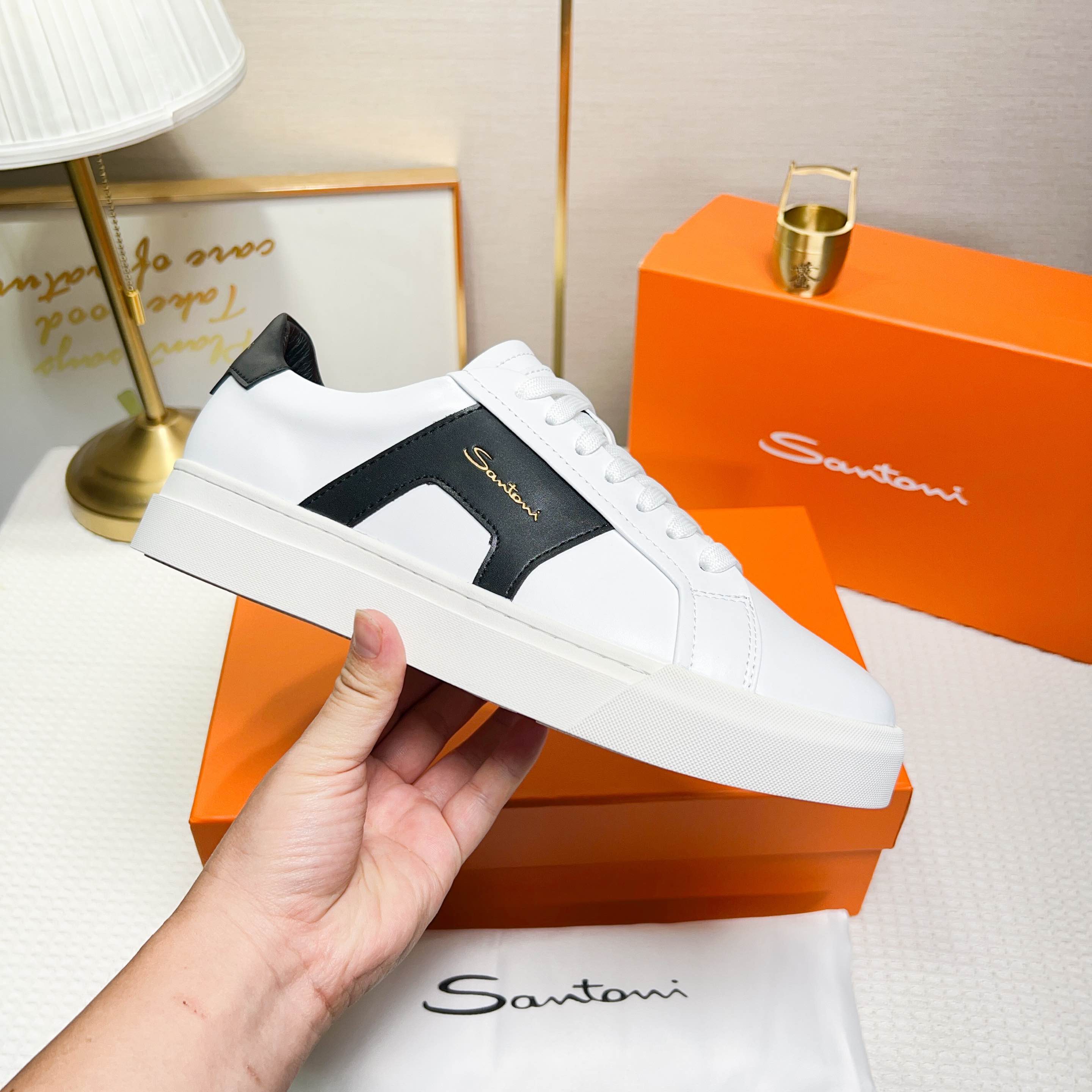 NO:272312,Santoni is a men's low-top sneaker made of leather, in white and orange, with exquisite and distinctive design details. Material and color The shoe is made of leather, the main color is white and black, with bright and fashionable color. Design details The tongue and heel are decorated with leather brand logo, and the side design is designed with double buckles and inspiration for the shoe, which adds to the design sense of the shoe. The style and the shoes are worn are wide and round toe designed, and are comfortable to wear. The lace-up fixing method is used to facilitate adjustment of elasticity. The sole is constructed with rubber cup-shaped sole, which is wear-resistant and has good grip. The sole is molded with Santoni letters to highlight the brand's characteristics. Origin: The shoe is produced in Italy. This sneaker combines fashion and comfort, suitable for daily wear or special occasions.  38-44 codes (45 custom made), sneakers19860909Santoni(圣东尼) 这是一款男士低帮运动鞋,采用皮革材质,颜色 为白色和橙色,设计细节精致且富有特色. 材质与颜色该鞋采用皮革制作,主体颜色为 白色和黑色,配色鲜明且时尚. 设计细节鞋舌和鞋跟处饰有皮革品牌标识, 侧边设计有双扣环灵感的细节,增加了鞋子的设 计感. 版型与穿着鞋子为宽版型和圆头设计,穿着 舒适.采用系带式固定方式,方便调节松紧. 底部构造鞋底为橡胶杯型底,耐磨且具有良 好的抓地力.鞋底模印有Santoni字母,彰显品牌 特色. 产地该鞋产于意大利 这款运动鞋融合了时尚与舒适,适合日常穿着或 特殊场合搭配. 38-44码（45定做）,,sneakers,Men's shoes
